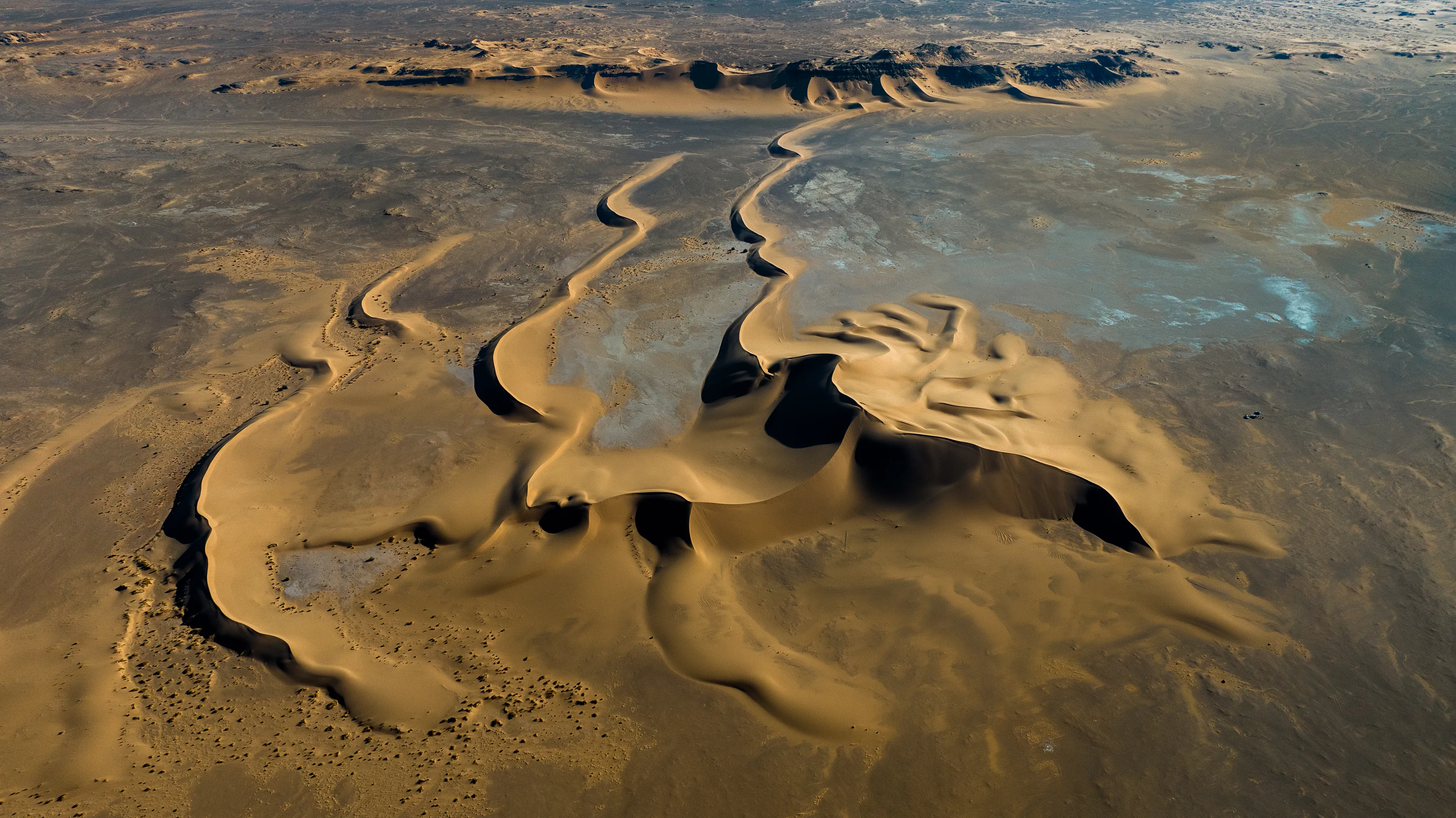 This stunning stretch of sand rises from a dry, flat pan, forming a series of distinctive barchan dunes. We were crossing back through the Sahara from south to north, passing by Magdit along the remote western border between Libya and Algeria, on our way to the ancient caravan town of Ghadames. We found ourselves in the Erg Titersin, a landscape where archaeologists have uncovered stone tumuli and burial structures. As we moved deeper into this immense terrain, we felt incredibly small beside this vast mass of sand dominating the barren desert.