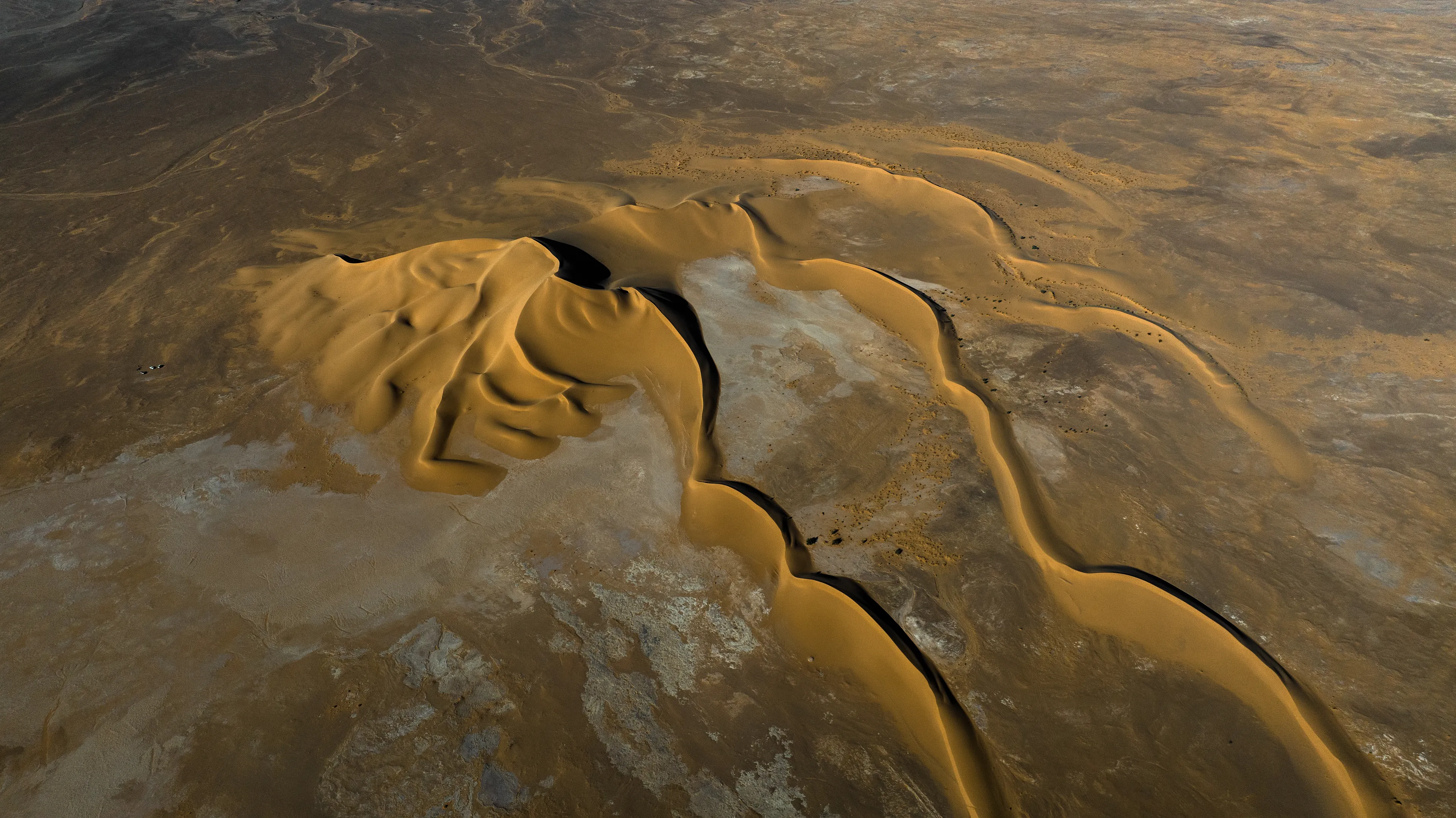 This stunning stretch of sand rises from a dry, flat pan, forming a series of distinctive barchan dunes. We were crossing back through the Sahara from south to north, passing by Magdit along the remote western border between Libya and Algeria, on our way to the ancient caravan town of Ghadames. We found ourselves in the Erg Titersin, a landscape where archaeologists have uncovered stone tumuli and burial structures. As we moved deeper into this immense terrain, we felt incredibly small beside this vast mass of sand dominating the barren desert.