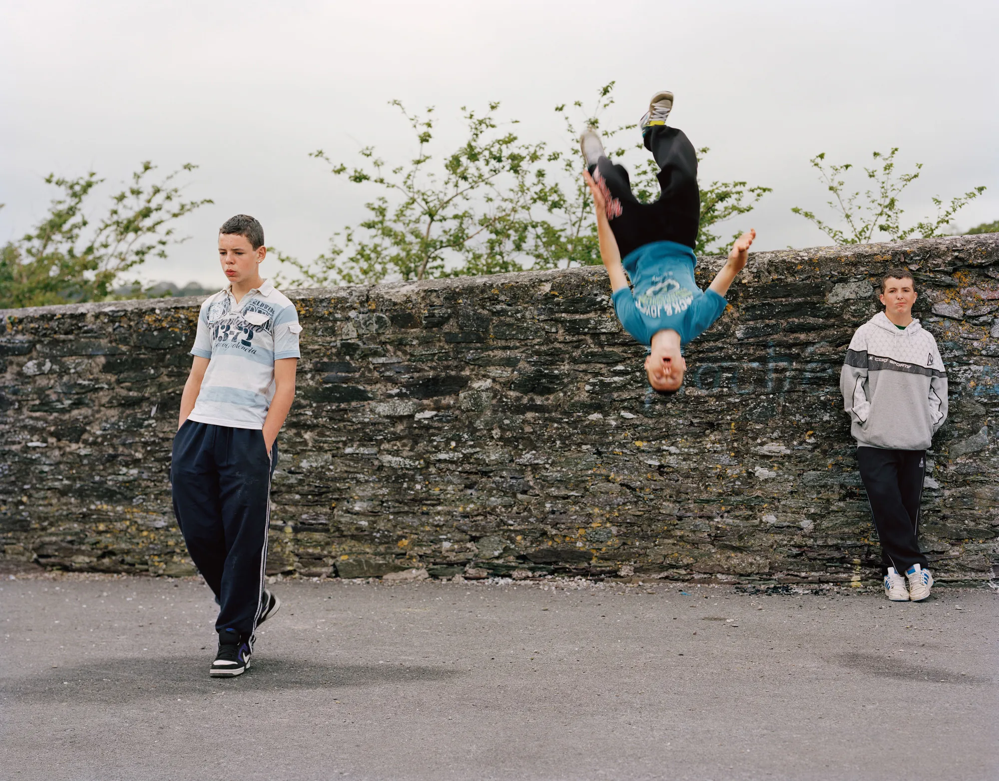 Image caption: Practicing parkour off the seawalls in Cuskinny.

Assembly and Sasha Wolf Projects present “My Last Day at Seventeen,” the genesis NFT collection by an American photographer Doug DuBois. Combining portraits, spontaneous encounters and collaborative performances, the images in "My Last Day at Seventeen" hover between documentary and fiction. Doug DuBois was first introduced to a group of teenagers from the Russell Heights housing estate while he was an artist-in-residence in Cobh, on the southwest coast of Ireland. He was fascinated by the insular neighborhood, in which "everyone seems to be someone's cousin, former girlfriend, or spouse." DuBois gained entry when two participants of a workshop he taught took him to a local hangout spot, opening his eyes to a world of not-quite-adults, struggling through the last days of their childhood. Over the course of five years, DuBois returned to Russell Heights examining the uncertainties of growing up in Ireland today while highlighting the unique relationship between artist and subject.

Doug Dubois is a widely-exhibited American photographer well known for capturing intimate familial scenes. His photographs are in the collection of the Museum of Modern Art in NY; SFMOMA in San Francisco; J. Paul Getty Museum and LACMA in Los Angeles; The Museum of Fine Art in Houston; the Library of Congress in Washington DC; and the Victoria and Albert Museum, London.