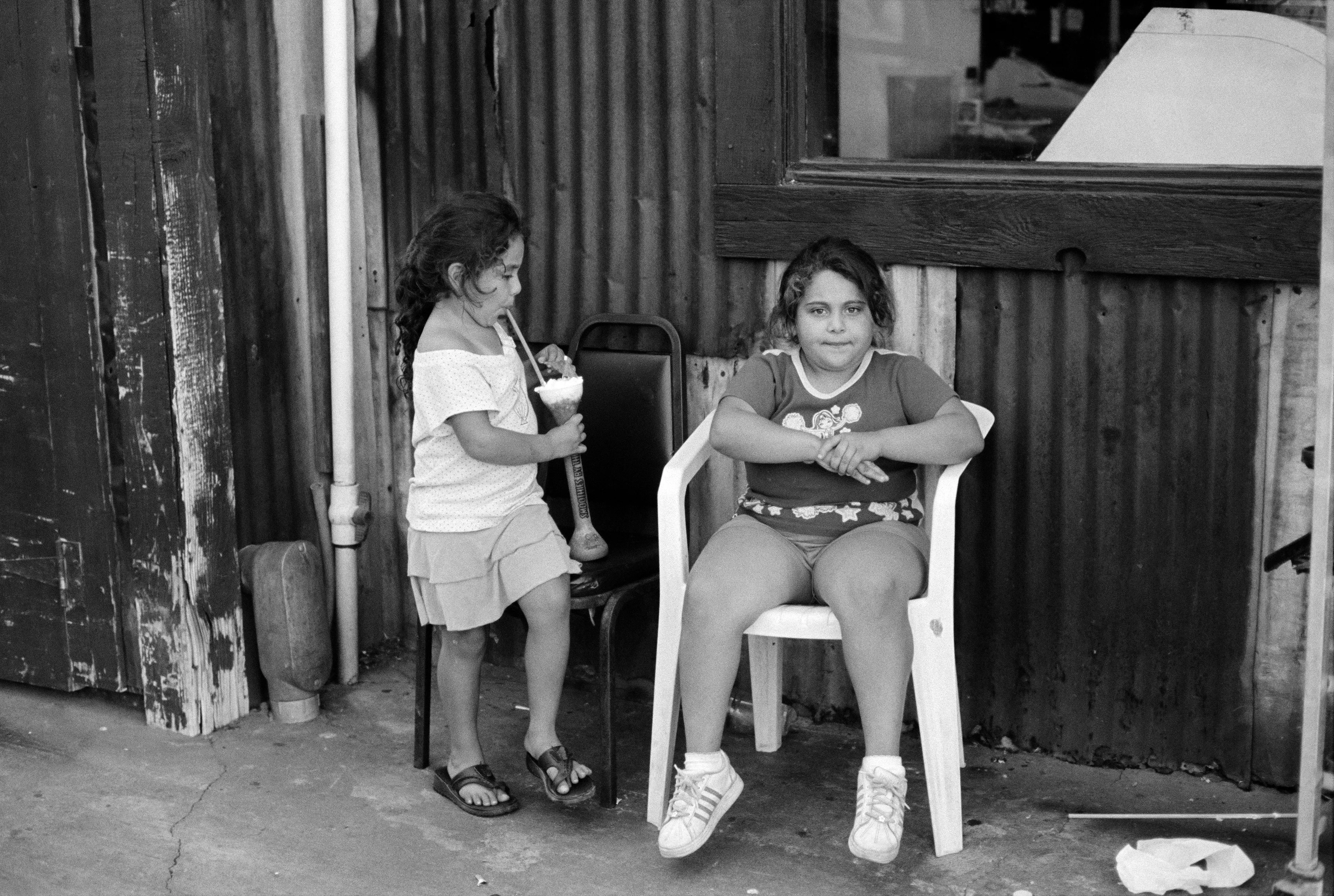 THE VILLAGE #4 TWO LITTLE GIRLS ONE WITH LARGE DRINK by Deanna Templeton

This project started in 2002. A year after my mother passed away, a few years after my father passed. What I remember was one day I was thinking about my parents and feeling a little bit lonely, a little empty and decided to go for a drive. So I decided to drive out to my grandmother's house in San Pedro, which is about a 45 minute drive from where I live. I just wanted to reminisce, to re-explore the surroundings where I would go when I was a child. The liquor store I would walk to to get a Lipton Ice Tea and a bag of Frito’s, to the bakery where I swore all the cookies didn’t have sugar in them and then I drove over to Ports O’Call Village. As soon as I started to walk around I came across a stage with some Mariachis playing and it just hit me, I felt like I was home, I was with family. Over the next 5 years, whenever I could, I started going out there on the weekends. Getting reacquainted with the village and the locals. To shoot everything I wanted to remember.

Edition: 1 of 1

Commissioned by Obscura
