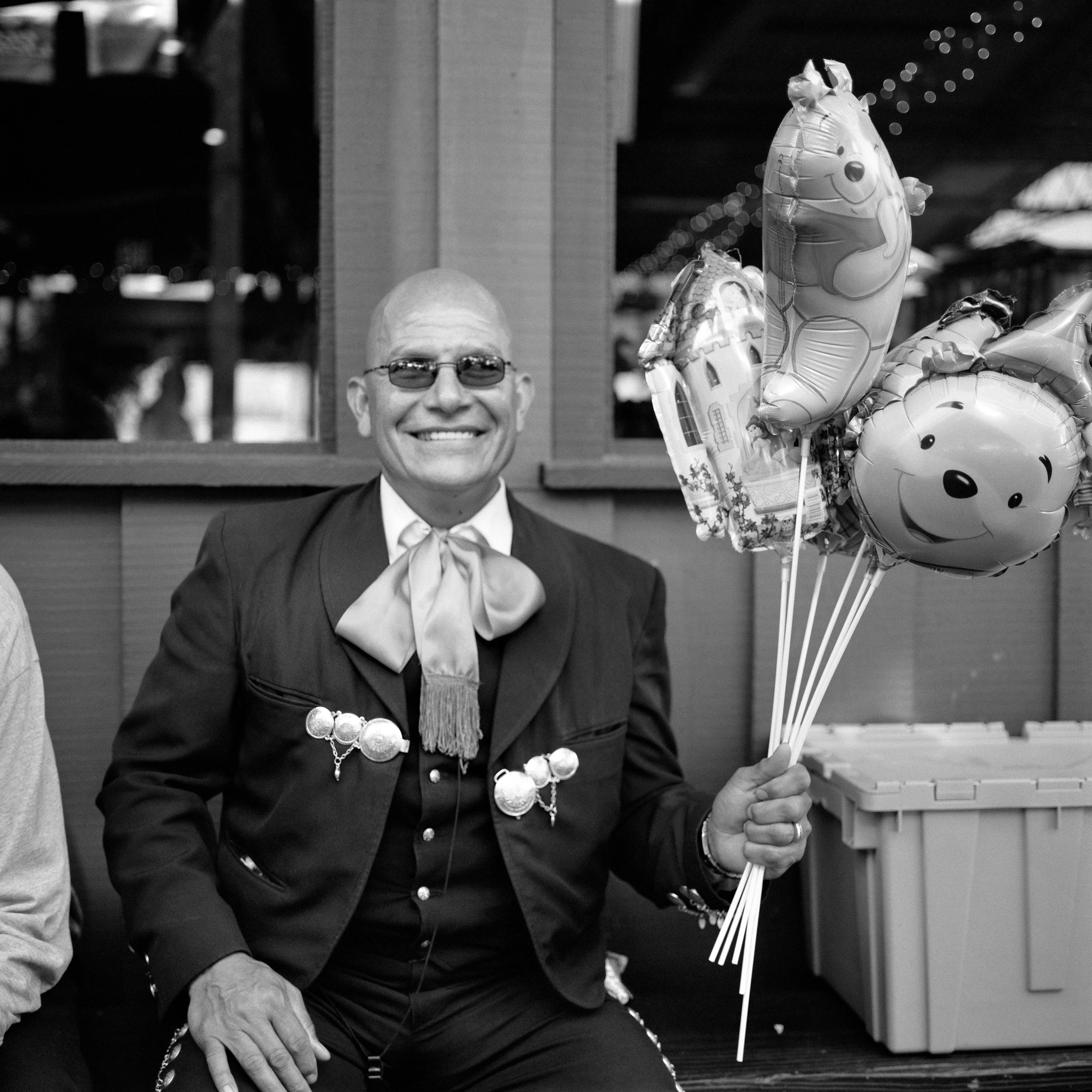 THE VILLAGE #34 MARIACHI HOLDING BALLOONS by Deanna Templeton

This project started in 2002. A year after my mother passed away, a few years after my father passed. What I remember was one day I was thinking about my parents and feeling a little bit lonely, a little empty and decided to go for a drive. So I decided to drive out to my grandmother's house in San Pedro, which is about a 45 minute drive from where I live. I just wanted to reminisce, to re-explore the surroundings where I would go when I was a child. The liquor store I would walk to to get a Lipton Ice Tea and a bag of Frito’s, to the bakery where I swore all the cookies didn’t have sugar in them and then I drove over to Ports O’Call Village. As soon as I started to walk around I came across a stage with some Mariachis playing and it just hit me, I felt like I was home, I was with family. Over the next 5 years, whenever I could, I started going out there on the weekends. Getting reacquainted with the village and the locals. To shoot everything I wanted to remember.

Edition: 1 of 1

Commissioned by Obscura