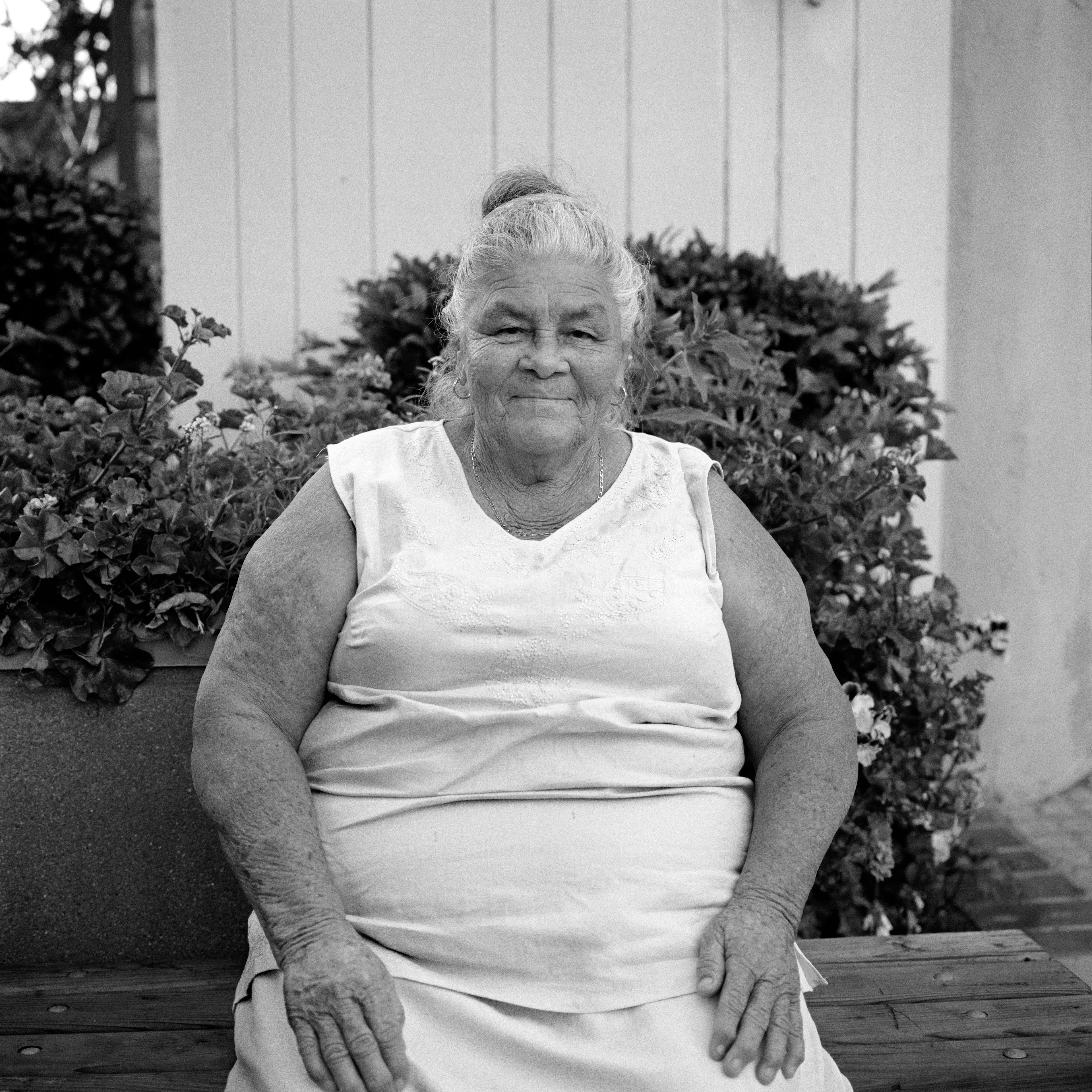 THE VILLAGE #37 PORTRAIT OF AN OLDER WOMAN IN TANK TOP by Deanna Templeton

This project started in 2002. A year after my mother passed away, a few years after my father passed. What I remember was one day I was thinking about my parents and feeling a little bit lonely, a little empty and decided to go for a drive. So I decided to drive out to my grandmother's house in San Pedro, which is about a 45 minute drive from where I live. I just wanted to reminisce, to re-explore the surroundings where I would go when I was a child. The liquor store I would walk to to get a Lipton Ice Tea and a bag of Frito’s, to the bakery where I swore all the cookies didn’t have sugar in them and then I drove over to Ports O’Call Village. As soon as I started to walk around I came across a stage with some Mariachis playing and it just hit me, I felt like I was home, I was with family. Over the next 5 years, whenever I could, I started going out there on the weekends. Getting reacquainted with the village and the locals. To shoot everything I wanted to remember.

Edition: 1 of 1

Commissioned by Obscura