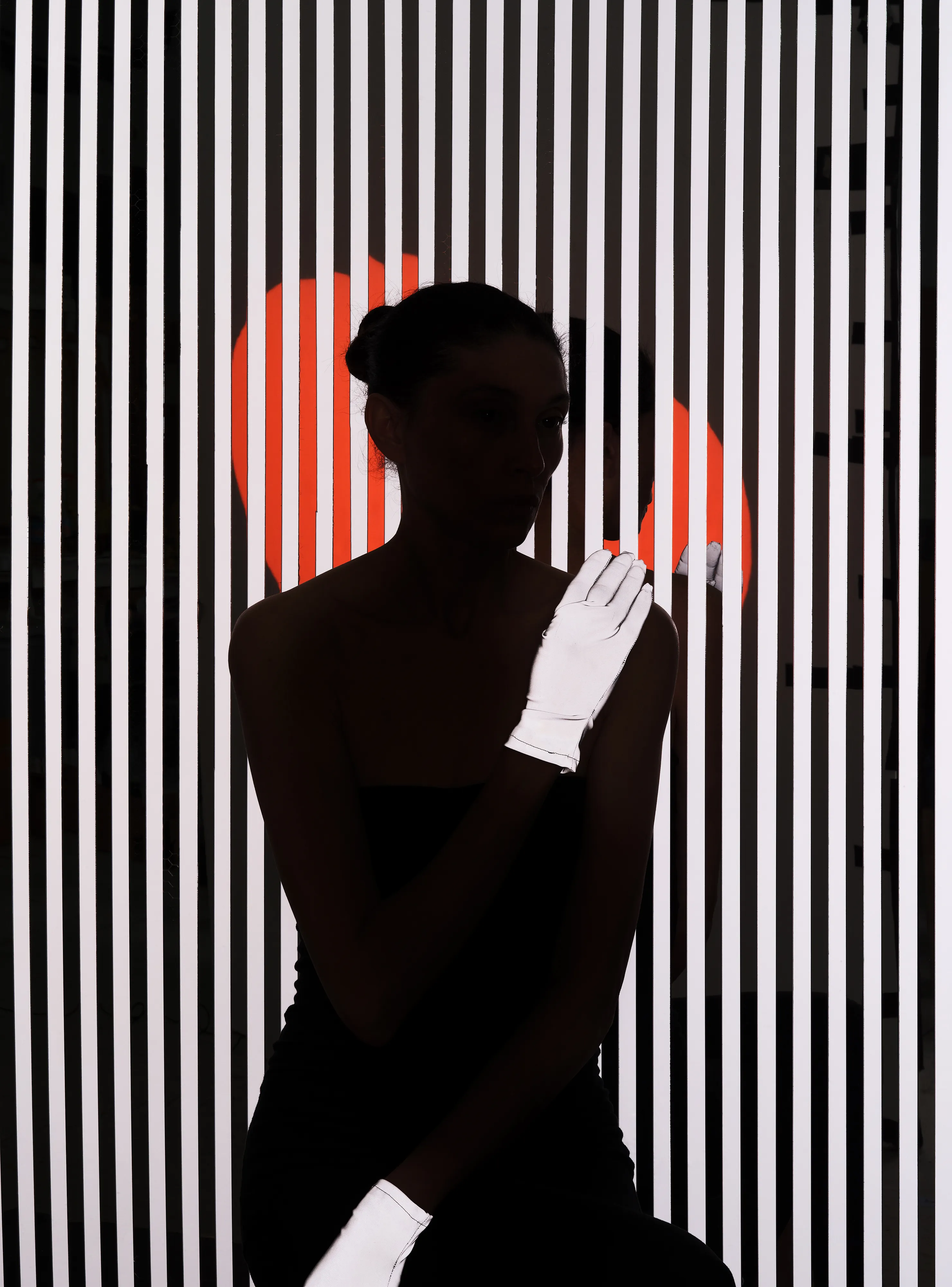 Ursula 3 #42 by Hannah Whitaker

This collection of photographs expands on a character who has been the focal point of my work for a few years: Ursula. I leave ambiguous exactly who and what she is. Her nature is something between an AI, a fictional character, an avatar, a product of the collective imagination, and a living, fully dimensional, being. 

I have previously made two bodies of work with her. The first I published with Image Text Ithaca Press in a book called Ursula. These photographs also comprise my genesis NFT drop. The second I showed recently at Galerie Christophe Gaillard in Paris in an exhibition called Shadow Detail. This third body of work is the first made specifically for the NFT space. I’m calling it Ursula 3, as the third iteration of the project, and in a nod to Web3.

These photographs incorporate some of the photographic techniques that I have used in the past in cultivating the mystique of Ursula—silhouettes, special effect lighting, and printed backgrounds. For Ursula 3 I combined these techniques with a more hands-on approach to set building. I had several props and set materials fabricated out of mirrored plexi, including patterned screens, Ursula’s profile, and her hands. I also had made a turtleneck, gloves, and hoods in reflective materials. In addition to using these props, I incorporated rear projection, a technique used in a pre-digital era of Hollywood filmmaking. 

The sets are more complex than I had done previously, with the intent of making the space in the photographs stranger, more layered, and more difficult to decipher. The resulting photographs evoke the established language of the Ursula lineage but usher her into an increasingly synthetic universe.

Edition: 1 of 1

Commissioned by Obscura