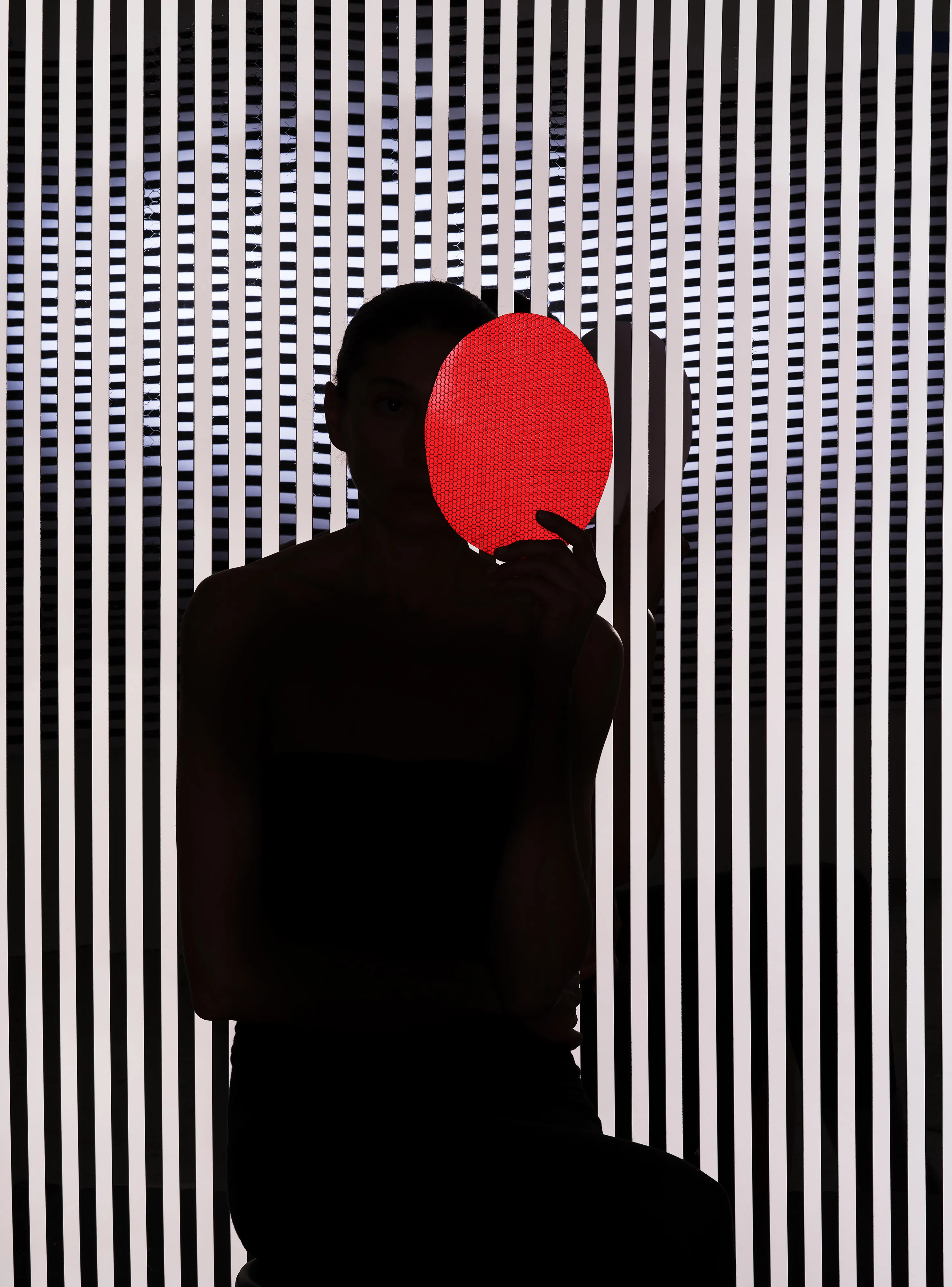 Ursula 3 #28 by Hannah Whitaker

This collection of photographs expands on a character who has been the focal point of my work for a few years: Ursula. I leave ambiguous exactly who and what she is. Her nature is something between an AI, a fictional character, an avatar, a product of the collective imagination, and a living, fully dimensional, being. 

I have previously made two bodies of work with her. The first I published with Image Text Ithaca Press in a book called Ursula. These photographs also comprise my genesis NFT drop. The second I showed recently at Galerie Christophe Gaillard in Paris in an exhibition called Shadow Detail. This third body of work is the first made specifically for the NFT space. I’m calling it Ursula 3, as the third iteration of the project, and in a nod to Web3.

These photographs incorporate some of the photographic techniques that I have used in the past in cultivating the mystique of Ursula—silhouettes, special effect lighting, and printed backgrounds. For Ursula 3 I combined these techniques with a more hands-on approach to set building. I had several props and set materials fabricated out of mirrored plexi, including patterned screens, Ursula’s profile, and her hands. I also had made a turtleneck, gloves, and hoods in reflective materials. In addition to using these props, I incorporated rear projection, a technique used in a pre-digital era of Hollywood filmmaking. 

The sets are more complex than I had done previously, with the intent of making the space in the photographs stranger, more layered, and more difficult to decipher. The resulting photographs evoke the established language of the Ursula lineage but usher her into an increasingly synthetic universe.

Edition: 1 of 1

Commissioned by Obscura