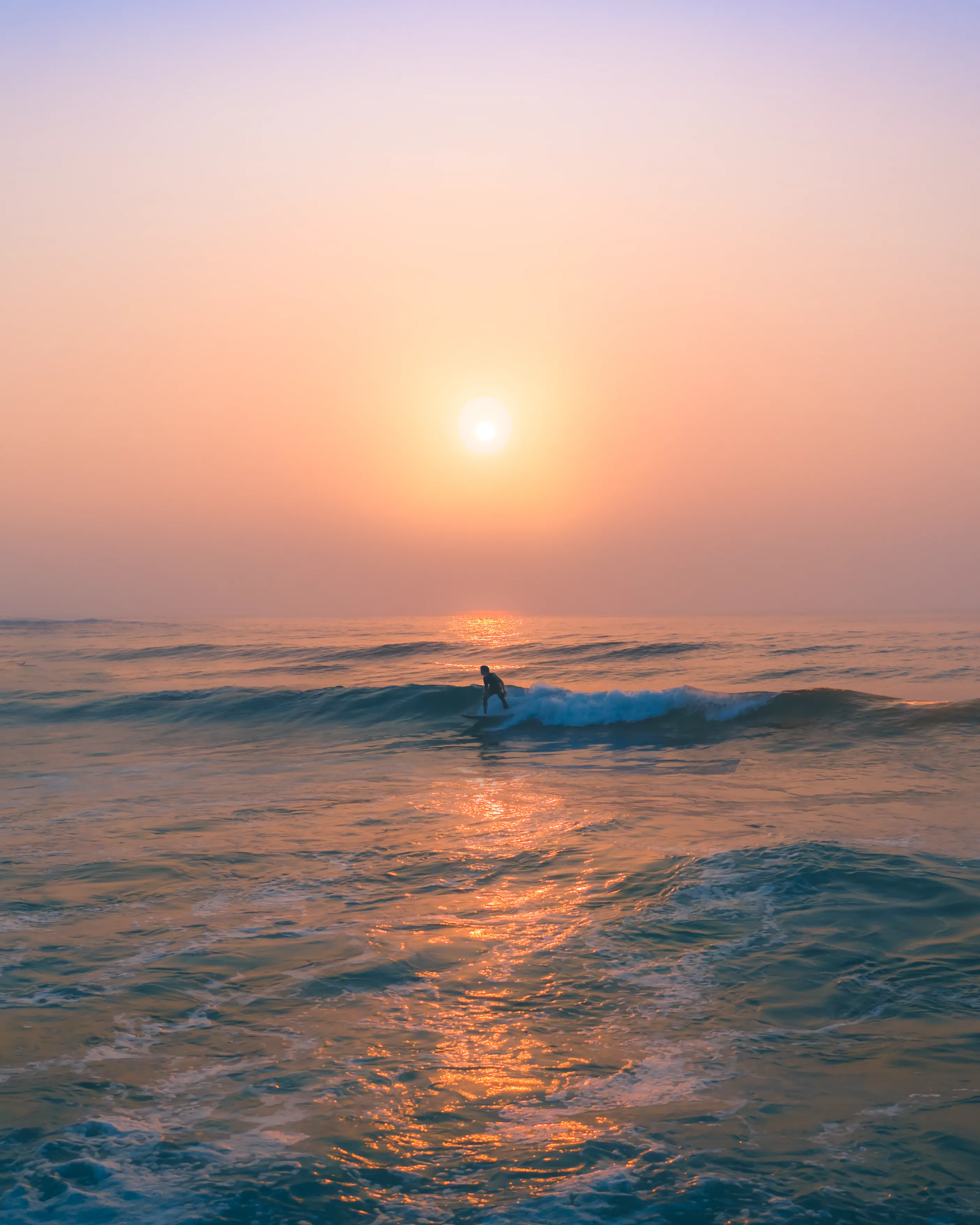 What do bushfires and surfing have in common? In the second half of 2019, Australia's east coast and inland bushland was on fire for nearly six months straight. This meant that thick smoke travelled thousands of kilometres and hung around for months. Breathing was difficult and going outdoors was mostly avoided.

Surfers everywhere soldiered on, including myself. My daily ritual of capturing images at sunrise was made difficult by the thick clouds of toxic smoke, limiting both breathing as well as the usual golden light reaching the shore.

There were a few days during this time where I was able to capture magic. The rising sun was engulfed in a beautiful hazy cloud, that created these incredibly surreal, diffused pastel colours and gradients.

Getting these images and then paddling out for some waves was hard, however, not doing it was harder. I am grateful I made the choice to get after it in these conditions, as we then entered lockdown shortly after this bushfire event. 

This image will forever serve as a reminder to do the things that give you strength and peace, no matter the circumstances and to always be grateful for the chance to do so.

Artist: New Light Visuals  

Title: Ocean Ablaze 
 
Edition: 1/25