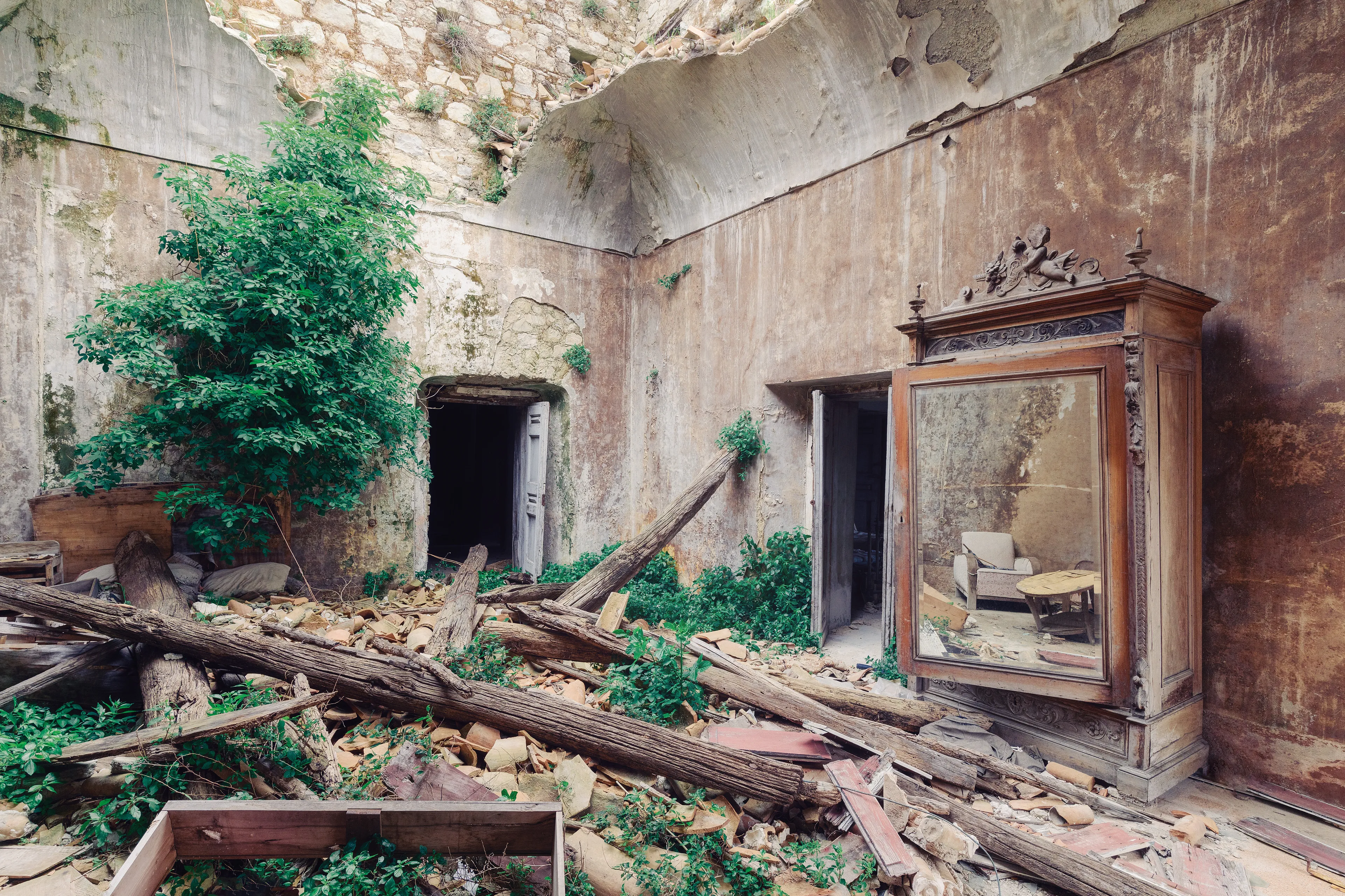 Almost 2 decades ago an earthquake destroyed the old village and its palace.

This old living room is a silent and interesting witness of the fateful event.

While a large hole gapes in the ceiling, on the left a tree is already growing towards the sky, on the right stands the almost undamaged old wooden mirror cabinet. This in turn reveals a view of other legacies