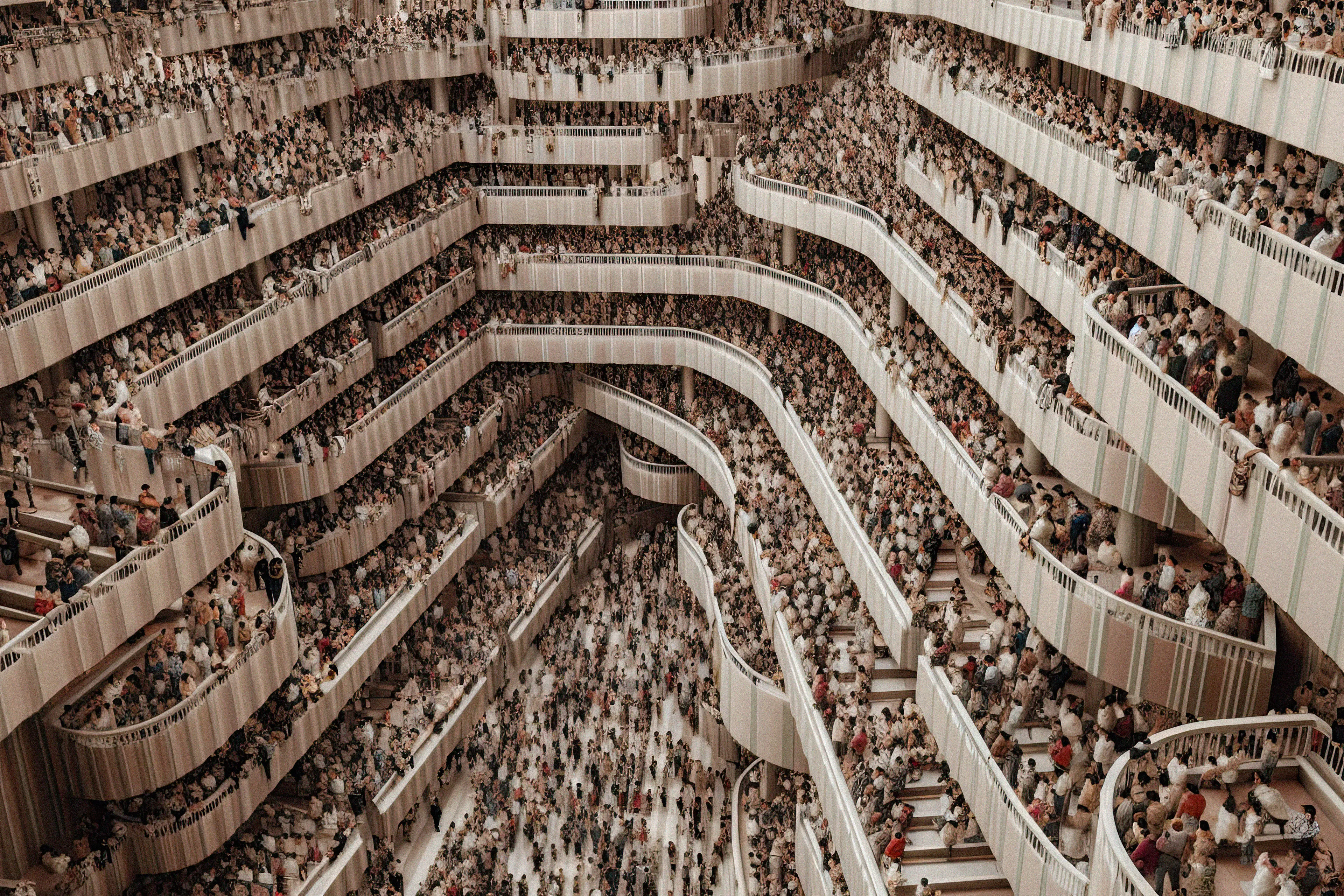 "Overpopulated Symphonies" is a collection of AI post-photography that immerses viewers in a commentary on the contemporary human condition. Through sprawling images of densely populated urban landscapes and human gatherings, the collection reduces individuals to minuscule points, forming an overwhelming sea of indistinguishable dots.

Beyond the literal portrayal of overpopulation, this collection utilizes the metaphor of crowd density as an analogy for the inundation of information in our modern era. It poses questions about identity, individuality, and the struggles faced by the human mind in processing and prioritizing the relentless surge of data we encounter daily. The figures in these photographs transcend mere physical bodies; they represent thoughts, ideas, and information, all vying for recognition and space within the confines of our mental landscapes. With humans depicted as dots in a chaotic neural network, these artworks serve as an allegory for the phenomenon of information overload.

The title "Overpopulated Symphonies" intends to evoke the intricate and often overwhelming nature of our current reality. "Overpopulated" alludes to the physical density of human gatherings depicted in the collection, but also metaphorically refers to the overflow of information and ideas that bombard us incessantly. The term "Symphonies" suggests a sense of harmony and order, offering an optimistic counterpoint to the chaos portrayed. It hints at the potential for synchronicity to arise from apparent disarray.