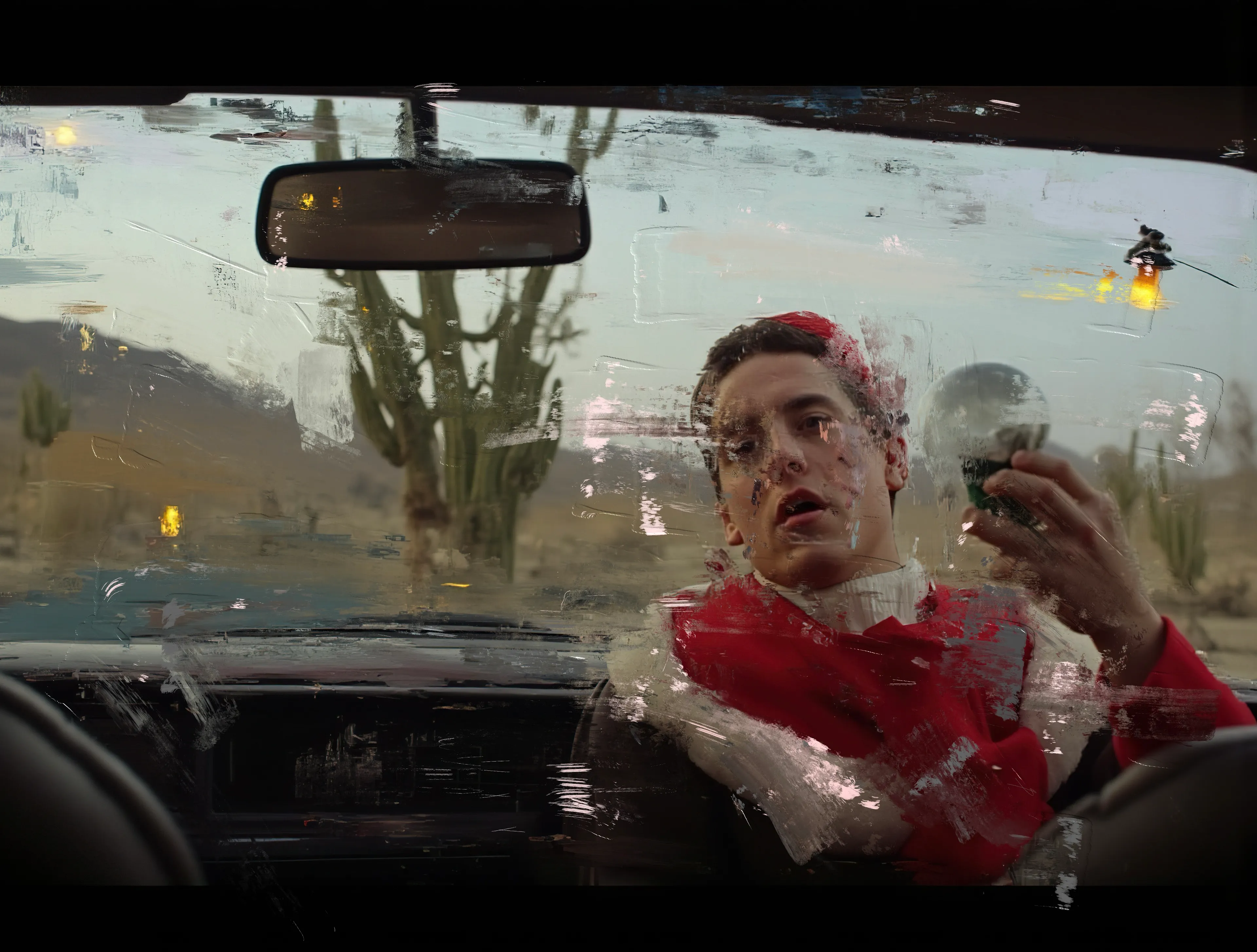 The desert stretches forever, pale and mute,
Where cacti stand like sentinels—silent and judgmental.
The man in red spins the glass orb in his hand,
A snowstorm trapped inside,
Swirling as if it knows something he doesn’t.

The rearview mirror hangs crooked,
Reflecting nothing but dust and dead roads,
While sunlight slinks through the cracks,
Soft, indifferent, too clean for what’s happening here.

His face is painted in hues of resignation,
Jaw slack, eyes caught somewhere
Between a question and a plea—
Where the line between fever dream and last chance
Grows razor thin.

The car feels heavier than the silence it carries,
An engine of exile with no destination.
Outside, the cacti mock him—
The kind of stillness that tells you to run.

But he doesn’t.
Instead, he clutches the snow globe tighter,
Watches the flakes fall like lost time,
And wonders if maybe the world
Always looked better behind glass.