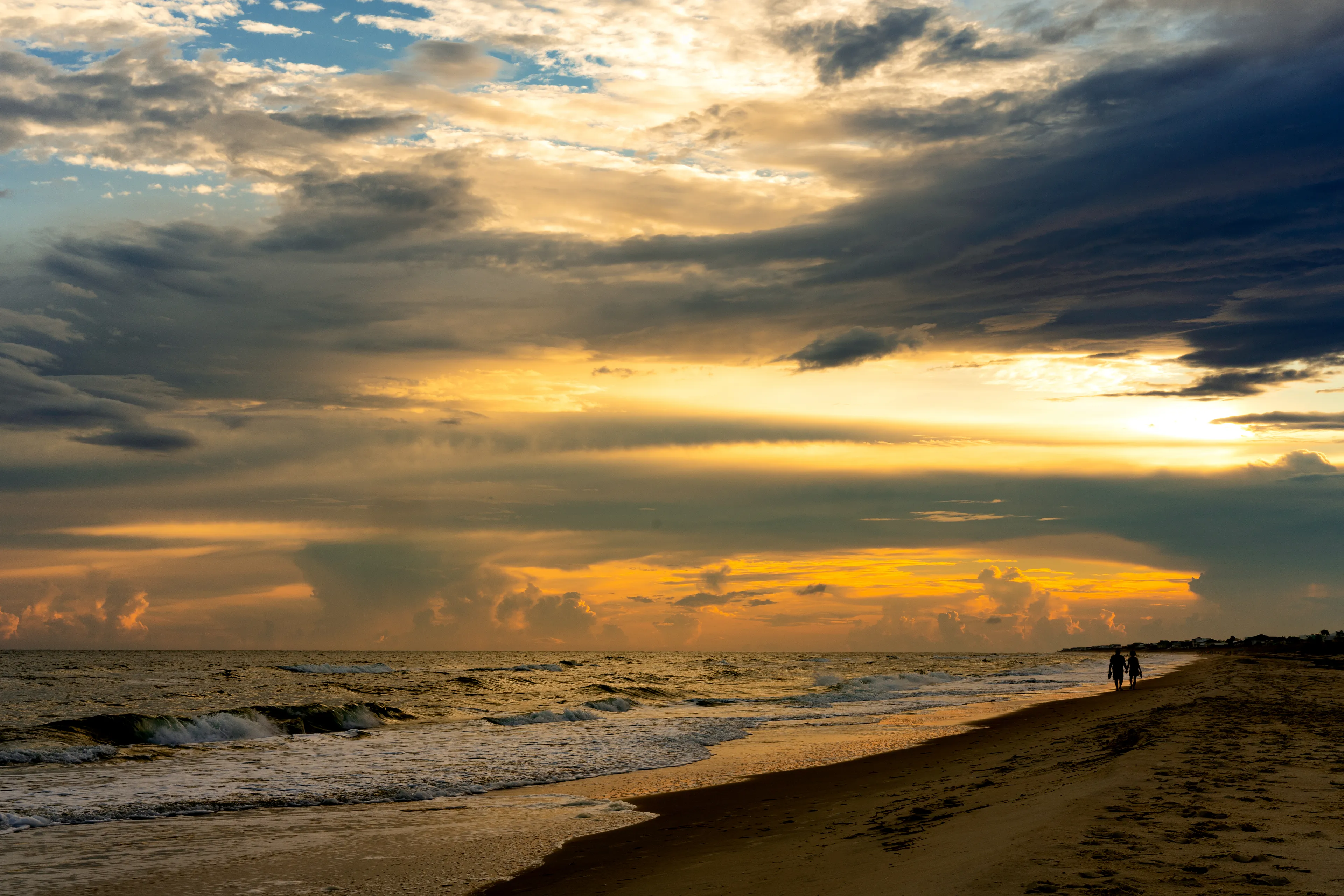 Lone couple walking on the beach at sunset.