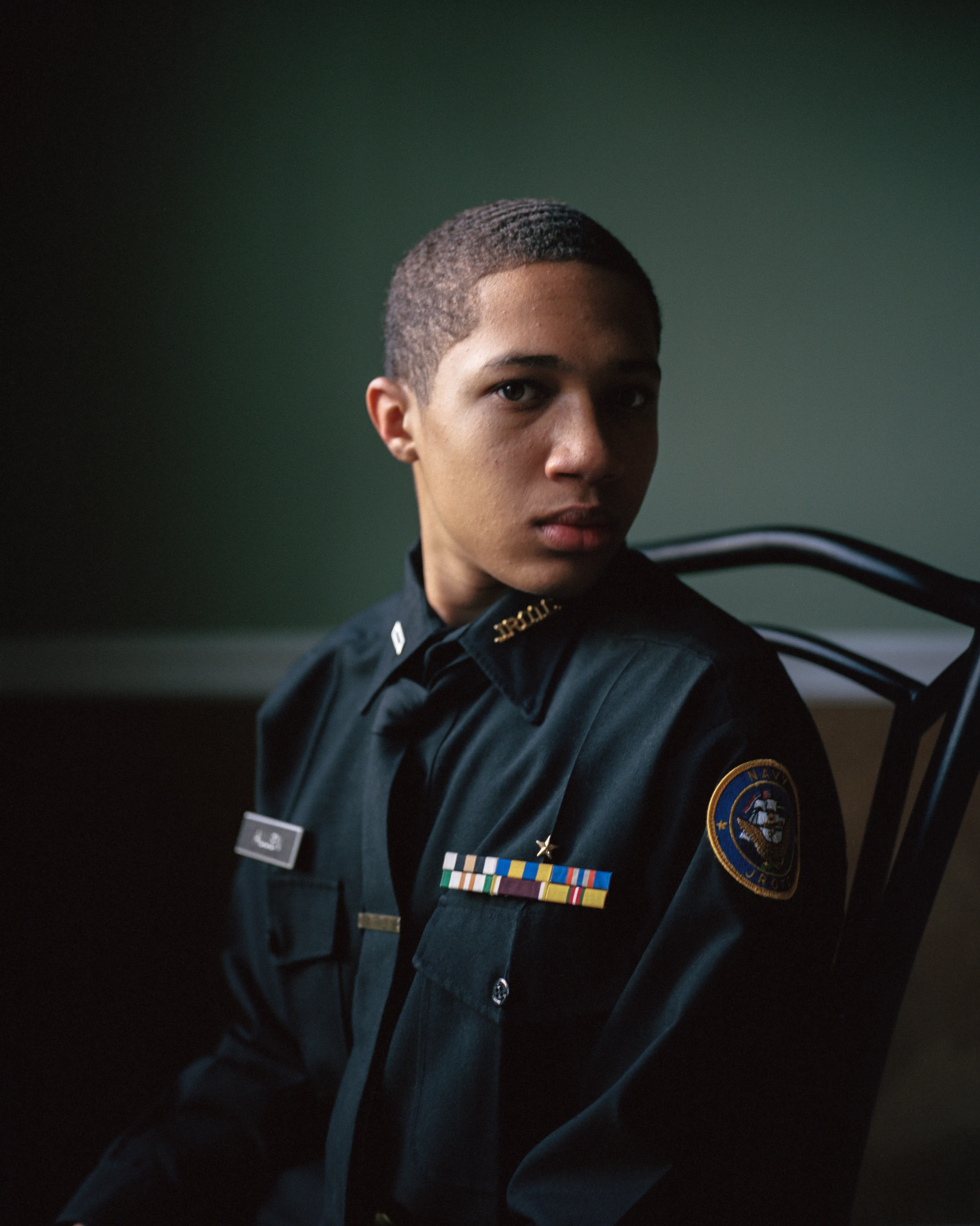 Right before I made the first image of Sharrod, when he went to his bedroom to change, his mother turned to me and said, “Whenever he puts on his uniform, I no longer see my son.”

In the winter of 2008 I met Sharrod, who was in his first year of high school and had recently enrolled in National Junior Reserve Officer’s Training Corps (NJROTC), a military preparatory program offered in high schools nationwide. After explaining my connection to the military and that I was an alum of the same high school that both Sharrod and his mother attended, I asked if I might photograph Sharrod from his freshman to senior year (2008-2012). They both agreed and over the course of the next four years, Sharrod played out his military fantasies for my camera. Sharrod also shared with me the photographs he was making with his cell phone and notebook doodles of weapon construction. These private images and examinations rub up against, color, and compliment the medium format images I’ve made providing the viewer a fuller image of Sharrod’s journey.

Over the course of making the images and video installations for "I slowly watched him disappear," I wondered about the process within which the military body is formed both literally but also psychologically, visually, and emotionally. What is the process of indoctrination and how does the heavy flow of military marketing messages — specifically in military towns— foreclose possibilities for a life beyond the uniform? Furthermore, can one photographically locate the transition from civilian to member of the military unit? 

"I slowly watched him disappear" is the first part of a multimedia “essay” including photographs, video installations, nonfiction films, curatorial projects, and texts which organize my meditations on the fantasy, construction, and deconstruction of the military body and its effects on the broader culture.  