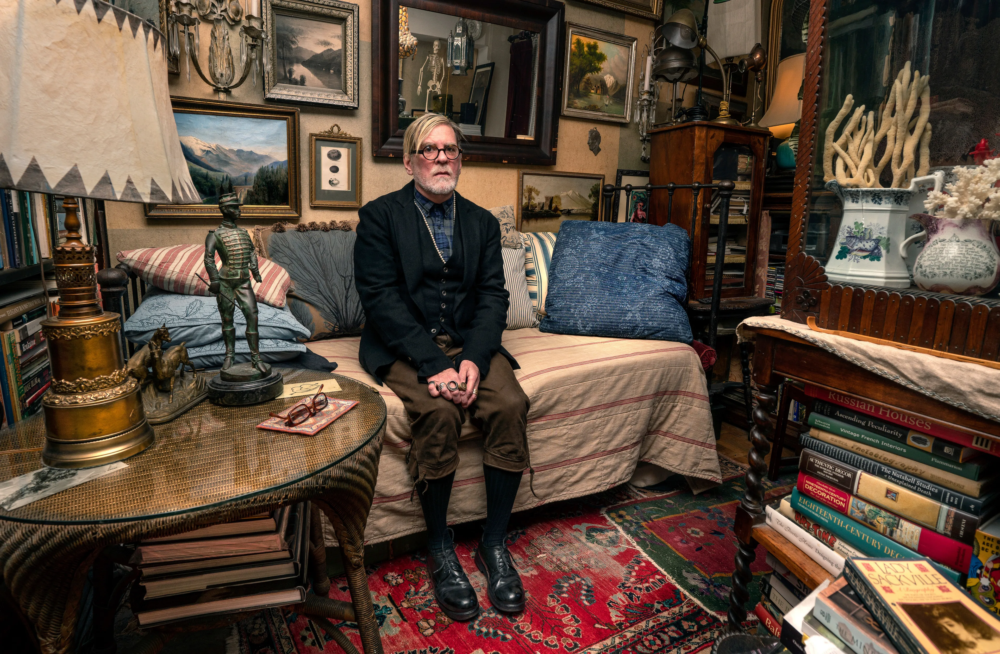 For the past 30 years, Sally Davies has been documenting the streets of Manhattan. She’s watched neighborhoods negotiate with gentrification, post-9/11 anxiety, economic uncertainty, and a steady stream of “if I can make it there, I’ll make it anywhere” optimism. Davies has taken memorable photographs of ordinary doorways, wet curbs and corners, the glow of bar-grill signs, bodegas, bakery windows, wheelchairs on rooftops, incoming weather, graffiti, and vintage cars. As she has said, “You either fall in love with moonlight on a garbage bag or you hate it and move along.”*

Davies started the New Yorkers by shifting from her usual view of the urban outdoors to the idea of chronicling the spaces and stories of the natives and transplants who give the city its particular vitality. 

In these portraits, you will meet waitresses, musicians, cab drivers, painters, teachers, shopkeepers, writers, designers, producers, parents, a gossip columnist, and a psychic to the stars, among others. They are singularly sensational, and they attest to multiple jobs, friendships, marriages, divorces, children, and pets. Young and old, straight and gay, casual and formal; they pose in cramped kitchens and elegant living rooms, laying on beds, sitting in bathtubs, surrounded by the surfaces and souvenirs of living. There is an abundance of brick, wood, leather, and metal, and collections of refrigerator magnets, religious and street art, books, Pez dispensers, vinyl records, and plants.

These photographs and texts speak to what all New Yorkers understand—to live in this city is to embrace struggle, sacrifice, love, and change. When I spoke with Davies over breakfast in February 2020, I asked her what this project reveals. She said, “This is the end of an era.” That comment has returned to me repeatedly. This book went to print during a pandemic that stopped the world as we knew it. We were in our homes for hours on end, adapting to new habits, while thinking and feeling deeply about where and how we live. These New York people were right on time.

by Stuart Horodner
*Sally Davies in Michael Ernest Sweet’s “Photographer Sally Davies Discusses Women Street Photographers,” HuffPost (December 15, 2015) 

Photographed at his home in Stuyvesant Town on November 2, 2019.