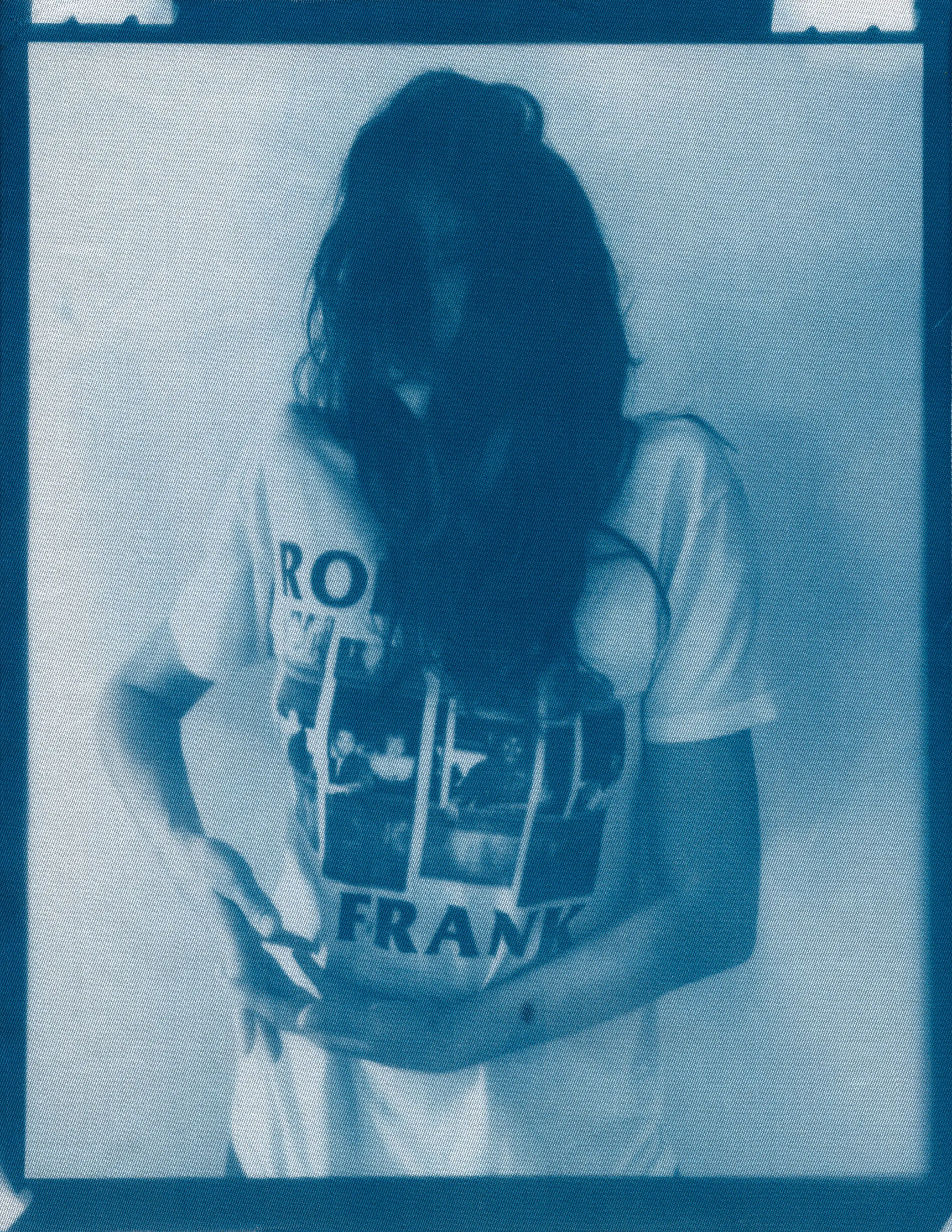 In the spring of 2020, panic surrounding COVID-19 erupted and mandatory shelter in place orders went into effect, forcing me to abandon long-planned portrait shoots, travel, and work in progress in my art studio.  I found myself in a 340 sq ft apartment in a Bay-area neighborhood that was emptying by the day.  The buzzing silence was profound. Two weeks into isolation, my drive to connect with others and make portraits only amplified.  With no safe way to do so, I spontaneously turned the camera on myself to create a portrait.  I printed it as a cyanotype, a simple nineteenth century photographic process that was only feasible due to the basic materials I happened to have on hand—a budget printer, transparency film and a package of fraying sheets of cotton pretreated with cyanotype chemicals.  At first, I exposed the prints in the unpredictable spring sunlight coming through my third floor apartment window.  As the seasons changed, I went on to make them in a garden, on the top of a car, or a patch of wobbly concrete tiles.  I rinsed them in water and varying shades of blue emerged.  I created a daily self-portrait using this technique for more than a year. 

I made most of these self-portraits inside various studio apartments that I lived in alone.  To make the earliest pictures in the series, I had to move a couch every day to create space against a white wall near a window.  I took others in fleeting spaces while traveling—in a guest room, in a medical examination room, during a pause in the wilderness, and later against the wall of an old California bungalow sandwiched between the mountains and the sea.  In the beginning, I often tried to cover as much of my body and face as possible as a commentary on my fear of the virus and my efforts to guard against it.  My armor and props ranged from common household items—potholders, tinfoil, dish towels, bedsheets, and toilet paper— to more telling evidence of the unusual consumption that resulted from being stuck indoors indefinitely— Amazon packaging, takeout bags and trash leftover from groceries purchased while wearing rubber gloves and sterilized in whatever way  was possible and later consumed.  These items shifted as the duration of the pandemic blurred into an unknown stretch of time. The portraits became less about those initial fears and more about confronting the boredom, anxiety, grief, and fatigue of living in indefinite isolation during a global pandemic. 

In total, I made these portraits for 377 consecutive days.  I made the first portrait on March 30th, 2020, a day when my head was raging in pain, my throat was constricted, and the fear that I might have contracted COVID hung over me before testing was easily accessible.  I made the last portrait on April 10th, 2021, the day I received my 2nd vaccination.  The days, weeks, and months in between feel like a fever dream—frayed and flickering in multitudes of blue.

2021_0104