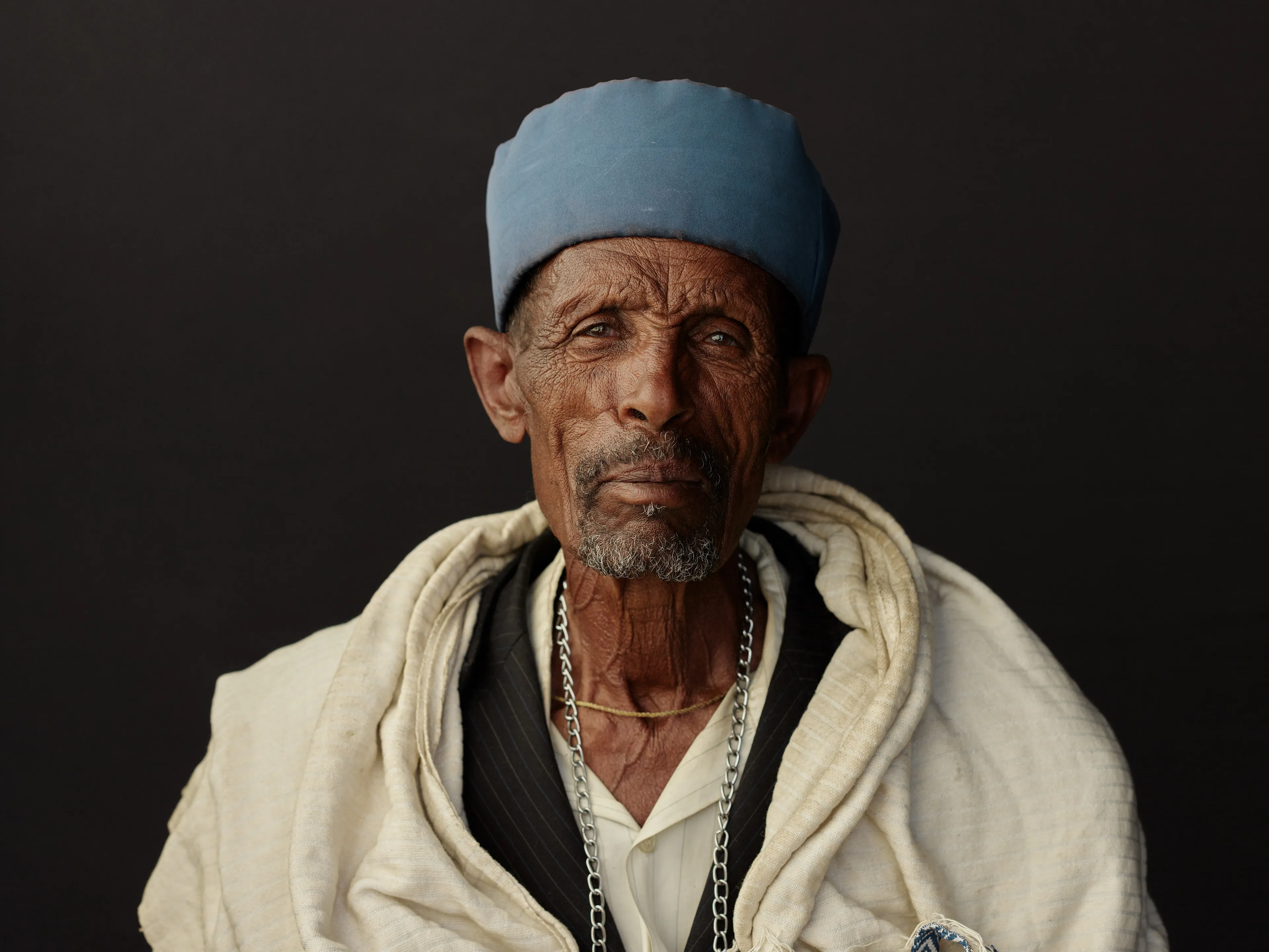Joey L. returns to Quantum with Ethiopia - Portraits: a collection directly linked to his genesis drop during Season 1. For every environmental image from Joey’s first drop, there is a portrait companion.

“For years, we dragged our nomadic studio tent across almost every region of Ethiopia. In our tent, everyone was equal. We captured pure magic. Every kind of person entered and had their portrait taken. The tent was our little fantasy world. It was the Ethiopia that we dreamed of, even when the reality outside of it was sometimes stricken with searing pain. Each portrait was a tribute to a distinct region of the country. Disconnected cultural threads were woven together in a cohesive visual style in order to truly see Ethiopia— which itself is a modern nation state, but is also the sum of all the diverse people who inhabit it.”

Joey’s portraits alternating on red and black backdrops are the visual backbone of my forthcoming book “Ethiopia” (Insight Editions, January 2023), which compiles 13 years of work.

The tent itself is a metal frame modified with diffusion material made out of netela fabric, which is a hand-spun cotton perfected by Dorze craftspeople. Every portrait is created with natural light molded from the tent itself and photographed on location.

Lalibela, Amhara Region, Ethiopia 
January 2021