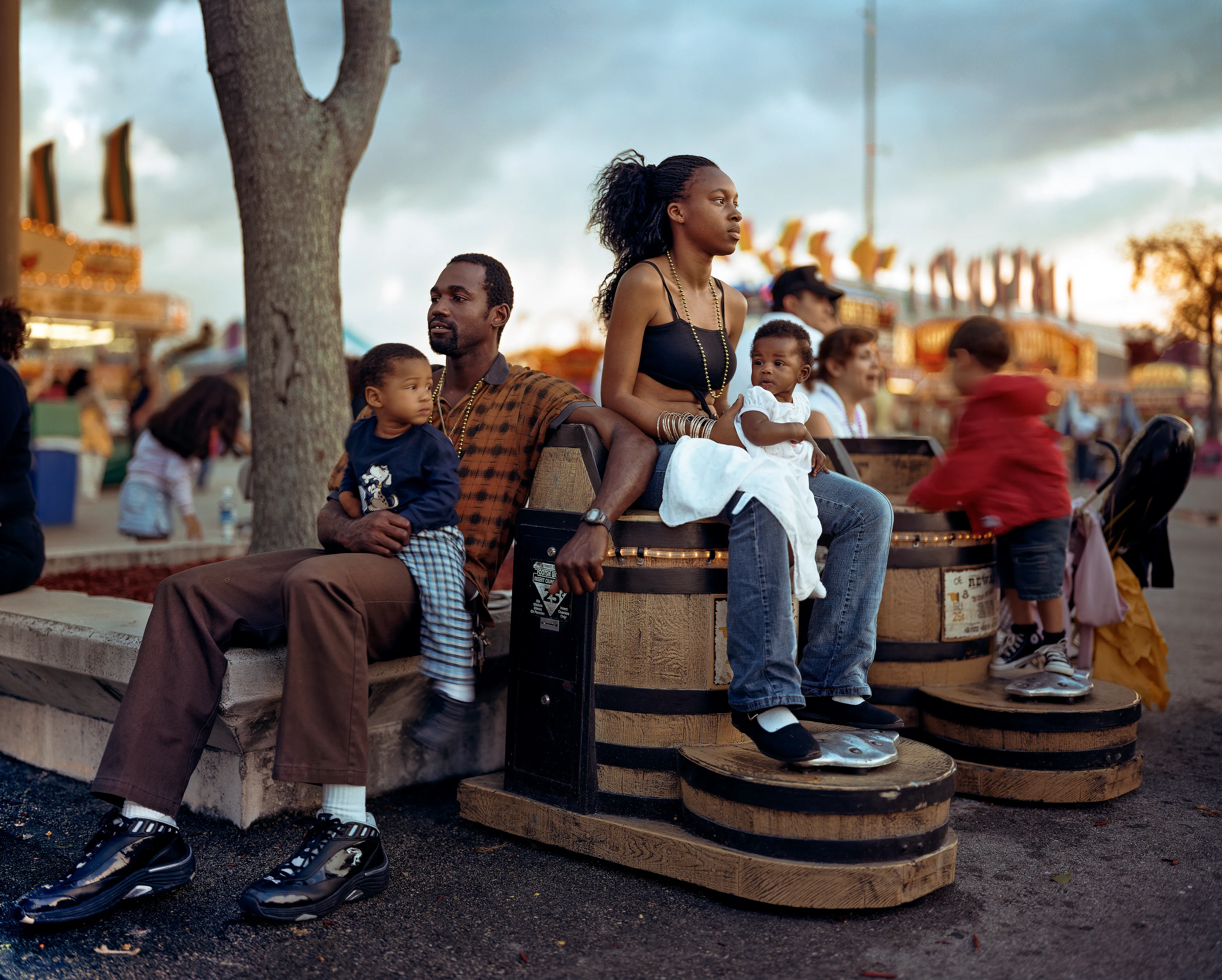 County fairs conjure ideas of tilt-a-whirls, stuffed animals, cotton candy, and blue ribbons. Rooted in local agricultural practices, fairs have been a ubiquitous part of American life for two centuries. In a reassuring way, they seem impervious to economic, technological, or fashion trends. For better or for worse, fairs look the same through the decades.

Though they are places to meet each other, there sure is a lot of loneliness at the fair. The series County Fair captures that duality: an adolescent boy looks up at the woman working the Hot Dog on a Stick stand as if she were a museum diorama; a little red haired girl haltingly befriends a robot; young couples, leaning and draped over each other, hide from the world in plain sight.


In my pictures, the dizzying atmosphere, colorfully decorated to provide amusement and distraction, is imbued with sadness and longing. These feelings, which permeate society, are laid bare at the fair. Sadness and longing circulate, intersect and incubate in the confined space between the ticket booths and the craft barns. People come out to participate and show, to see and be seen. Ultimately, connection remains elusive. 

