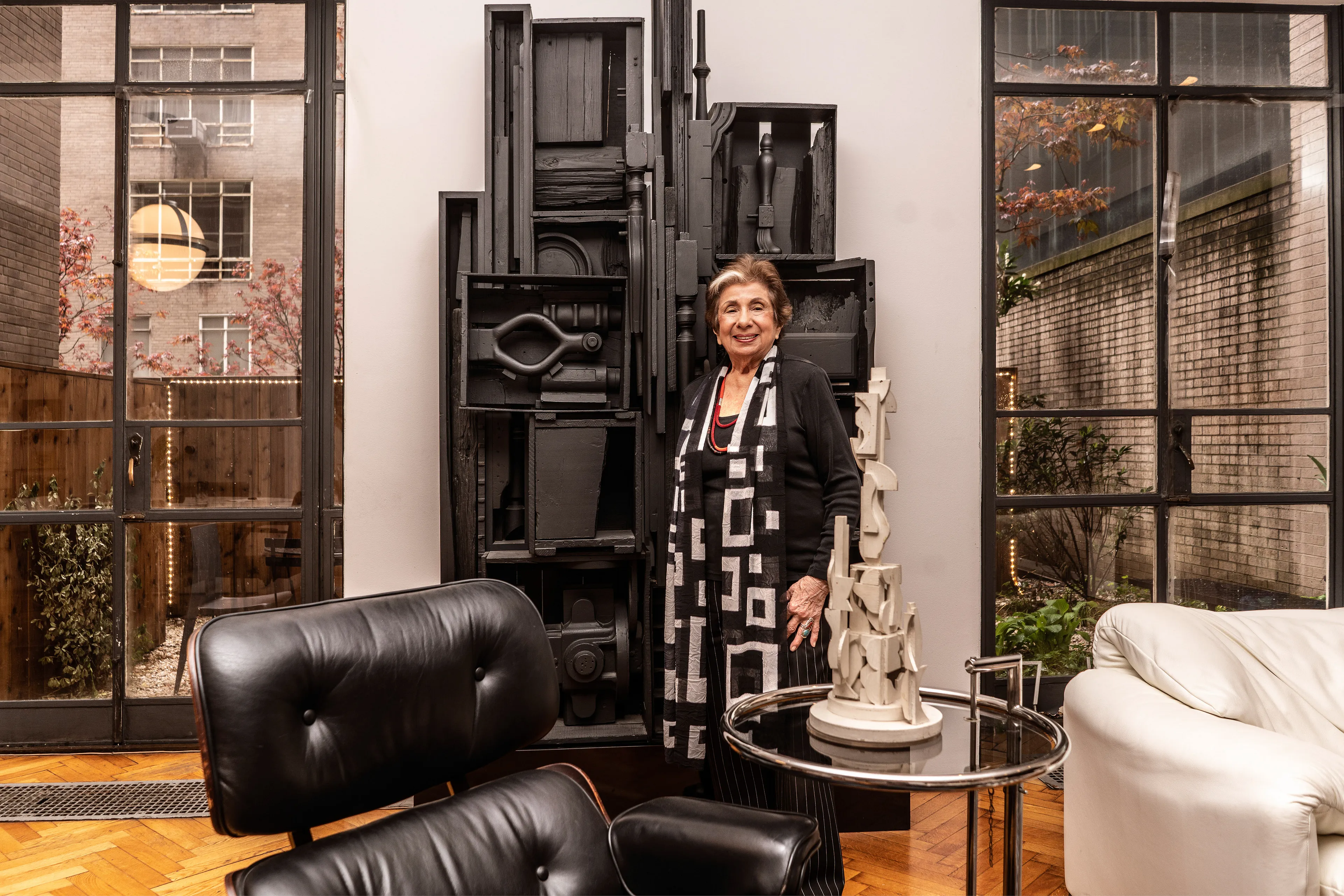 For the past 30 years, Sally Davies has been documenting the streets of Manhattan. She’s watched neighborhoods negotiate with gentrification, post-9/11 anxiety, economic uncertainty, and a steady stream of “if I can make it there, I’ll make it anywhere” optimism. Davies has taken memorable photographs of ordinary doorways, wet curbs and corners, the glow of bar-grill signs, bodegas, bakery windows, wheelchairs on rooftops, incoming weather, graffiti, and vintage cars. As she has said, “You either fall in love with moonlight on a garbage bag or you hate it and move along.”*

Davies started the New Yorkers by shifting from her usual view of the urban outdoors to the idea of chronicling the spaces and stories of the natives and transplants who give the city its particular vitality. 

In these portraits, you will meet waitresses, musicians, cab drivers, painters, teachers, shopkeepers, writers, designers, producers, parents, a gossip columnist, and a psychic to the stars, among others. They are singularly sensational, and they attest to multiple jobs, friendships, marriages, divorces, children, and pets. Young and old, straight and gay, casual and formal; they pose in cramped kitchens and elegant living rooms, laying on beds, sitting in bathtubs, surrounded by the surfaces and souvenirs of living. There is an abundance of brick, wood, leather, and metal, and collections of refrigerator magnets, religious and street art, books, Pez dispensers, vinyl records, and plants.

These photographs and texts speak to what all New Yorkers understand—to live in this city is to embrace struggle, sacrifice, love, and change. When I spoke with Davies over breakfast in February 2020, I asked her what this project reveals. She said, “This is the end of an era.” That comment has returned to me repeatedly. This book went to print during a pandemic that stopped the world as we knew it. We were in our homes for hours on end, adapting to new habits, while thinking and feeling deeply about where and how we live. These New York people were right on time.

by Stuart Horodner
*Sally Davies in Michael Ernest Sweet’s “Photographer Sally Davies Discusses Women Street Photographers,” HuffPost (December 15, 2015) 

Photographed at her home near the Museum of Modern Art, with her Louise Nevelson sculpture,
on April 26, 2019.