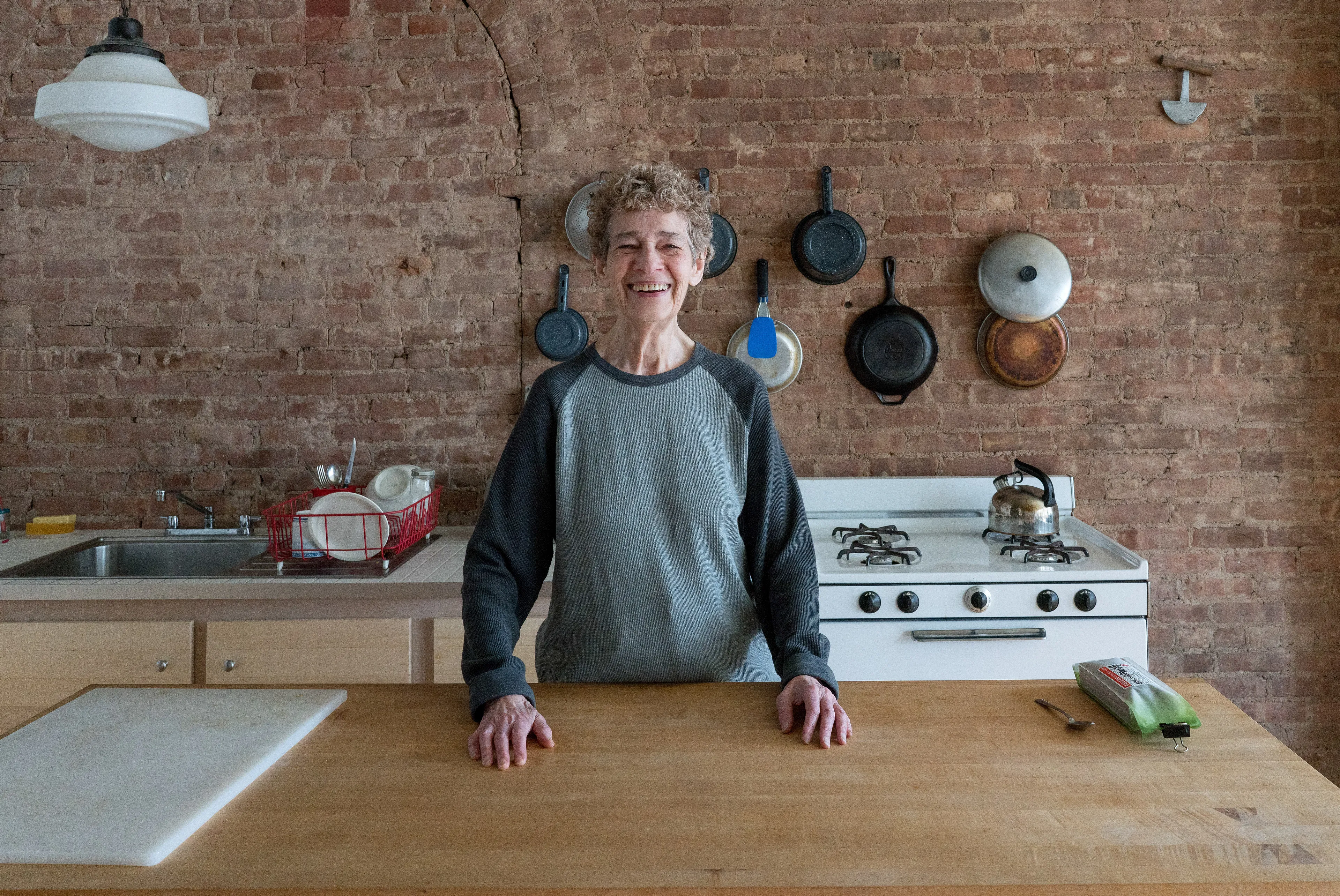 For the past 30 years, Sally Davies has been documenting the streets of Manhattan. She’s watched neighborhoods negotiate with gentrification, post-9/11 anxiety, economic uncertainty, and a steady stream of “if I can make it there, I’ll make it anywhere” optimism. Davies has taken memorable photographs of ordinary doorways, wet curbs and corners, the glow of bar-grill signs, bodegas, bakery windows, wheelchairs on rooftops, incoming weather, graffiti, and vintage cars. As she has said, “You either fall in love with moonlight on a garbage bag or you hate it and move along.”*

Davies started the New Yorkers by shifting from her usual view of the urban outdoors to the idea of chronicling the spaces and stories of the natives and transplants who give the city its particular vitality. 

In these portraits, you will meet waitresses, musicians, cab drivers, painters, teachers, shopkeepers, writers, designers, producers, parents, a gossip columnist, and a psychic to the stars, among others. They are singularly sensational, and they attest to multiple jobs, friendships, marriages, divorces, children, and pets. Young and old, straight and gay, casual and formal; they pose in cramped kitchens and elegant living rooms, laying on beds, sitting in bathtubs, surrounded by the surfaces and souvenirs of living. There is an abundance of brick, wood, leather, and metal, and collections of refrigerator magnets, religious and street art, books, Pez dispensers, vinyl records, and plants.

These photographs and texts speak to what all New Yorkers understand—to live in this city is to embrace struggle, sacrifice, love, and change. When I spoke with Davies over breakfast in February 2020, I asked her what this project reveals. She said, “This is the end of an era.” That comment has returned to me repeatedly. This book went to print during a pandemic that stopped the world as we knew it. We were in our homes for hours on end, adapting to new habits, while thinking and feeling deeply about where and how we live. These New York people were right on time.

by Stuart Horodner
*Sally Davies in Michael Ernest Sweet’s “Photographer Sally Davies Discusses Women Street Photographers,” HuffPost (December 15, 2015) 

Photographed at her SoHo loft on April 9, 2019.