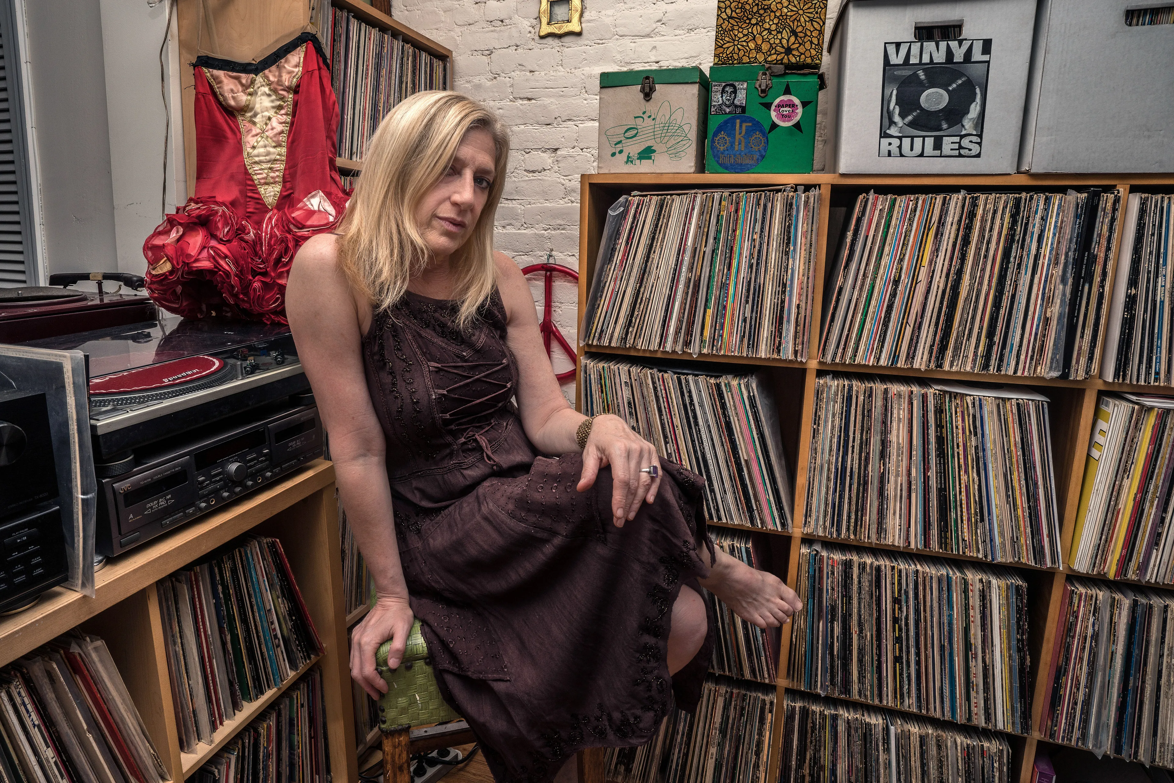 For the past 30 years, Sally Davies has been documenting the streets of Manhattan. She’s watched neighborhoods negotiate with gentrification, post-9/11 anxiety, economic uncertainty, and a steady stream of “if I can make it there, I’ll make it anywhere” optimism. Davies has taken memorable photographs of ordinary doorways, wet curbs and corners, the glow of bar-grill signs, bodegas, bakery windows, wheelchairs on rooftops, incoming weather, graffiti, and vintage cars. As she has said, “You either fall in love with moonlight on a garbage bag or you hate it and move along.”*

Davies started the New Yorkers by shifting from her usual view of the urban outdoors to the idea of chronicling the spaces and stories of the natives and transplants who give the city its particular vitality. 

In these portraits, you will meet waitresses, musicians, cab drivers, painters, teachers, shopkeepers, writers, designers, producers, parents, a gossip columnist, and a psychic to the stars, among others. They are singularly sensational, and they attest to multiple jobs, friendships, marriages, divorces, children, and pets. Young and old, straight and gay, casual and formal; they pose in cramped kitchens and elegant living rooms, laying on beds, sitting in bathtubs, surrounded by the surfaces and souvenirs of living. There is an abundance of brick, wood, leather, and metal, and collections of refrigerator magnets, religious and street art, books, Pez dispensers, vinyl records, and plants.

These photographs and texts speak to what all New Yorkers understand—to live in this city is to embrace struggle, sacrifice, love, and change. When I spoke with Davies over breakfast in February 2020, I asked her what this project reveals. She said, “This is the end of an era.” That comment has returned to me repeatedly. This book went to print during a pandemic that stopped the world as we knew it. We were in our homes for hours on end, adapting to new habits, while thinking and feeling deeply about where and how we live. These New York people were right on time.

by Stuart Horodner
*Sally Davies in Michael Ernest Sweet’s “Photographer Sally Davies Discusses Women Street Photographers,” HuffPost (December 15, 2015) 

Photographed at her home in the East Village, with her vintage Rockettes corset, on June 30, 2019.