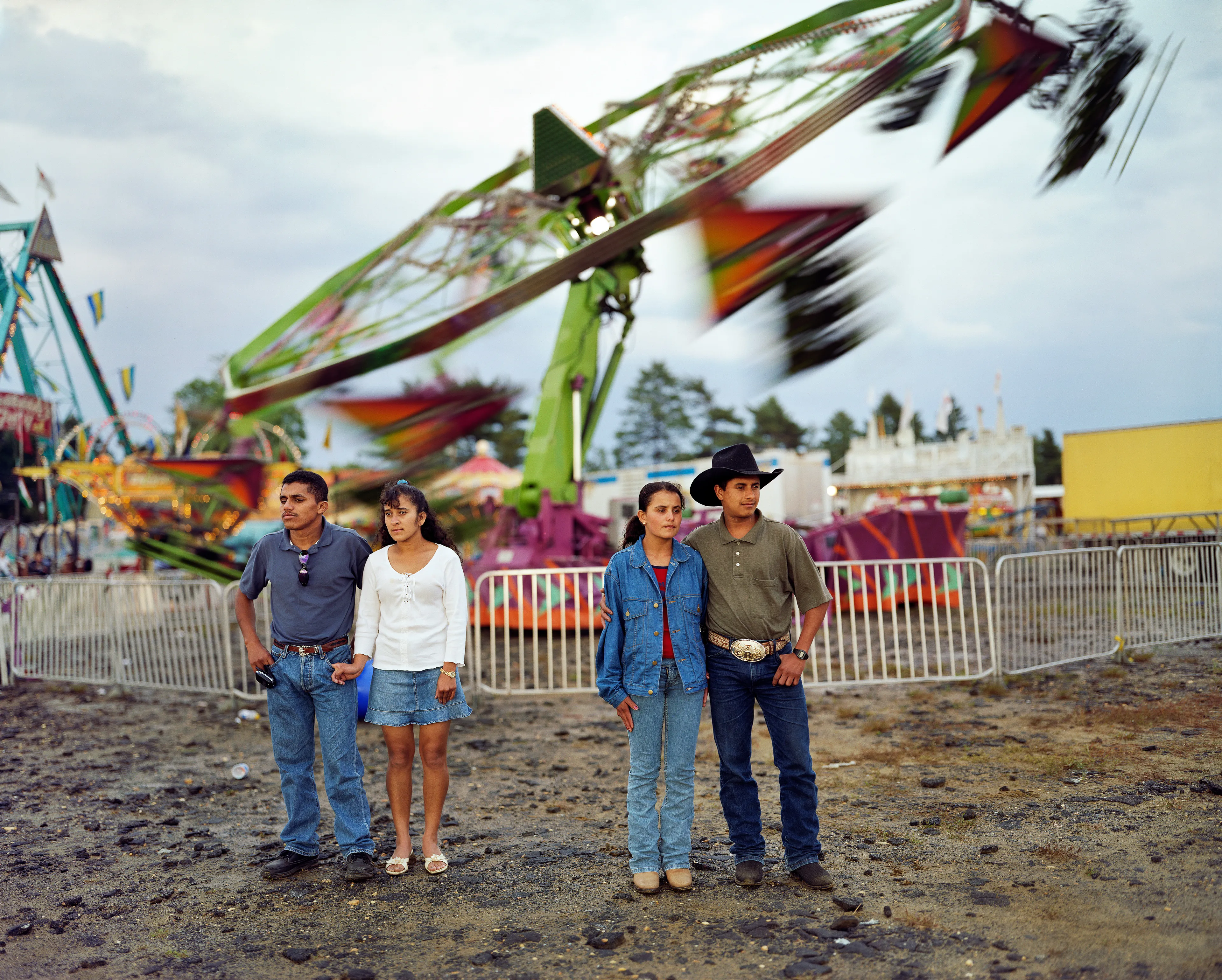 County fairs conjure ideas of tilt-a-whirls, stuffed animals, cotton candy, and blue ribbons. Rooted in local agricultural practices, fairs have been a ubiquitous part of American life for two centuries. In a reassuring way, they seem impervious to economic, technological, or fashion trends. For better or for worse, fairs look the same through the decades.

Though they are places to meet each other, there sure is a lot of loneliness at the fair. The series County Fair captures that duality: an adolescent boy looks up at the woman working the Hot Dog on a Stick stand as if she were a museum diorama; a little red haired girl haltingly befriends a robot; young couples, leaning and draped over each other, hide from the world in plain sight.


In my pictures, the dizzying atmosphere, colorfully decorated to provide amusement and distraction, is imbued with sadness and longing. These feelings, which permeate society, are laid bare at the fair. Sadness and longing circulate, intersect and incubate in the confined space between the ticket booths and the craft barns. People come out to participate and show, to see and be seen. Ultimately, connection remains elusive. 

