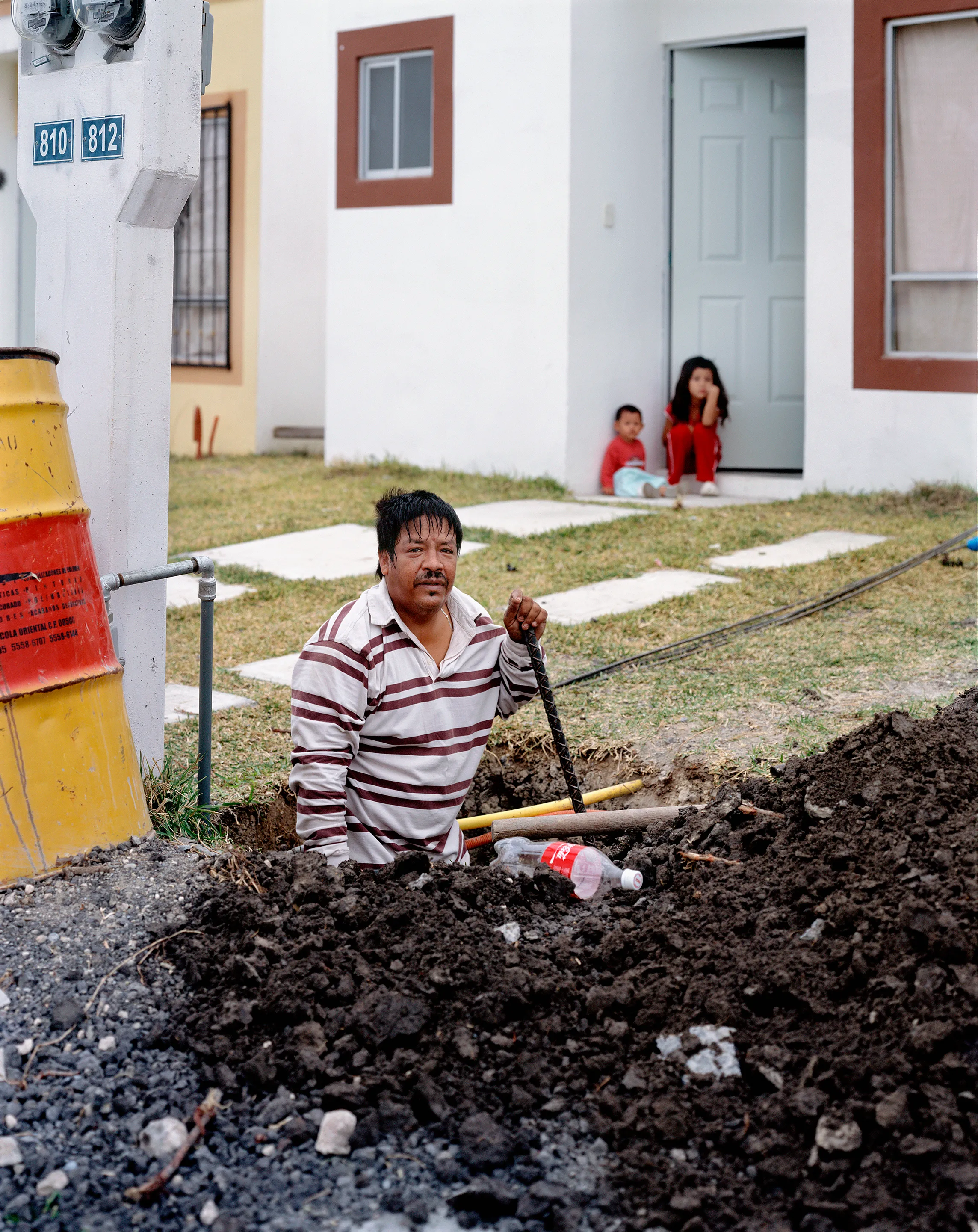 Man digging a whole in front of his house in Juárez, Nuevo León, Mexico, 2005-2010. This image is part of a 5-year project called Suburbia Mexicana. During the first 10 years of the 21st Century, Mexico put forward a housing project that resulted in the construction of hundreds of thousands of homes around my hometown of Monterrey. These are the people who dared to dream to own a new home. I encountered them in their new suburbs and asked them to be part of the representation of a changing landscape we were both living through at that time.  All images were done with a large format 4x5 film camera.