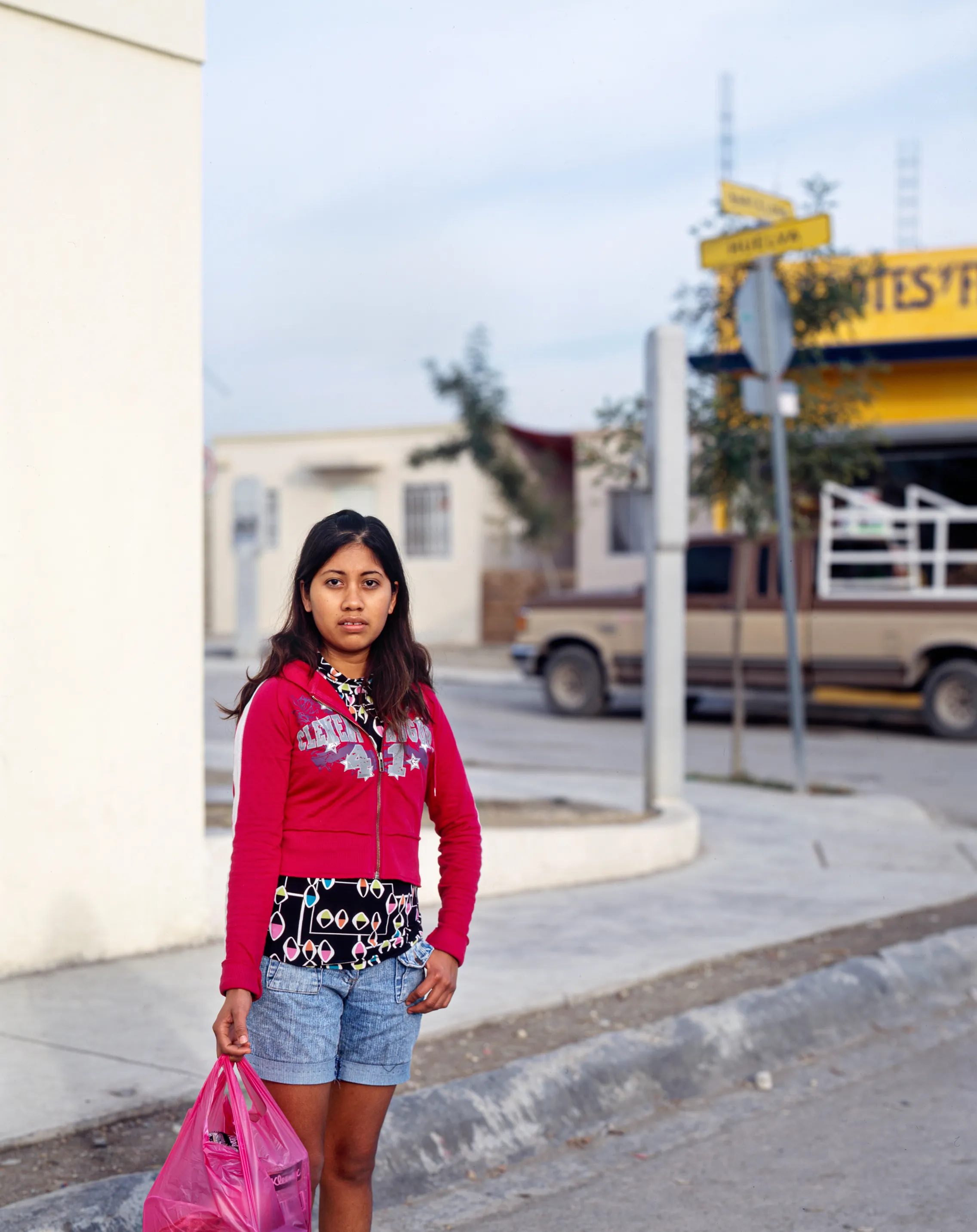 Girl coming home from the store in Juárez, Nuevo León, Mexico, 2005-2010. This image is part of a 5-year project called Suburbia Mexicana. During the first 10 years of the 21st Century, Mexico put forward a housing project that resulted in the construction of hundreds of thousands of homes around my hometown of Monterrey. These are the people who dared to dream to own a new home. I encountered them in their new suburbs and asked them to be part of the representation of a changing landscape we were both living through at that time.  All images were done with a large format 4x5 film camera.