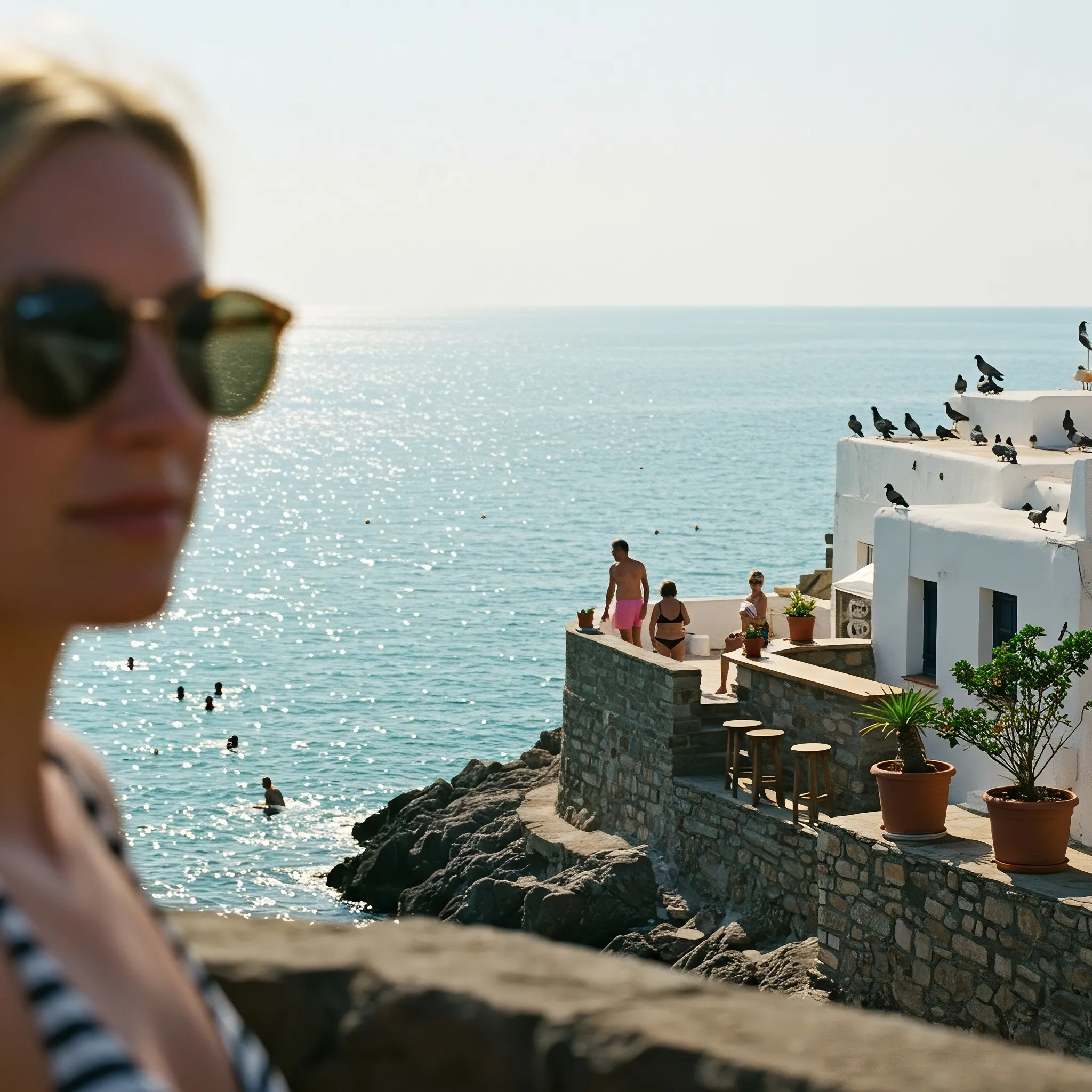 The memory returns not as a whole, but in sun-bleached fragments. There is the rough, warm texture of a rocky ledge beneath my hands, a foreground too close to truly see. My own form is a blur of blonde hair and sunglasses, a ghost overlooking the scene. Beyond me, the world is sharp and alive—a stone terrace where phantom figures in swimwear laugh around a bar, pigeons taking flight from a white-washed roof. The sea holds the most vivid color, a turquoise dream shifting to deep sapphire, and on its glittering surface, tiny swimmers are suspended in a perfect, endless afternoon. I am here, and not here, the silent observer of a day that may have only ever happened in a dream.