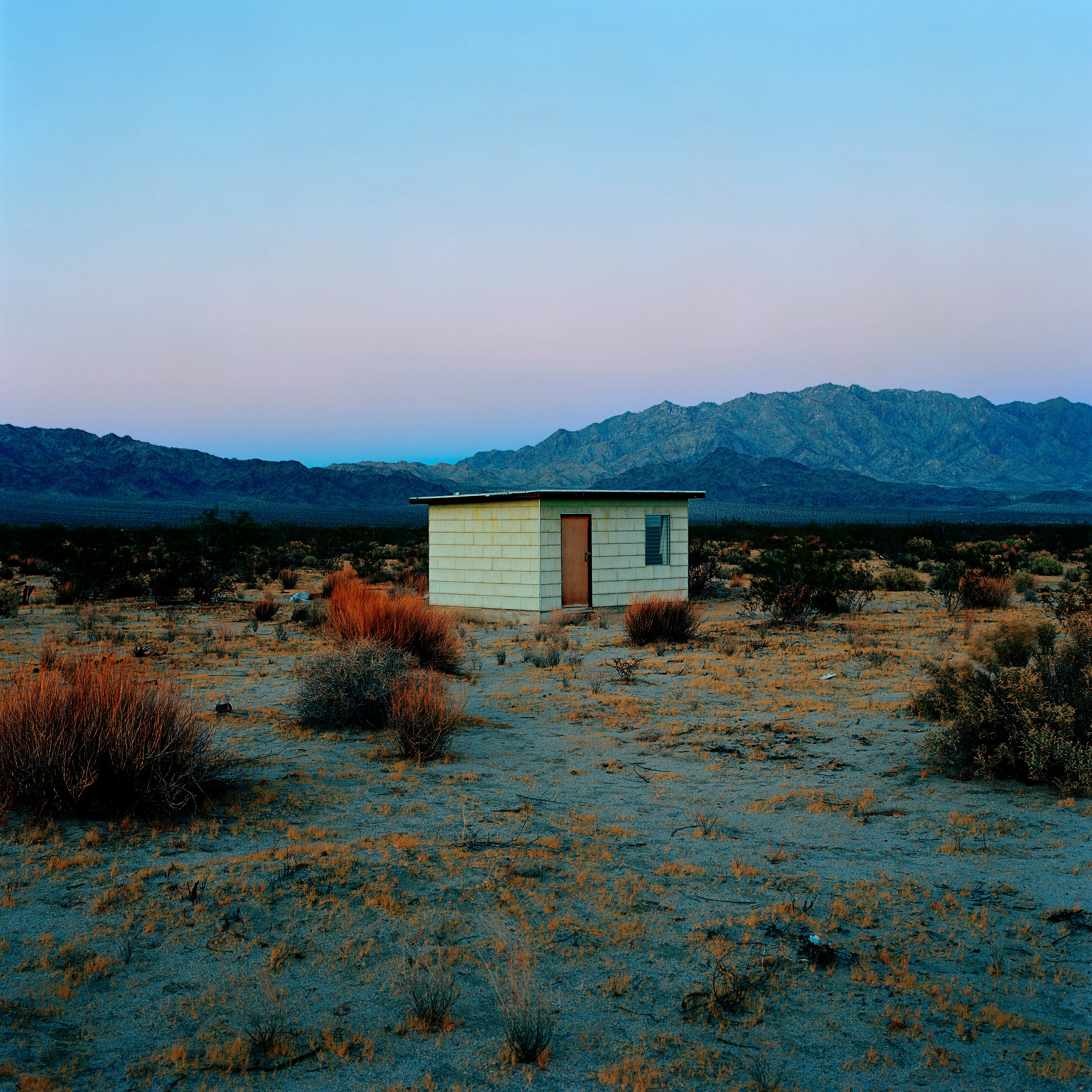 “These are photographs of isolated structures in the high desert of Southern California. All of the images are made in the east end of the Morongo Valley Basin, Wonder Valley, and the area surrounding the town of Twenty-Nine Palms. This is an area approximately one hundred- and fifty-miles due East of Los Angeles. From the oceans edge in L.A., to the area that I am photographing, the landscape is continuously occupied. This area is the final edge of a vast urban expanse. For social, financial, or personal reasons individuals are pushed, or pulled, or simply seek this literal cultural edge. Beyond this point is unoccupied desert.  In the past I have perused projects which dealt with the iconography of transcendence and the sublime. In other projects I have investigated the literal desire to get "outside" of or beyond the cultural (a desire with the ironic consequence of transforming the natural into the very condition one wishes to escape). It is this conceptual trajectory which has led me to this current body of work. This current body of work is an extension of the investigation begun in the "four landscape" portfolio. The structural rigor of that work has been replaced with concerns which are aesthetic and social. On the simplest level I am drawn to the vernacular character of the architecture (painted with a Home Depot palette) as well as the amazing visual character of these structures on this vast desert plain lit by an extraordinary light. However, at base, my primary interest is to create images which are iconographic of a desire. A desire to be "beyond," a desire to be alone, a sign of man on the landscape”. - John Divola.

Edition: 1 of 1