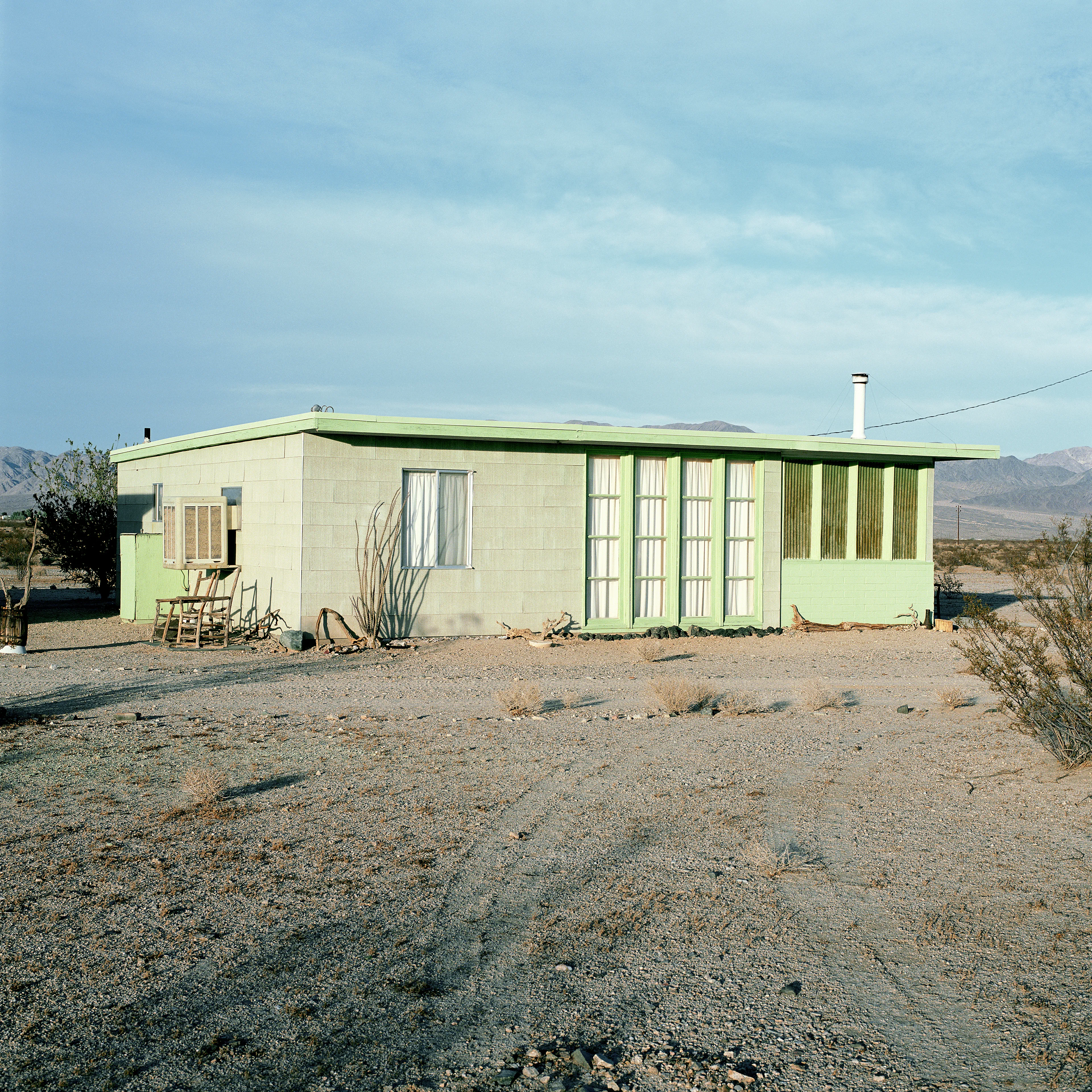 “These are photographs of isolated structures in the high desert of Southern California. All of the images are made in the east end of the Morongo Valley Basin, Wonder Valley, and the area surrounding the town of Twenty-Nine Palms. This is an area approximately one hundred- and fifty-miles due East of Los Angeles. From the oceans edge in L.A., to the area that I am photographing, the landscape is continuously occupied. This area is the final edge of a vast urban expanse. For social, financial, or personal reasons individuals are pushed, or pulled, or simply seek this literal cultural edge. Beyond this point is unoccupied desert.  In the past I have perused projects which dealt with the iconography of transcendence and the sublime. In other projects I have investigated the literal desire to get "outside" of or beyond the cultural (a desire with the ironic consequence of transforming the natural into the very condition one wishes to escape). It is this conceptual trajectory which has led me to this current body of work. This current body of work is an extension of the investigation begun in the "four landscape" portfolio. The structural rigor of that work has been replaced with concerns which are aesthetic and social. On the simplest level I am drawn to the vernacular character of the architecture (painted with a Home Depot palette) as well as the amazing visual character of these structures on this vast desert plain lit by an extraordinary light. However, at base, my primary interest is to create images which are iconographic of a desire. A desire to be "beyond", a desire to be alone, a sign of man on the landscape”. - John Divola.

Edition: 1 of 1