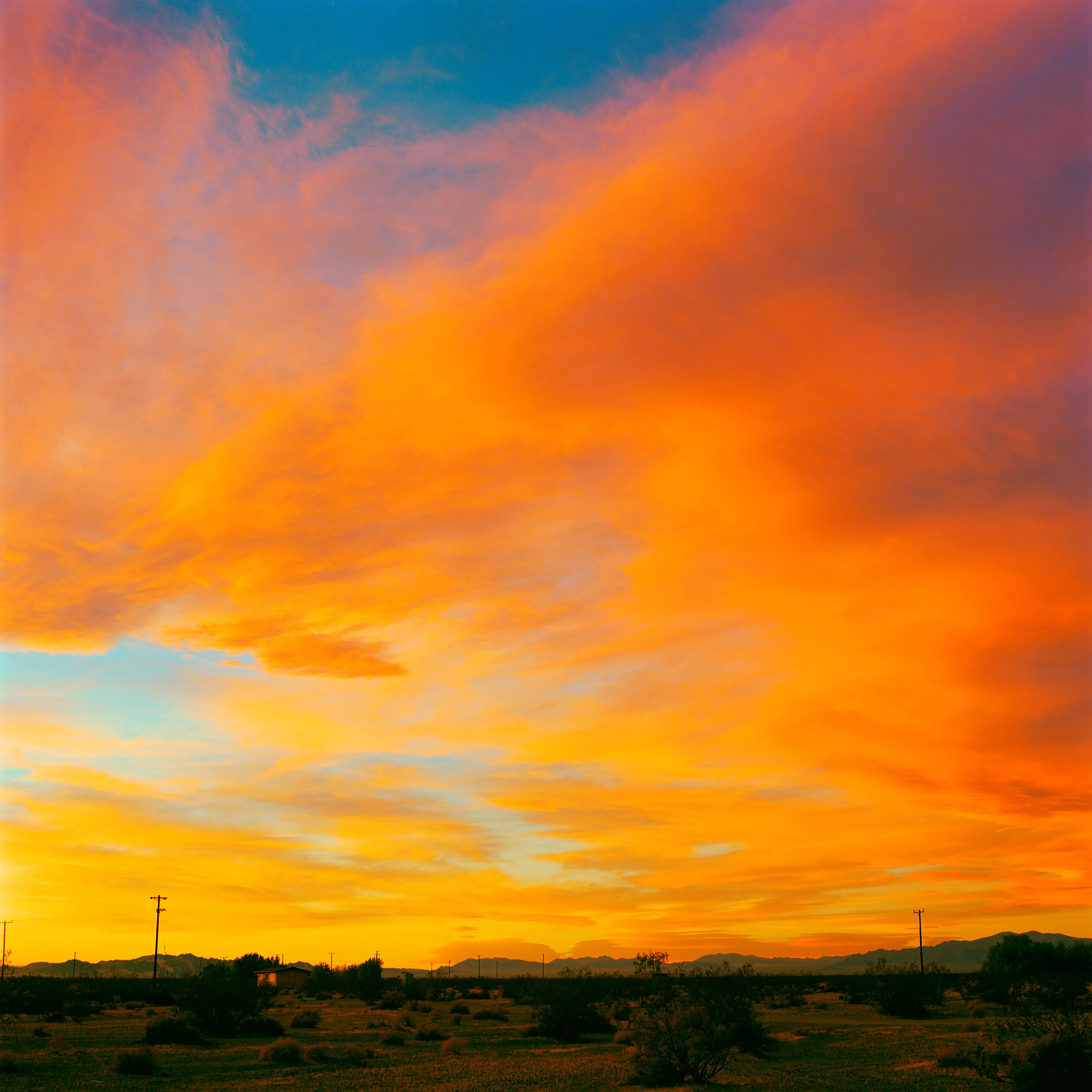 “These are photographs of isolated structures in the high desert of Southern California. All of the images are made in the east end of the Morongo Valley Basin, Wonder Valley, and the area surrounding the town of Twenty-Nine Palms. This is an area approximately one hundred- and fifty-miles due East of Los Angeles. From the oceans edge in L.A., to the area that I am photographing, the landscape is continuously occupied. This area is the final edge of a vast urban expanse. For social, financial, or personal reasons individuals are pushed, or pulled, or simply seek this literal cultural edge. Beyond this point is unoccupied desert.  In the past I have perused projects which dealt with the iconography of transcendence and the sublime. In other projects I have investigated the literal desire to get "outside" of or beyond the cultural (a desire with the ironic consequence of transforming the natural into the very condition one wishes to escape). It is this conceptual trajectory which has led me to this current body of work. This current body of work is an extension of the investigation begun in the "four landscape" portfolio. The structural rigor of that work has been replaced with concerns which are aesthetic and social. On the simplest level I am drawn to the vernacular character of the architecture (painted with a Home Depot palette) as well as the amazing visual character of these structures on this vast desert plain lit by an extraordinary light. However, at base, my primary interest is to create images which are iconographic of a desire. A desire to be "beyond," a desire to be alone, a sign of man on the landscape”. - John Divola.

Edition: 1 of 1