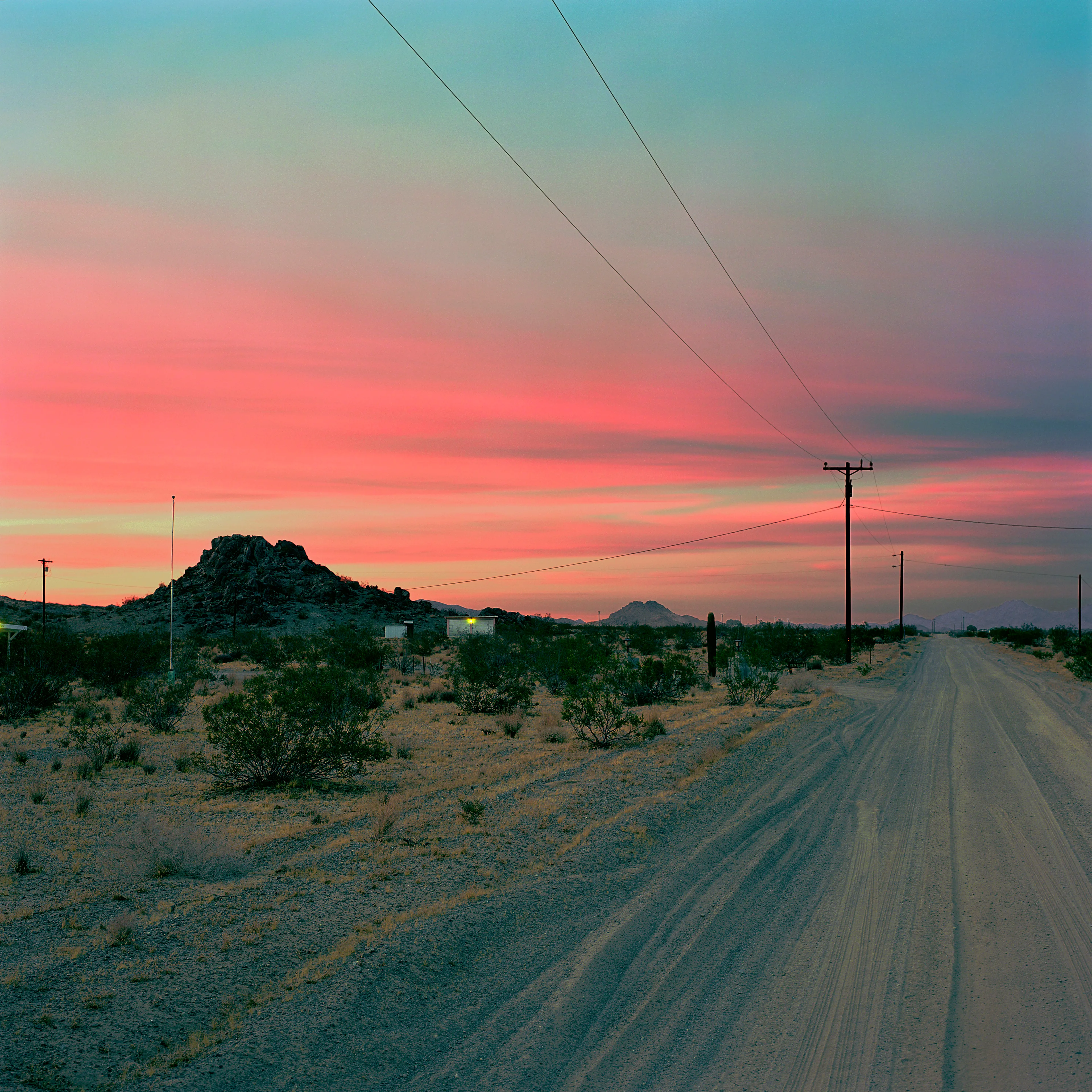 “These are photographs of isolated structures in the high desert of Southern California. All of the images are made in the east end of the Morongo Valley Basin, Wonder Valley, and the area surrounding the town of Twenty-Nine Palms. This is an area approximately one hundred- and fifty-miles due East of Los Angeles. From the oceans edge in L.A., to the area that I am photographing, the landscape is continuously occupied. This area is the final edge of a vast urban expanse. For social, financial, or personal reasons individuals are pushed, or pulled, or simply seek this literal cultural edge. Beyond this point is unoccupied desert.  In the past I have perused projects which dealt with the iconography of transcendence and the sublime. In other projects I have investigated the literal desire to get "outside" of or beyond the cultural (a desire with the ironic consequence of transforming the natural into the very condition one wishes to escape). It is this conceptual trajectory which has led me to this current body of work. This current body of work is an extension of the investigation begun in the "four landscape" portfolio. The structural rigor of that work has been replaced with concerns which are aesthetic and social. On the simplest level I am drawn to the vernacular character of the architecture (painted with a Home Depot palette) as well as the amazing visual character of these structures on this vast desert plain lit by an extraordinary light. However, at base, my primary interest is to create images which are iconographic of a desire. A desire to be "beyond," a desire to be alone, a sign of man on the landscape”. - John Divola.

Edition: 1 of 1