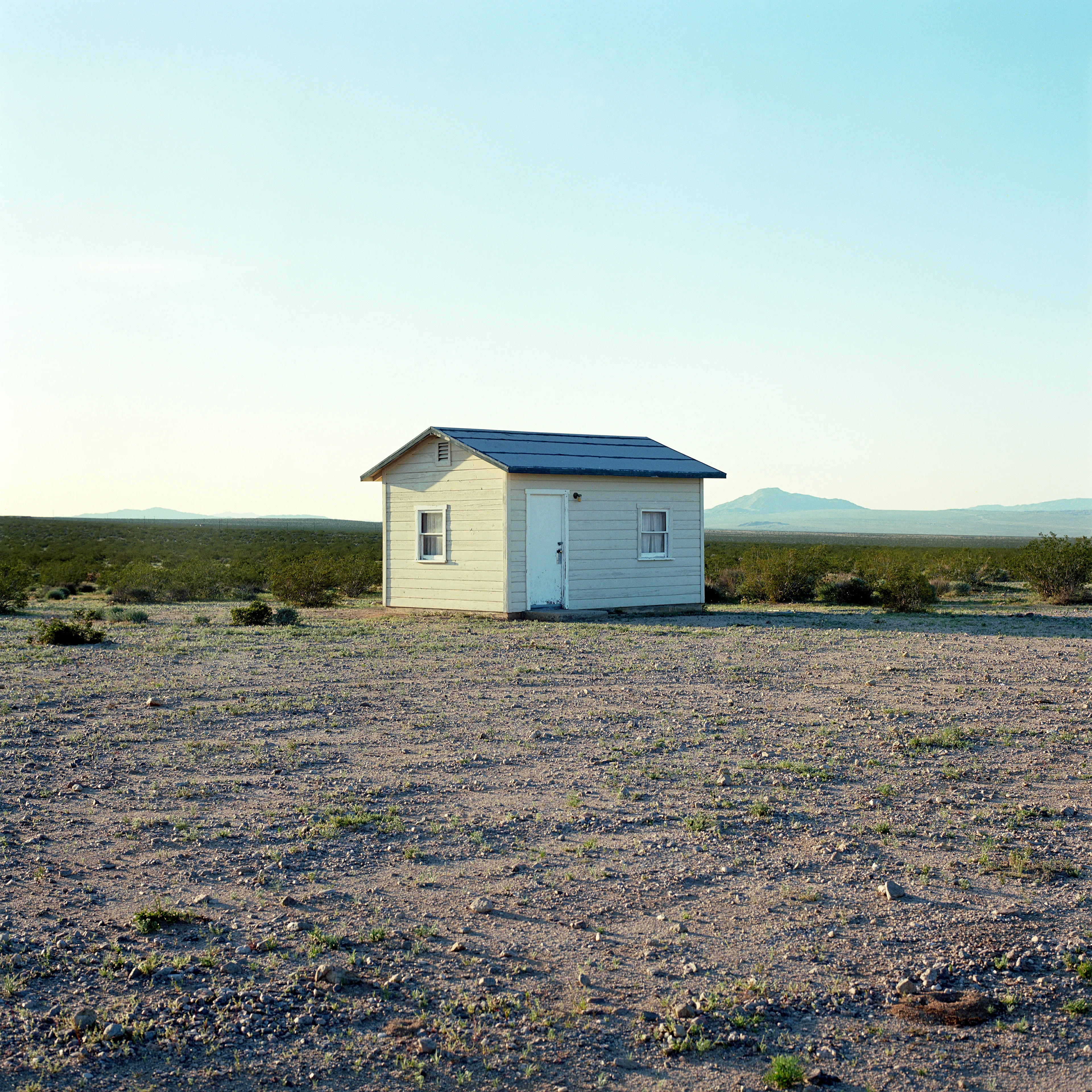 “These are photographs of isolated structures in the high desert of Southern California. All of the images are made in the east end of the Morongo Valley Basin, Wonder Valley, and the area surrounding the town of Twenty-Nine Palms. This is an area approximately one hundred- and fifty-miles due East of Los Angeles. From the oceans edge in L.A., to the area that I am photographing, the landscape is continuously occupied. This area is the final edge of a vast urban expanse. For social, financial, or personal reasons individuals are pushed, or pulled, or simply seek this literal cultural edge. Beyond this point is unoccupied desert.  In the past I have perused projects which dealt with the iconography of transcendence and the sublime. In other projects I have investigated the literal desire to get "outside" of or beyond the cultural (a desire with the ironic consequence of transforming the natural into the very condition one wishes to escape). It is this conceptual trajectory which has led me to this current body of work. This current body of work is an extension of the investigation begun in the "four landscape" portfolio. The structural rigor of that work has been replaced with concerns which are aesthetic and social. On the simplest level I am drawn to the vernacular character of the architecture (painted with a Home Depot palette) as well as the amazing visual character of these structures on this vast desert plain lit by an extraordinary light. However, at base, my primary interest is to create images which are iconographic of a desire. A desire to be "beyond", a desire to be alone, a sign of man on the landscape”. - John Divola.

Edition: 1 of 1