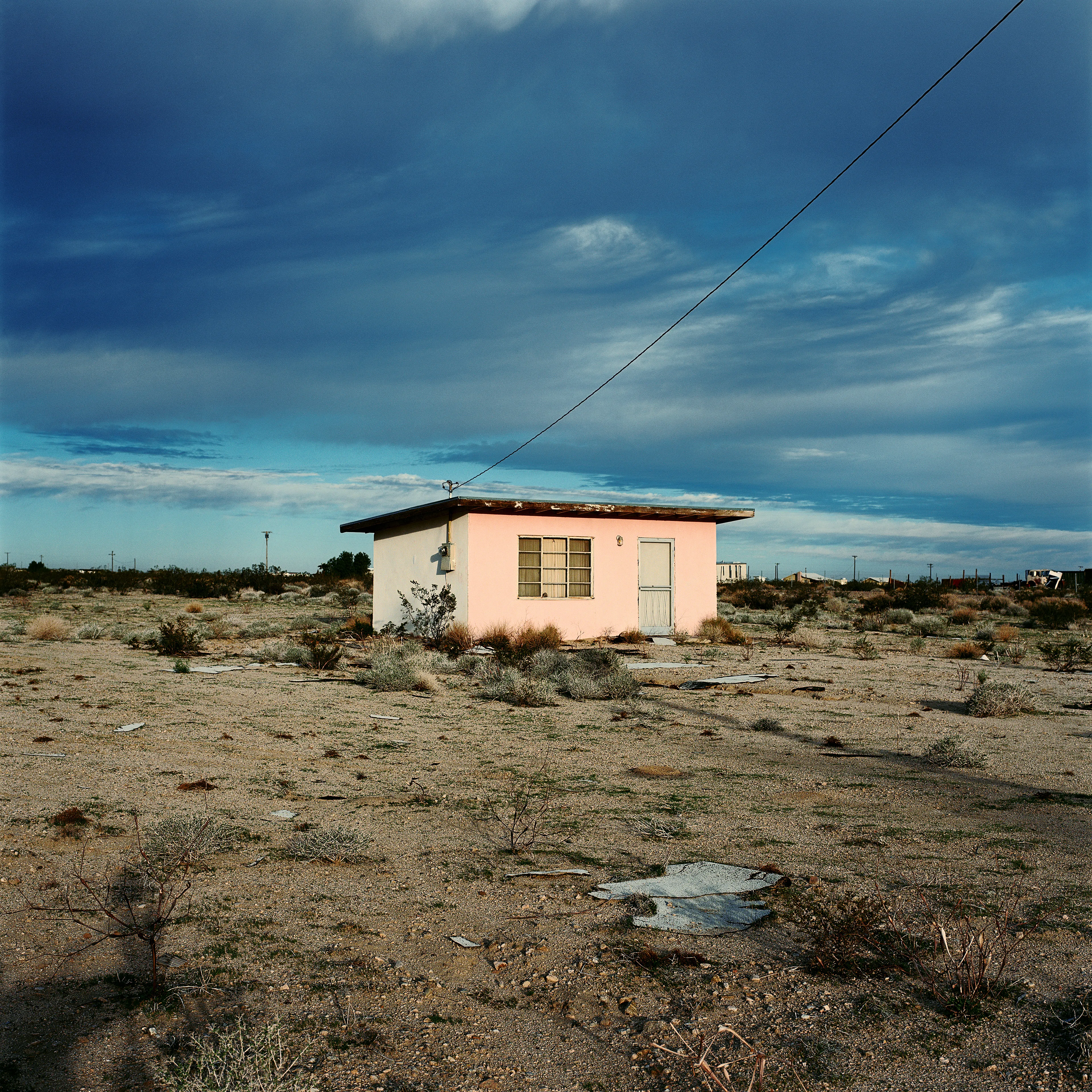 “These are photographs of isolated structures in the high desert of Southern California. All of the images are made in the east end of the Morongo Valley Basin, Wonder Valley, and the area surrounding the town of Twenty-Nine Palms. This is an area approximately one hundred- and fifty-miles due East of Los Angeles. From the oceans edge in L.A., to the area that I am photographing, the landscape is continuously occupied. This area is the final edge of a vast urban expanse. For social, financial, or personal reasons individuals are pushed, or pulled, or simply seek this literal cultural edge. Beyond this point is unoccupied desert.  In the past I have perused projects which dealt with the iconography of transcendence and the sublime. In other projects I have investigated the literal desire to get "outside" of or beyond the cultural (a desire with the ironic consequence of transforming the natural into the very condition one wishes to escape). It is this conceptual trajectory which has led me to this current body of work. This current body of work is an extension of the investigation begun in the "four landscape" portfolio. The structural rigor of that work has been replaced with concerns which are aesthetic and social. On the simplest level I am drawn to the vernacular character of the architecture (painted with a Home Depot palette) as well as the amazing visual character of these structures on this vast desert plain lit by an extraordinary light. However, at base, my primary interest is to create images which are iconographic of a desire. A desire to be "beyond," a desire to be alone, a sign of man on the landscape”. - John Divola.

Edition: 1 of 1