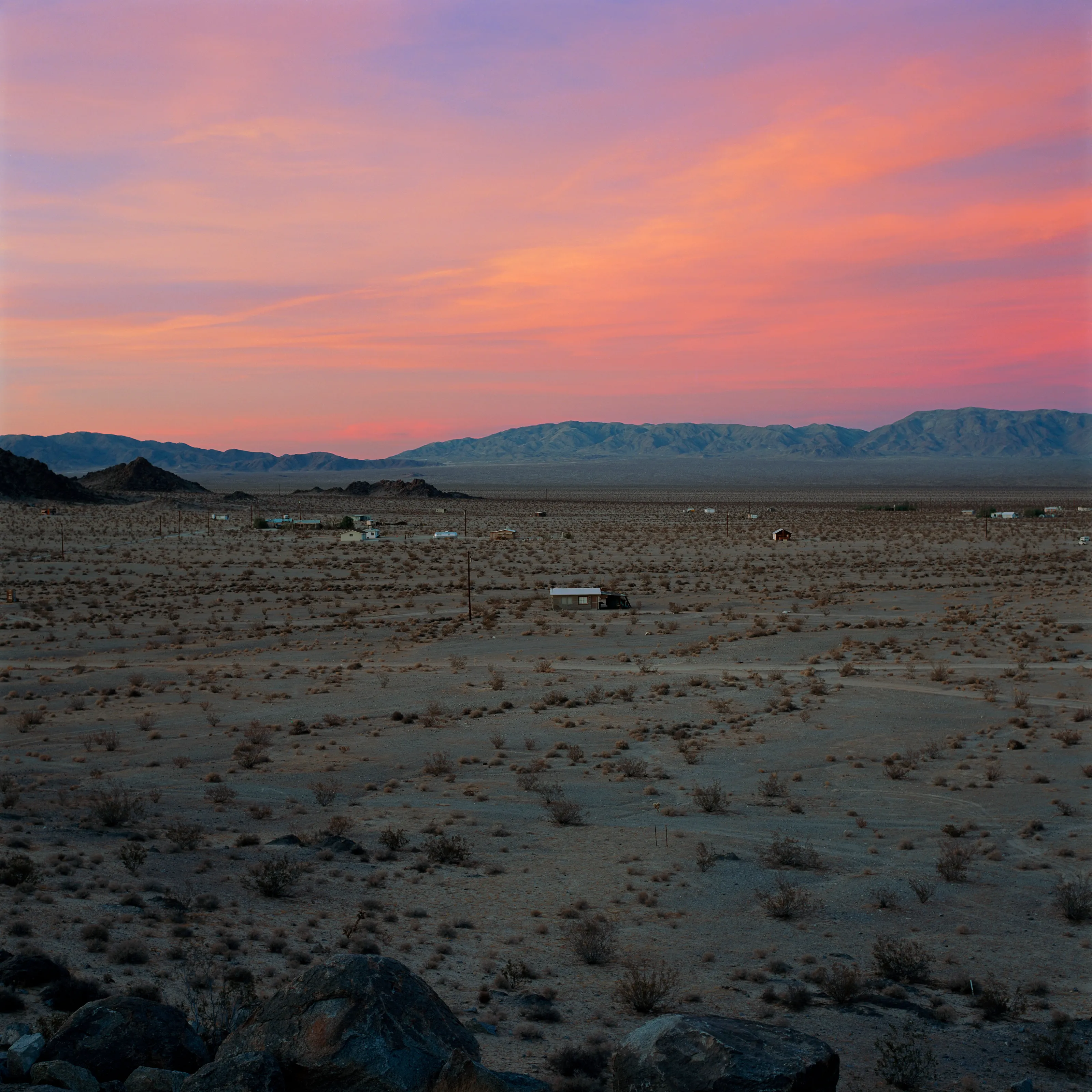 “These are photographs of isolated structures in the high desert of Southern California. All of the images are made in the east end of the Morongo Valley Basin, Wonder Valley, and the area surrounding the town of Twenty-Nine Palms. This is an area approximately one hundred- and fifty-miles due East of Los Angeles. From the oceans edge in L.A., to the area that I am photographing, the landscape is continuously occupied. This area is the final edge of a vast urban expanse. For social, financial, or personal reasons individuals are pushed, or pulled, or simply seek this literal cultural edge. Beyond this point is unoccupied desert.  In the past I have perused projects which dealt with the iconography of transcendence and the sublime. In other projects I have investigated the literal desire to get "outside" of or beyond the cultural (a desire with the ironic consequence of transforming the natural into the very condition one wishes to escape). It is this conceptual trajectory which has led me to this current body of work. This current body of work is an extension of the investigation begun in the "four landscape" portfolio. The structural rigor of that work has been replaced with concerns which are aesthetic and social. On the simplest level I am drawn to the vernacular character of the architecture (painted with a Home Depot palette) as well as the amazing visual character of these structures on this vast desert plain lit by an extraordinary light. However, at base, my primary interest is to create images which are iconographic of a desire. A desire to be "beyond," a desire to be alone, a sign of man on the landscape”. - John Divola.

Edition: 1 of 1