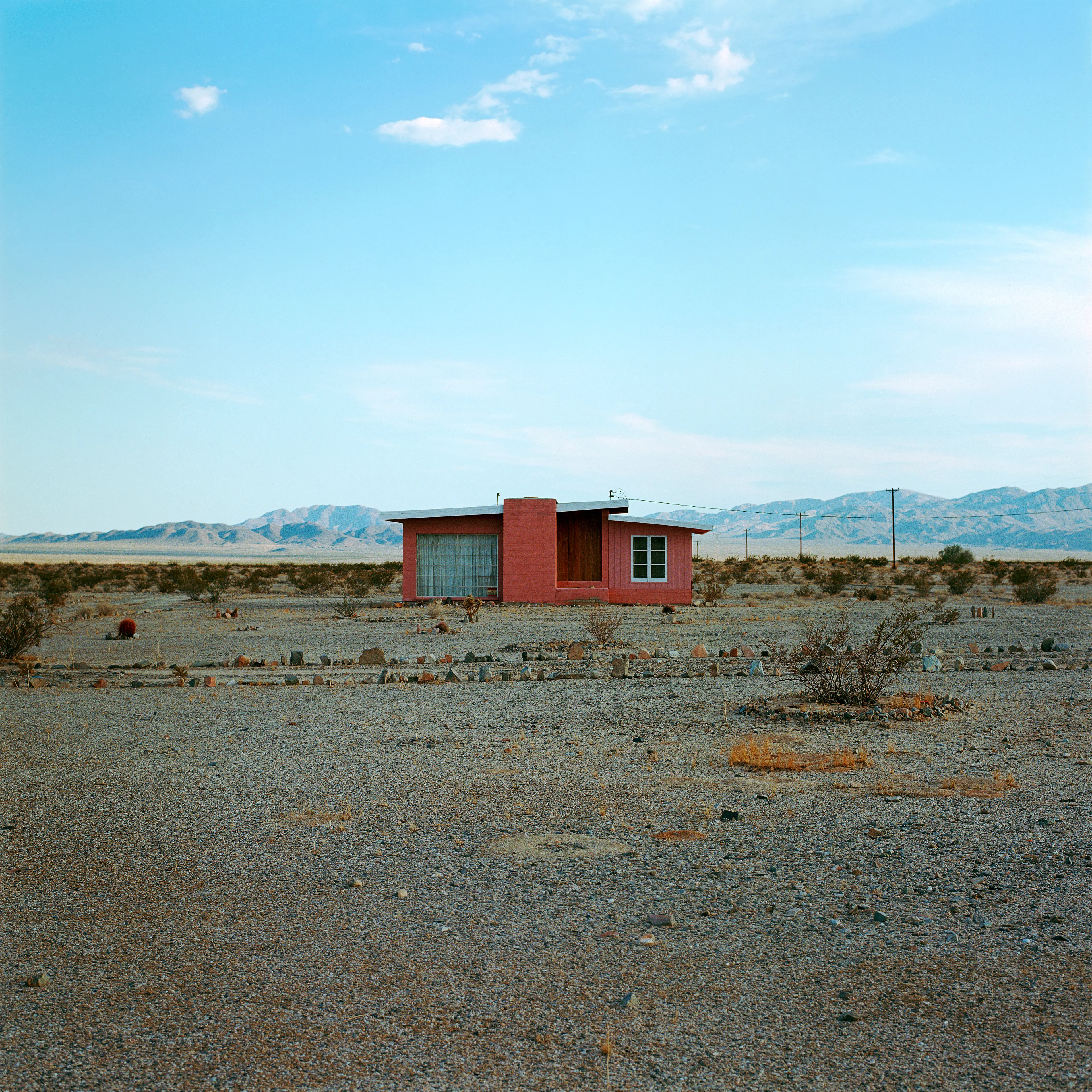 “These are photographs of isolated structures in the high desert of Southern California. All of the images are made in the east end of the Morongo Valley Basin, Wonder Valley, and the area surrounding the town of Twenty-Nine Palms. This is an area approximately one hundred- and fifty-miles due East of Los Angeles. From the oceans edge in L.A., to the area that I am photographing, the landscape is continuously occupied. This area is the final edge of a vast urban expanse. For social, financial, or personal reasons individuals are pushed, or pulled, or simply seek this literal cultural edge. Beyond this point is unoccupied desert.  In the past I have perused projects which dealt with the iconography of transcendence and the sublime. In other projects I have investigated the literal desire to get "outside" of or beyond the cultural (a desire with the ironic consequence of transforming the natural into the very condition one wishes to escape). It is this conceptual trajectory which has led me to this current body of work. This current body of work is an extension of the investigation begun in the "four landscape" portfolio. The structural rigor of that work has been replaced with concerns which are aesthetic and social. On the simplest level I am drawn to the vernacular character of the architecture (painted with a Home Depot palette) as well as the amazing visual character of these structures on this vast desert plain lit by an extraordinary light. However, at base, my primary interest is to create images which are iconographic of a desire. A desire to be "beyond", a desire to be alone, a sign of man on the landscape”. - John Divola.

Edition: 1 of 1