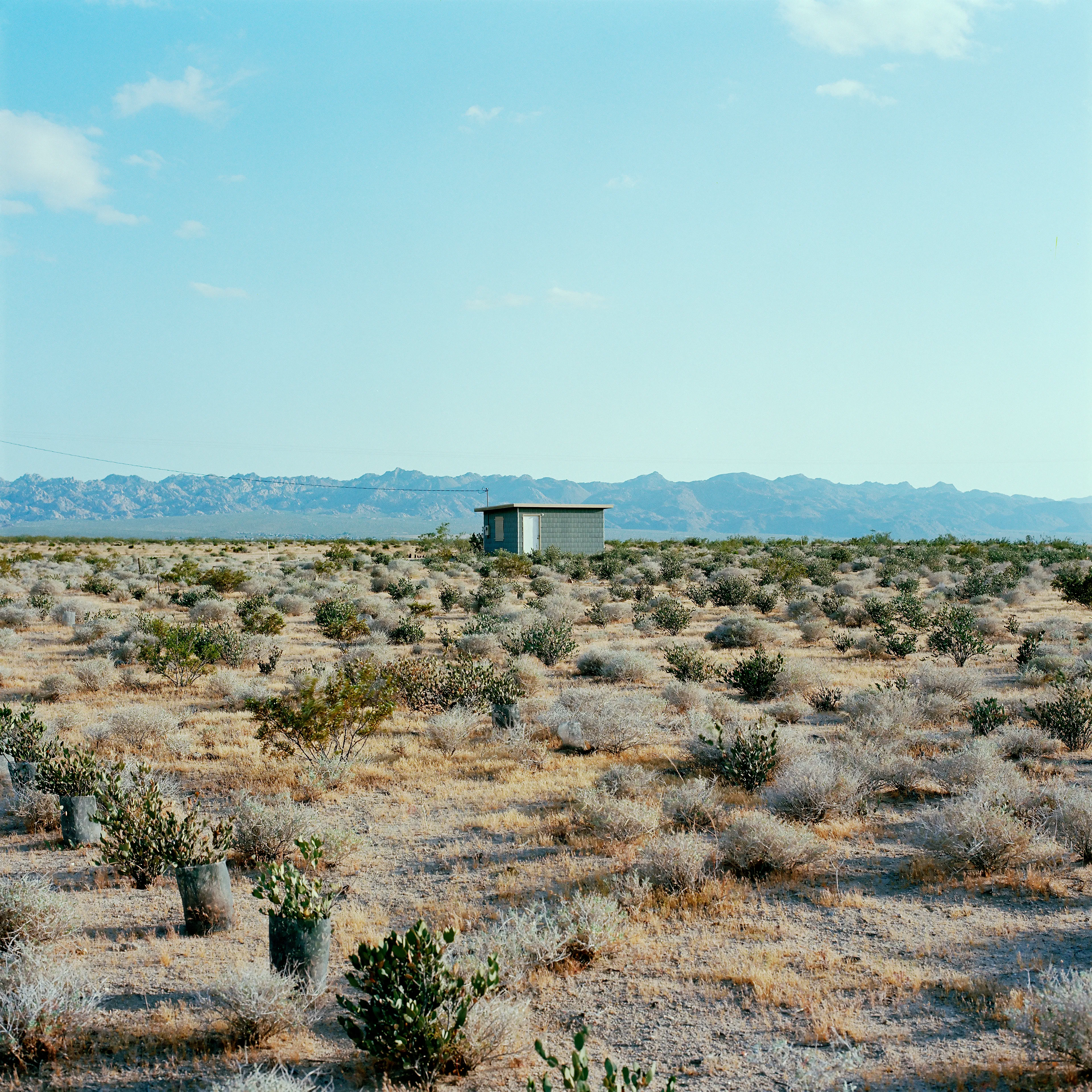 “These are photographs of isolated structures in the high desert of Southern California. All of the images are made in the east end of the Morongo Valley Basin, Wonder Valley, and the area surrounding the town of Twenty-Nine Palms. This is an area approximately one hundred- and fifty-miles due East of Los Angeles. From the oceans edge in L.A., to the area that I am photographing, the landscape is continuously occupied. This area is the final edge of a vast urban expanse. For social, financial, or personal reasons individuals are pushed, or pulled, or simply seek this literal cultural edge. Beyond this point is unoccupied desert.  In the past I have perused projects which dealt with the iconography of transcendence and the sublime. In other projects I have investigated the literal desire to get "outside" of or beyond the cultural (a desire with the ironic consequence of transforming the natural into the very condition one wishes to escape). It is this conceptual trajectory which has led me to this current body of work. This current body of work is an extension of the investigation begun in the "four landscape" portfolio. The structural rigor of that work has been replaced with concerns which are aesthetic and social. On the simplest level I am drawn to the vernacular character of the architecture (painted with a Home Depot palette) as well as the amazing visual character of these structures on this vast desert plain lit by an extraordinary light. However, at base, my primary interest is to create images which are iconographic of a desire. A desire to be "beyond", a desire to be alone, a sign of man on the landscape”. - John Divola.

Edition: 1 of 1