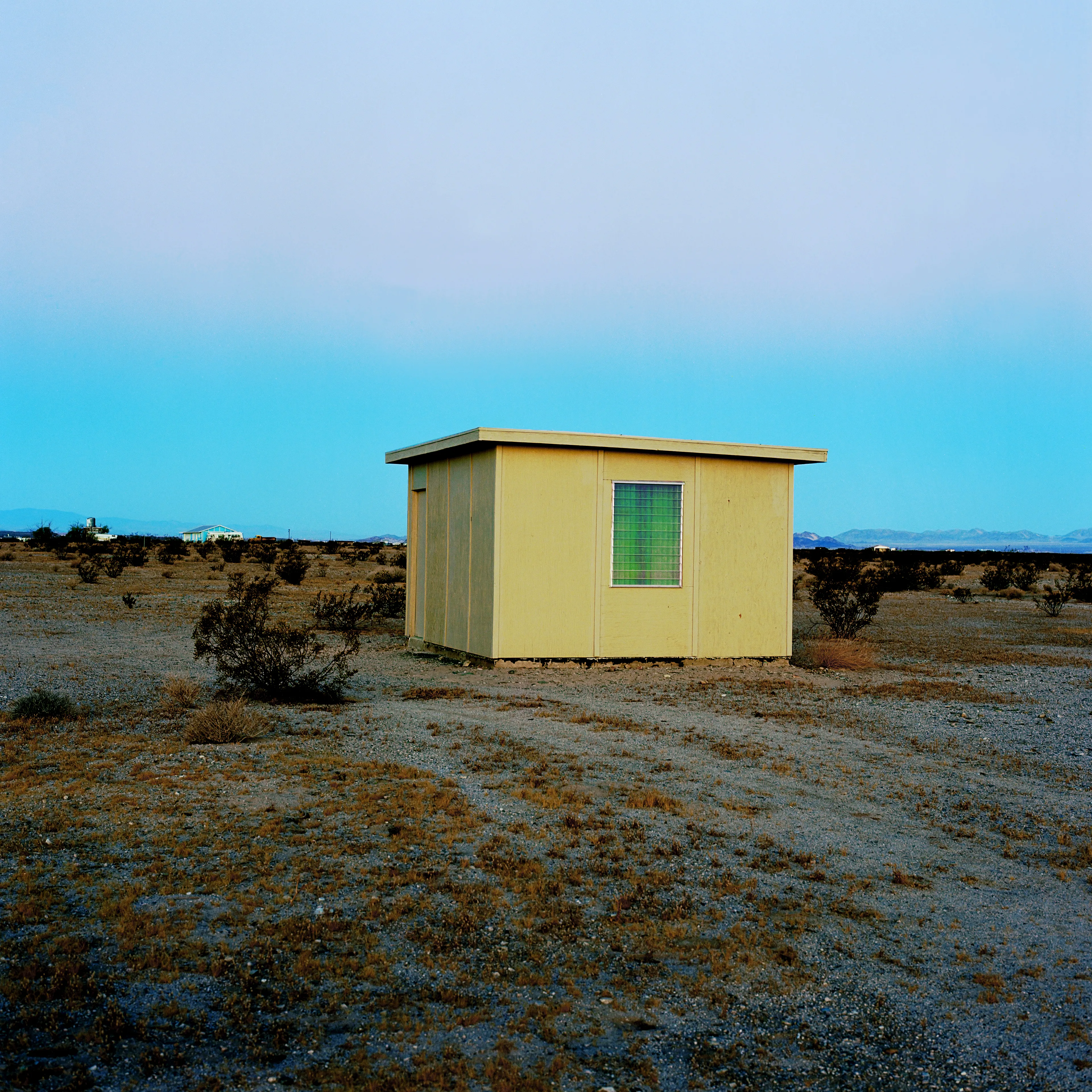 “These are photographs of isolated structures in the high desert of Southern California. All of the images are made in the east end of the Morongo Valley Basin, Wonder Valley, and the area surrounding the town of Twenty-Nine Palms. This is an area approximately one hundred- and fifty-miles due East of Los Angeles. From the oceans edge in L.A., to the area that I am photographing, the landscape is continuously occupied. This area is the final edge of a vast urban expanse. For social, financial, or personal reasons individuals are pushed, or pulled, or simply seek this literal cultural edge. Beyond this point is unoccupied desert.  In the past I have perused projects which dealt with the iconography of transcendence and the sublime. In other projects I have investigated the literal desire to get "outside" of or beyond the cultural (a desire with the ironic consequence of transforming the natural into the very condition one wishes to escape). It is this conceptual trajectory which has led me to this current body of work. This current body of work is an extension of the investigation begun in the "four landscape" portfolio. The structural rigor of that work has been replaced with concerns which are aesthetic and social. On the simplest level I am drawn to the vernacular character of the architecture (painted with a Home Depot palette) as well as the amazing visual character of these structures on this vast desert plain lit by an extraordinary light. However, at base, my primary interest is to create images which are iconographic of a desire. A desire to be "beyond", a desire to be alone, a sign of man on the landscape”. - John Divola.

Edition: 1 of 1