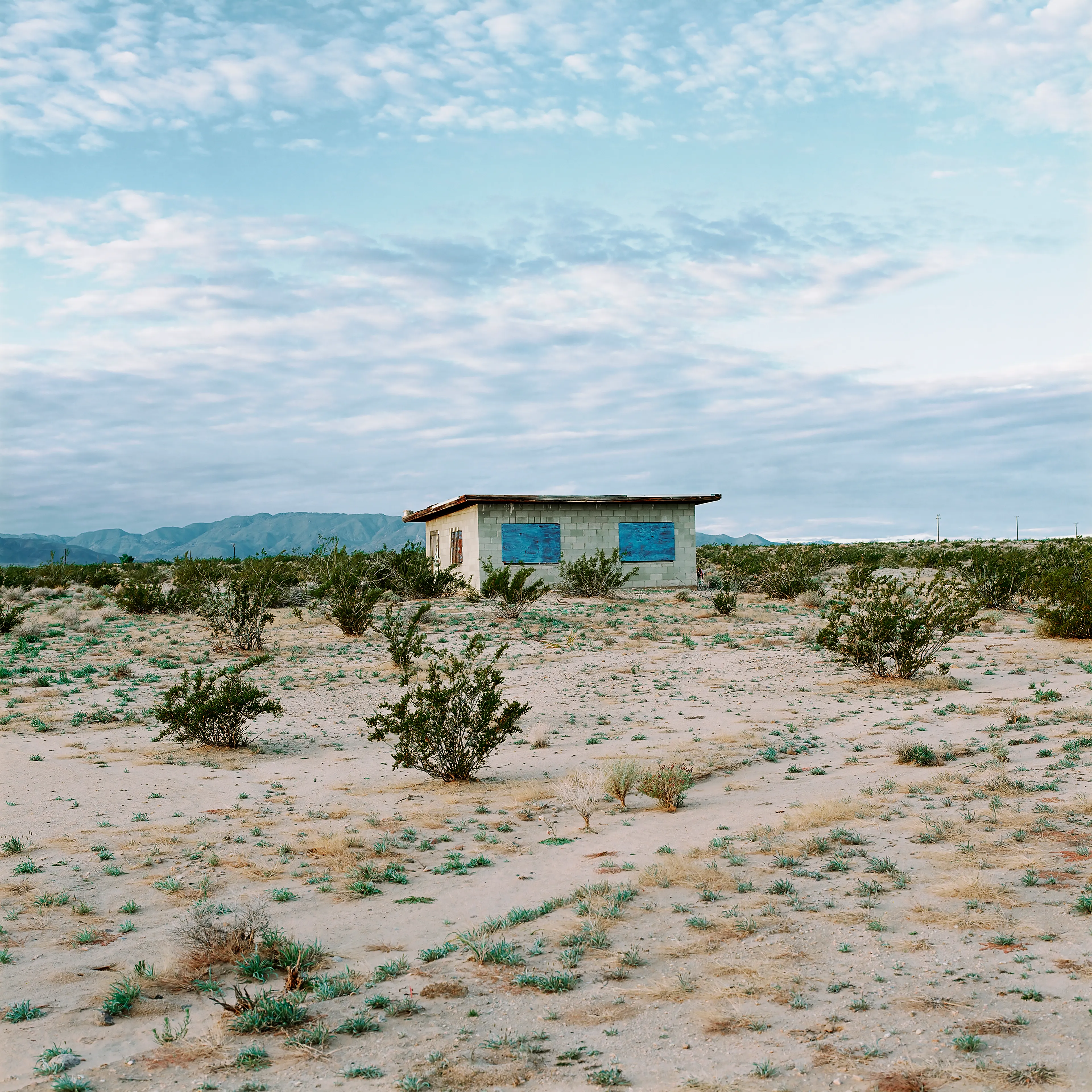 “These are photographs of isolated structures in the high desert of Southern California. All of the images are made in the east end of the Morongo Valley Basin, Wonder Valley, and the area surrounding the town of Twenty-Nine Palms. This is an area approximately one hundred- and fifty-miles due East of Los Angeles. From the oceans edge in L.A., to the area that I am photographing, the landscape is continuously occupied. This area is the final edge of a vast urban expanse. For social, financial, or personal reasons individuals are pushed, or pulled, or simply seek this literal cultural edge. Beyond this point is unoccupied desert.  In the past I have perused projects which dealt with the iconography of transcendence and the sublime. In other projects I have investigated the literal desire to get "outside" of or beyond the cultural (a desire with the ironic consequence of transforming the natural into the very condition one wishes to escape). It is this conceptual trajectory which has led me to this current body of work. This current body of work is an extension of the investigation begun in the "four landscape" portfolio. The structural rigor of that work has been replaced with concerns which are aesthetic and social. On the simplest level I am drawn to the vernacular character of the architecture (painted with a Home Depot palette) as well as the amazing visual character of these structures on this vast desert plain lit by an extraordinary light. However, at base, my primary interest is to create images which are iconographic of a desire. A desire to be "beyond", a desire to be alone, a sign of man on the landscape”. - John Divola.

Edition: 1 of 1