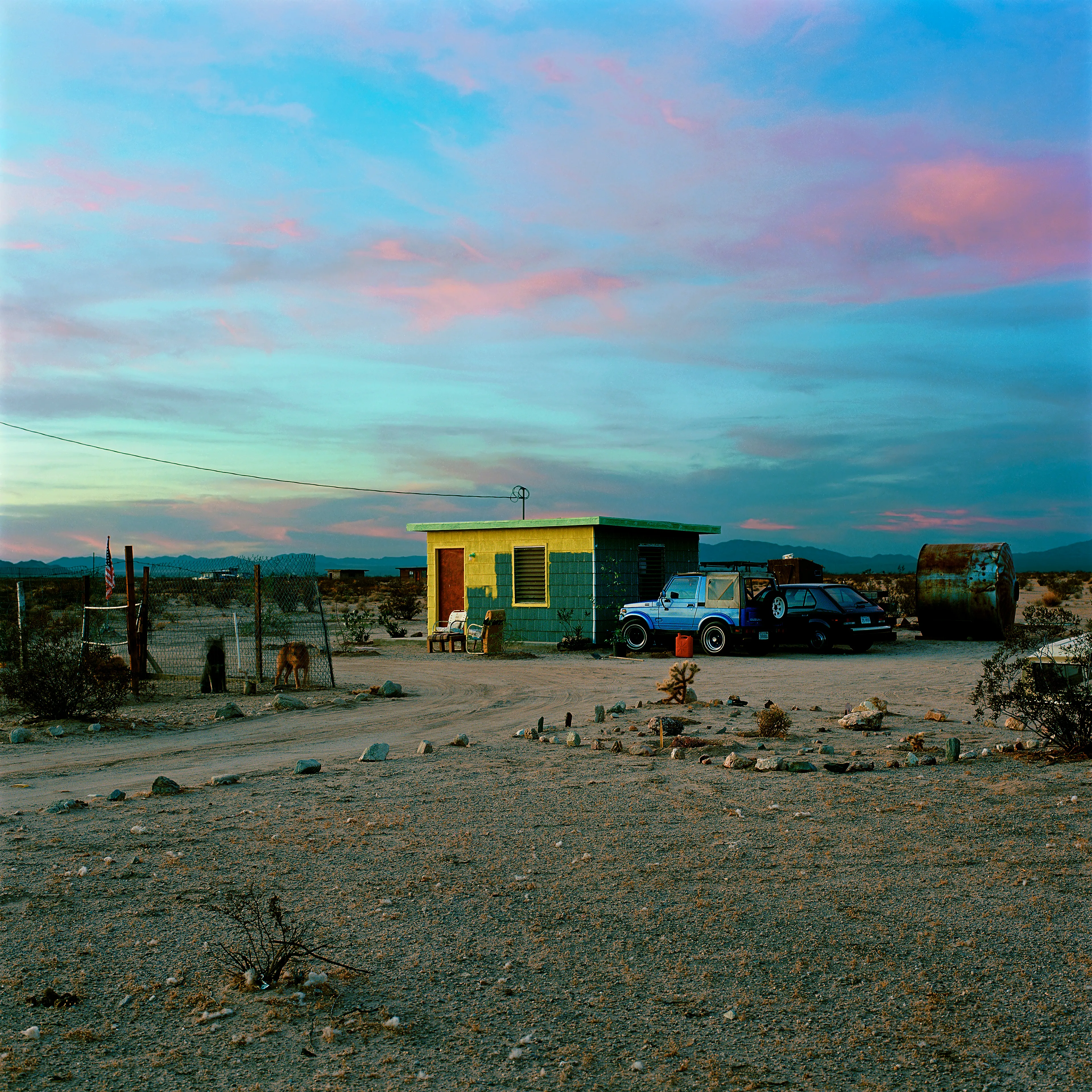 “These are photographs of isolated structures in the high desert of Southern California. All of the images are made in the east end of the Morongo Valley Basin, Wonder Valley, and the area surrounding the town of Twenty-Nine Palms. This is an area approximately one hundred- and fifty-miles due East of Los Angeles. From the oceans edge in L.A., to the area that I am photographing, the landscape is continuously occupied. This area is the final edge of a vast urban expanse. For social, financial, or personal reasons individuals are pushed, or pulled, or simply seek this literal cultural edge. Beyond this point is unoccupied desert.  In the past I have perused projects which dealt with the iconography of transcendence and the sublime. In other projects I have investigated the literal desire to get "outside" of or beyond the cultural (a desire with the ironic consequence of transforming the natural into the very condition one wishes to escape). It is this conceptual trajectory which has led me to this current body of work. This current body of work is an extension of the investigation begun in the "four landscape" portfolio. The structural rigor of that work has been replaced with concerns which are aesthetic and social. On the simplest level I am drawn to the vernacular character of the architecture (painted with a Home Depot palette) as well as the amazing visual character of these structures on this vast desert plain lit by an extraordinary light. However, at base, my primary interest is to create images which are iconographic of a desire. A desire to be "beyond", a desire to be alone, a sign of man on the landscape”. - John Divola.

Edition: 1 of 1