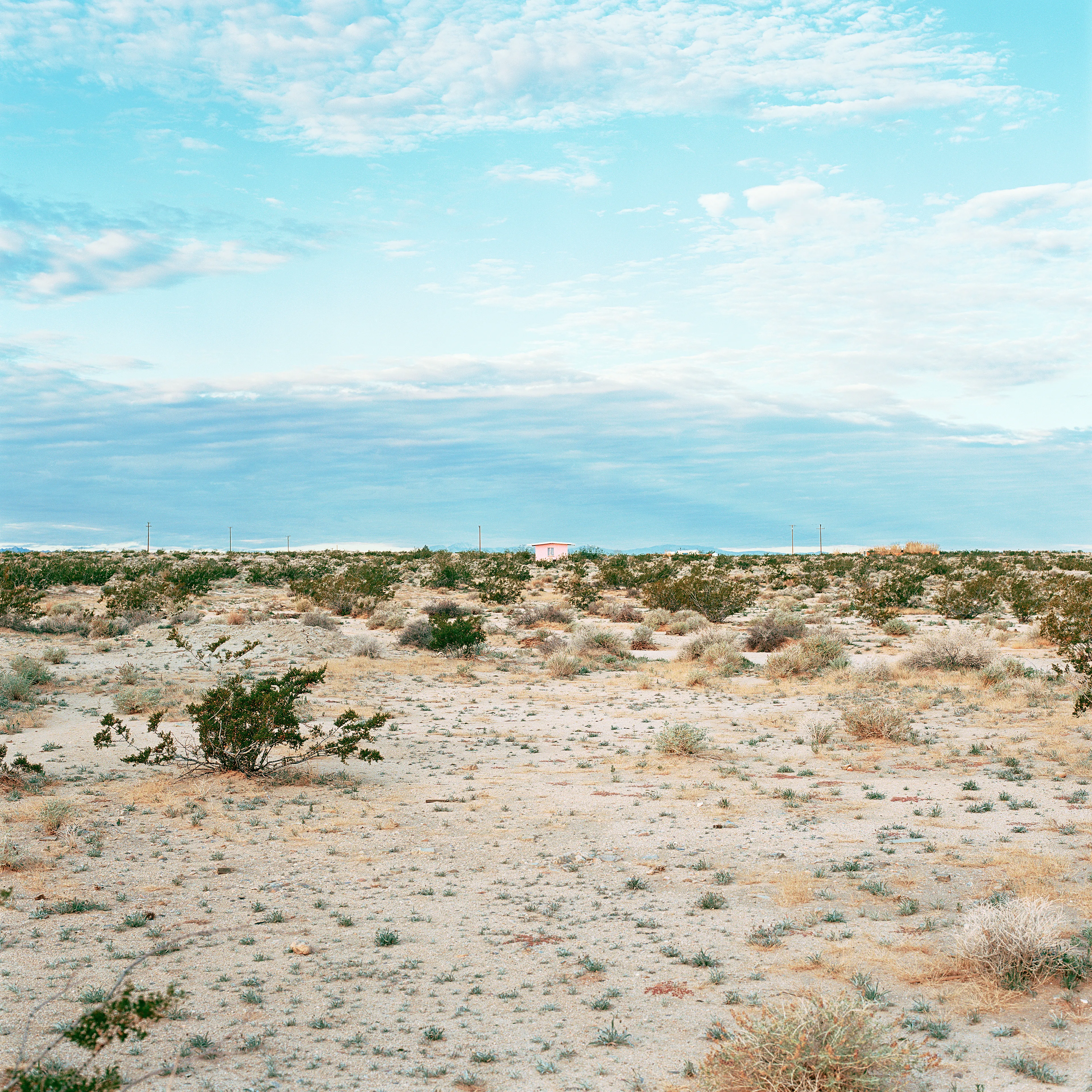 “These are photographs of isolated structures in the high desert of Southern California. All of the images are made in the east end of the Morongo Valley Basin, Wonder Valley, and the area surrounding the town of Twenty-Nine Palms. This is an area approximately one hundred- and fifty-miles due East of Los Angeles. From the oceans edge in L.A., to the area that I am photographing, the landscape is continuously occupied. This area is the final edge of a vast urban expanse. For social, financial, or personal reasons individuals are pushed, or pulled, or simply seek this literal cultural edge. Beyond this point is unoccupied desert.  In the past I have perused projects which dealt with the iconography of transcendence and the sublime. In other projects I have investigated the literal desire to get "outside" of or beyond the cultural (a desire with the ironic consequence of transforming the natural into the very condition one wishes to escape). It is this conceptual trajectory which has led me to this current body of work. This current body of work is an extension of the investigation begun in the "four landscape" portfolio. The structural rigor of that work has been replaced with concerns which are aesthetic and social. On the simplest level I am drawn to the vernacular character of the architecture (painted with a Home Depot palette) as well as the amazing visual character of these structures on this vast desert plain lit by an extraordinary light. However, at base, my primary interest is to create images which are iconographic of a desire. A desire to be "beyond", a desire to be alone, a sign of man on the landscape”. - John Divola.

Edition: 1 of 1