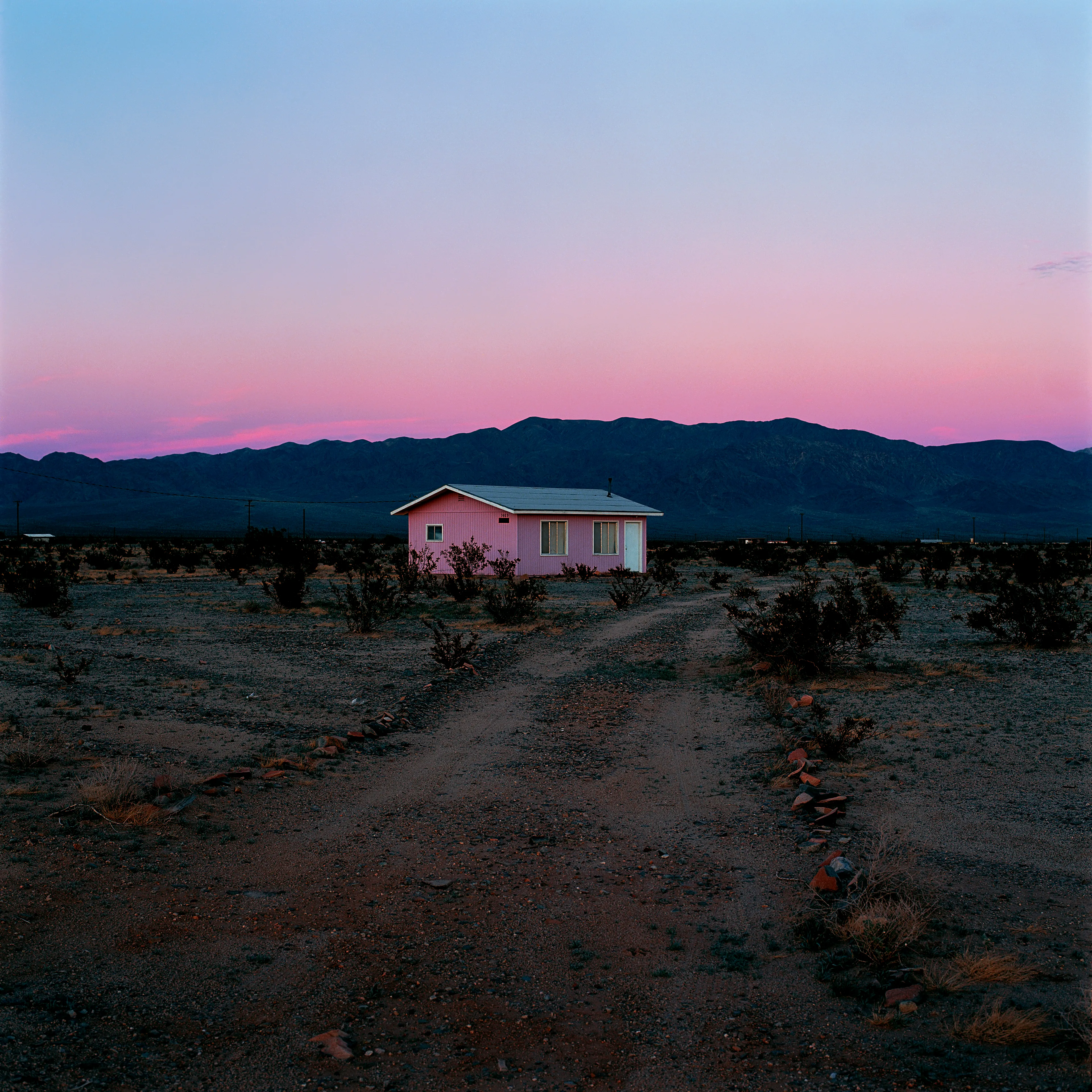 “These are photographs of isolated structures in the high desert of Southern California. All of the images are made in the east end of the Morongo Valley Basin, Wonder Valley, and the area surrounding the town of Twenty-Nine Palms. This is an area approximately one hundred- and fifty-miles due East of Los Angeles. From the oceans edge in L.A., to the area that I am photographing, the landscape is continuously occupied. This area is the final edge of a vast urban expanse. For social, financial, or personal reasons individuals are pushed, or pulled, or simply seek this literal cultural edge. Beyond this point is unoccupied desert.  In the past I have perused projects which dealt with the iconography of transcendence and the sublime. In other projects I have investigated the literal desire to get "outside" of or beyond the cultural (a desire with the ironic consequence of transforming the natural into the very condition one wishes to escape). It is this conceptual trajectory which has led me to this current body of work. This current body of work is an extension of the investigation begun in the "four landscape" portfolio. The structural rigor of that work has been replaced with concerns which are aesthetic and social. On the simplest level I am drawn to the vernacular character of the architecture (painted with a Home Depot palette) as well as the amazing visual character of these structures on this vast desert plain lit by an extraordinary light. However, at base, my primary interest is to create images which are iconographic of a desire. A desire to be "beyond", a desire to be alone, a sign of man on the landscape”. - John Divola.

Edition: 1 of 1