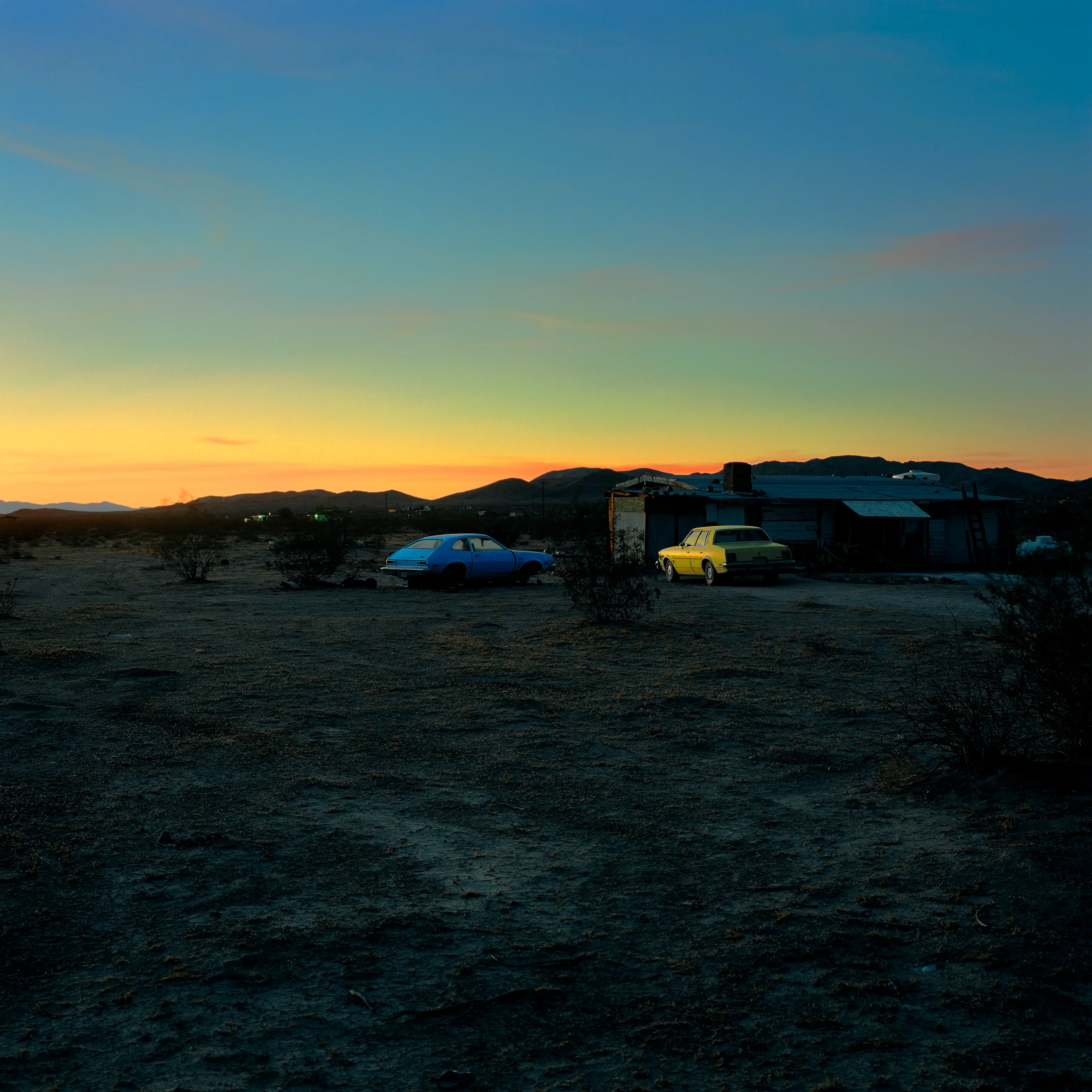 “These are photographs of isolated structures in the high desert of Southern California. All of the images are made in the east end of the Morongo Valley Basin, Wonder Valley, and the area surrounding the town of Twenty-Nine Palms. This is an area approximately one hundred- and fifty-miles due East of Los Angeles. From the oceans edge in L.A., to the area that I am photographing, the landscape is continuously occupied. This area is the final edge of a vast urban expanse. For social, financial, or personal reasons individuals are pushed, or pulled, or simply seek this literal cultural edge. Beyond this point is unoccupied desert.  In the past I have perused projects which dealt with the iconography of transcendence and the sublime. In other projects I have investigated the literal desire to get "outside" of or beyond the cultural (a desire with the ironic consequence of transforming the natural into the very condition one wishes to escape). It is this conceptual trajectory which has led me to this current body of work. This current body of work is an extension of the investigation begun in the "four landscape" portfolio. The structural rigor of that work has been replaced with concerns which are aesthetic and social. On the simplest level I am drawn to the vernacular character of the architecture (painted with a Home Depot palette) as well as the amazing visual character of these structures on this vast desert plain lit by an extraordinary light. However, at base, my primary interest is to create images which are iconographic of a desire. A desire to be "beyond", a desire to be alone, a sign of man on the landscape”. - John Divola.

Edition: 1 of 1