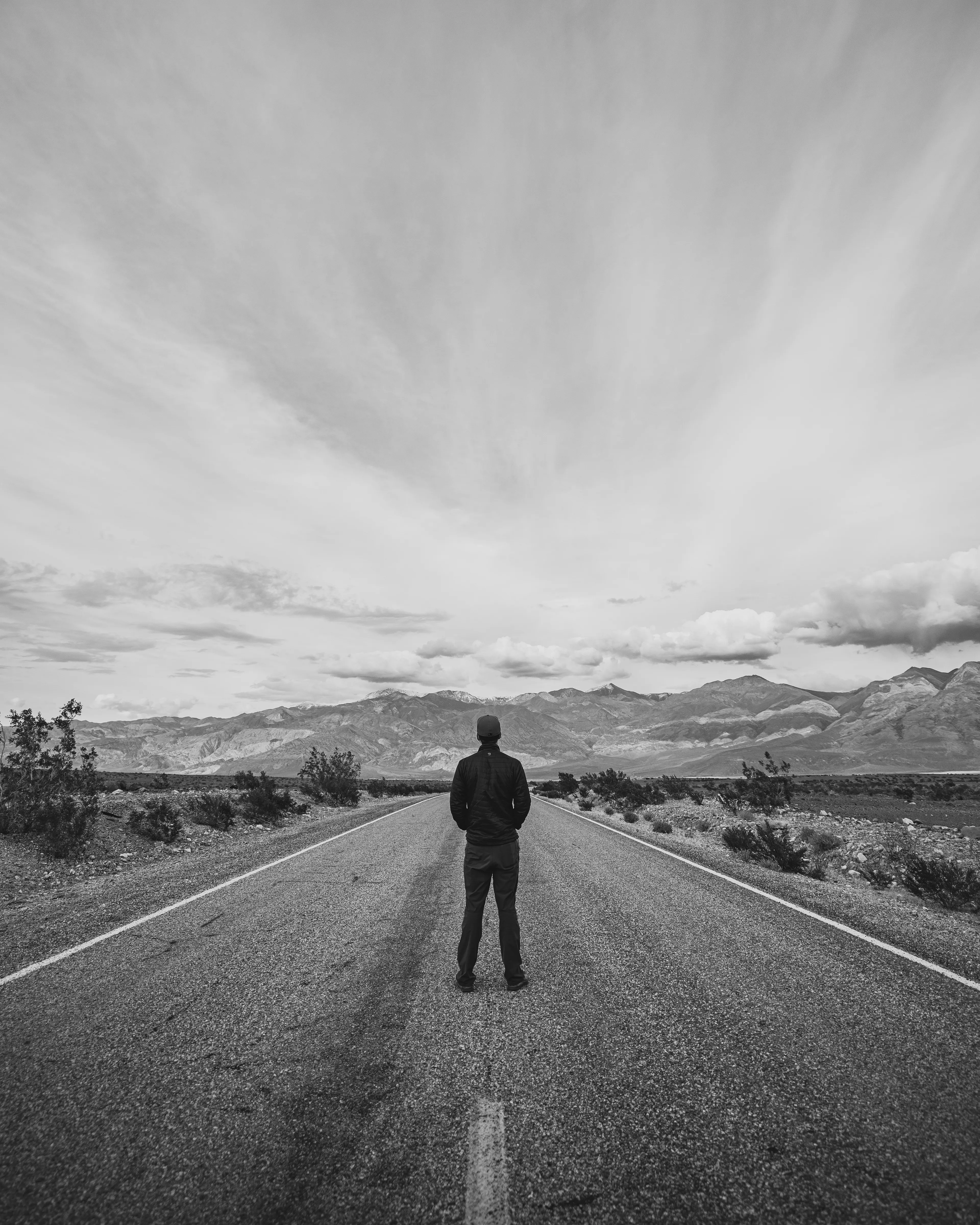 Standing still at the center of an empty road, the horizon feels both distant and inevitable. The mountains ahead rise quietly, worn by time, mirroring the weight of decisions not yet made and miles not yet walked.