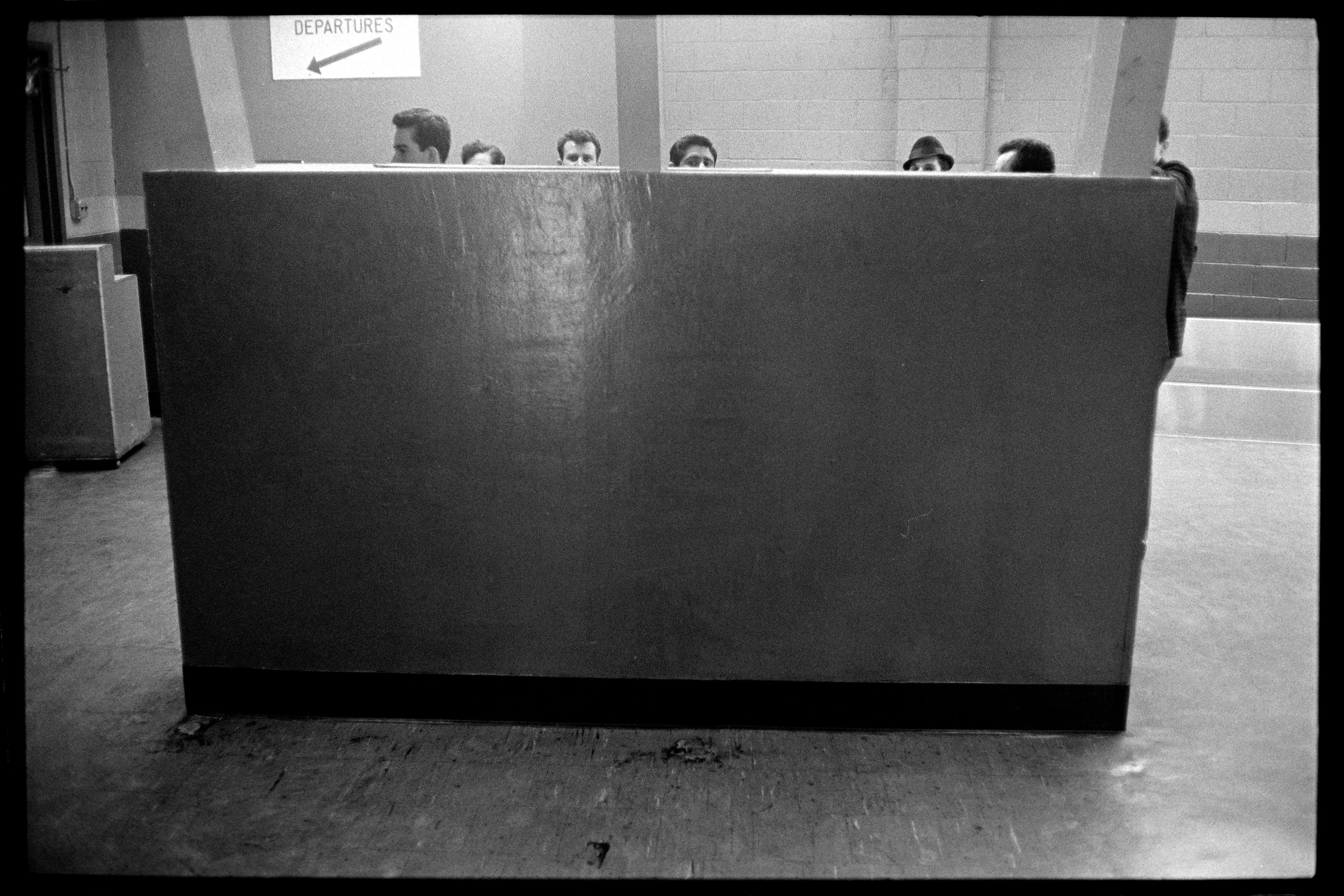 JFK Airport, New York City, USA, 1966

In a 1966 snapshot from JFK airport, small heads are seen hovering over a counter near the boarding gate, seemingly resting on the surface.