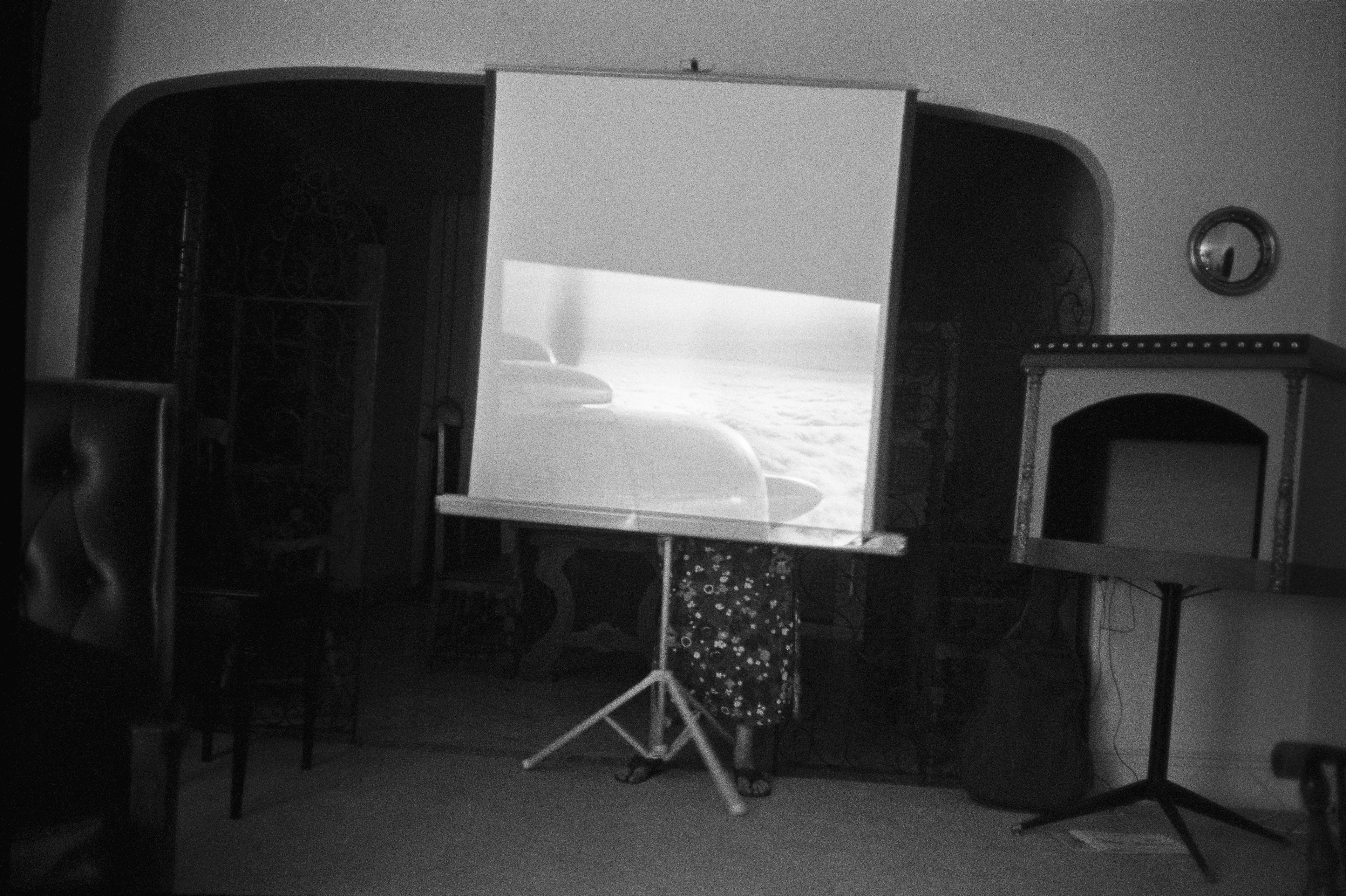 New Jersey, USA, 1966

A woman is adjusting a home movie screen that displays an image of airplane propellers, captured from the window of the plane. Near her is a miniature theatre set on a stand, and the image from this darkened space seamlessly transitions into the next photograph."