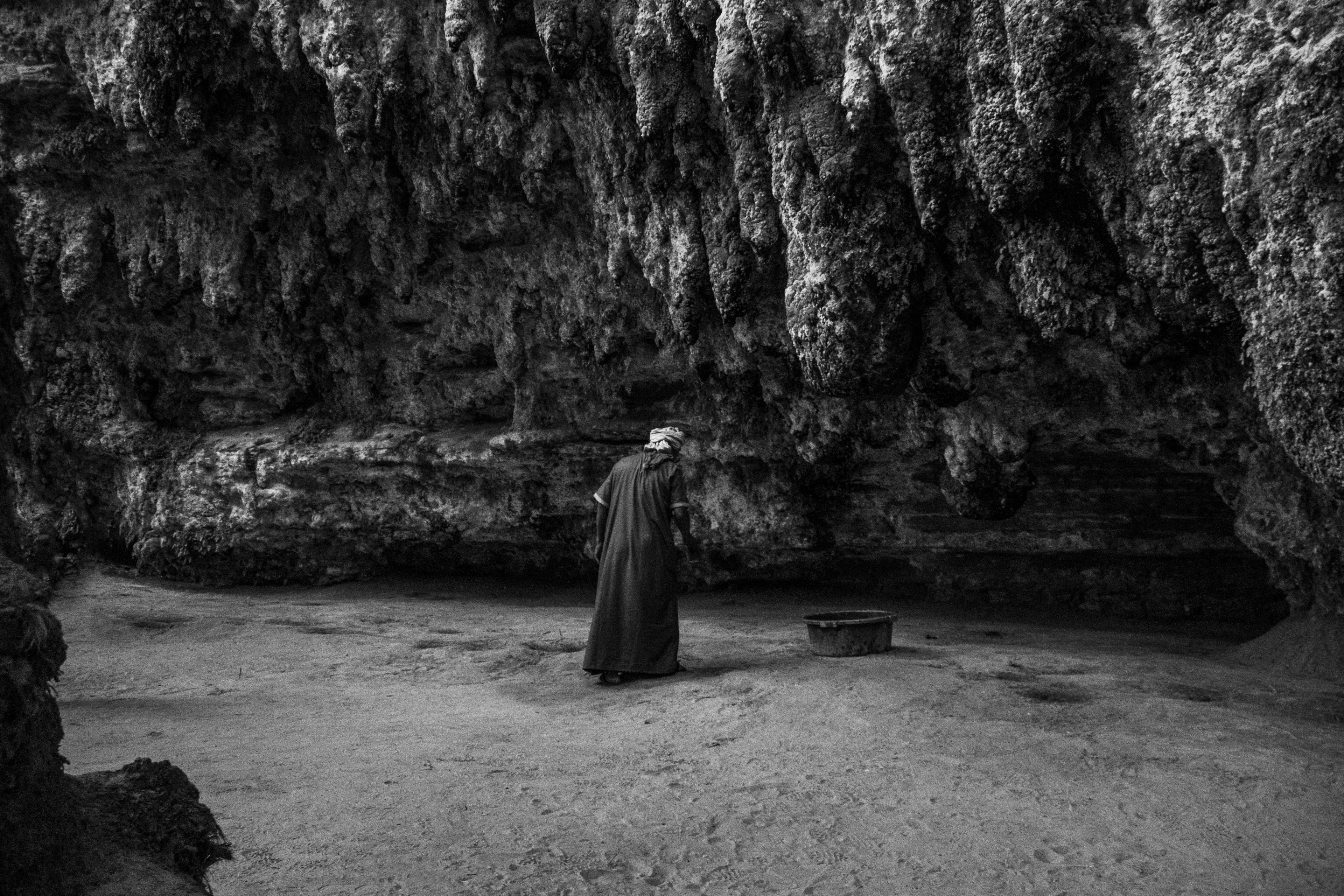 At the trickling waters of Terjit oasis, a man leans forward to watch the stream fall gently onto the sandy floor, a rare and precious reminder that water is life in the vast desert.