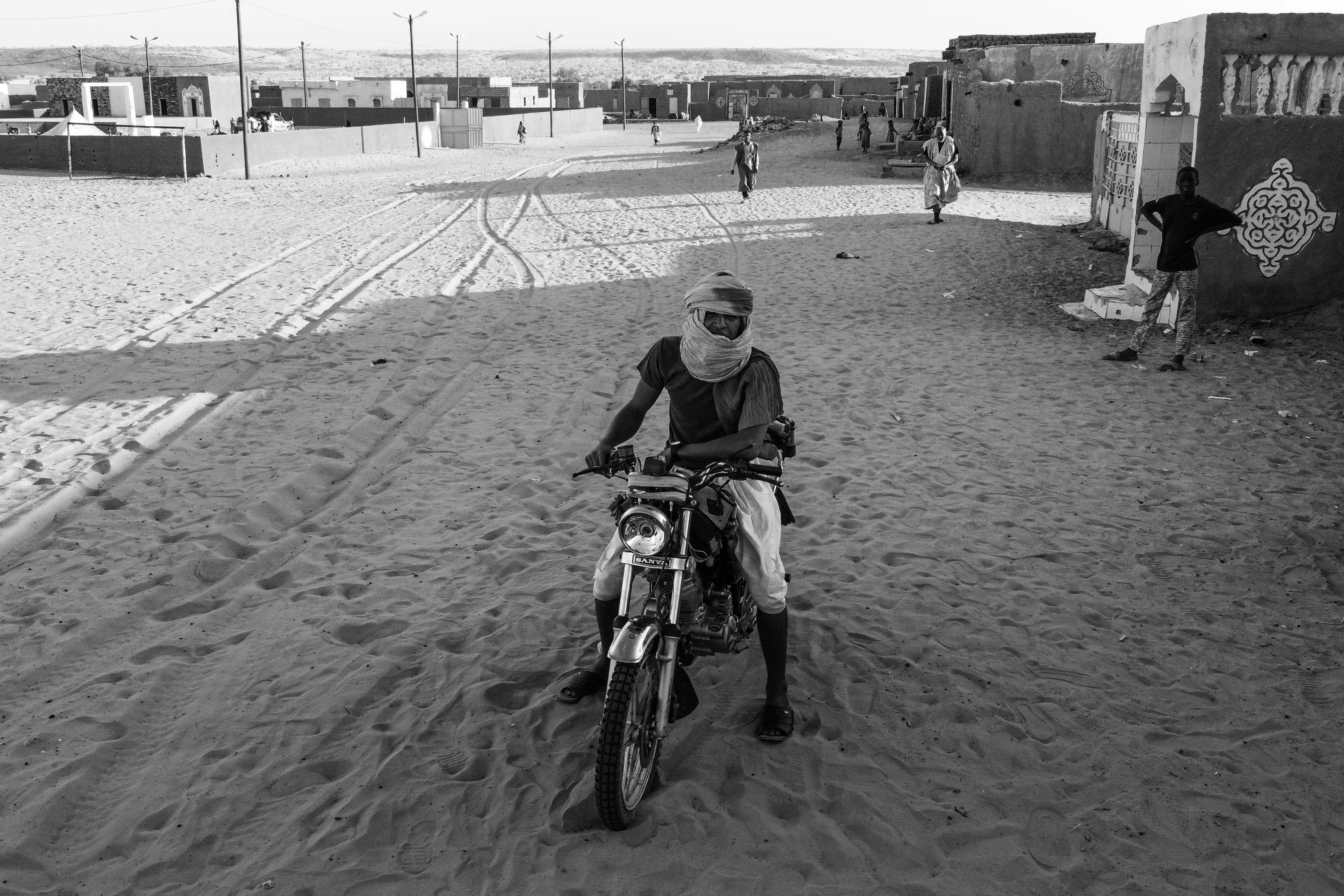 A desert journey calls for courage and curiosity. Who can imagine the countless paths carved on motorcycles across endless dunes and barren stretches of desert, right here at the edge of Mali. The desert nomads, ever-adaptable, are shifting their ways of travel; trading the slow, steady pace of camels for the speed and freedom of motorcycles and cars, embracing a new rhythm while still rooted in timeless lands.