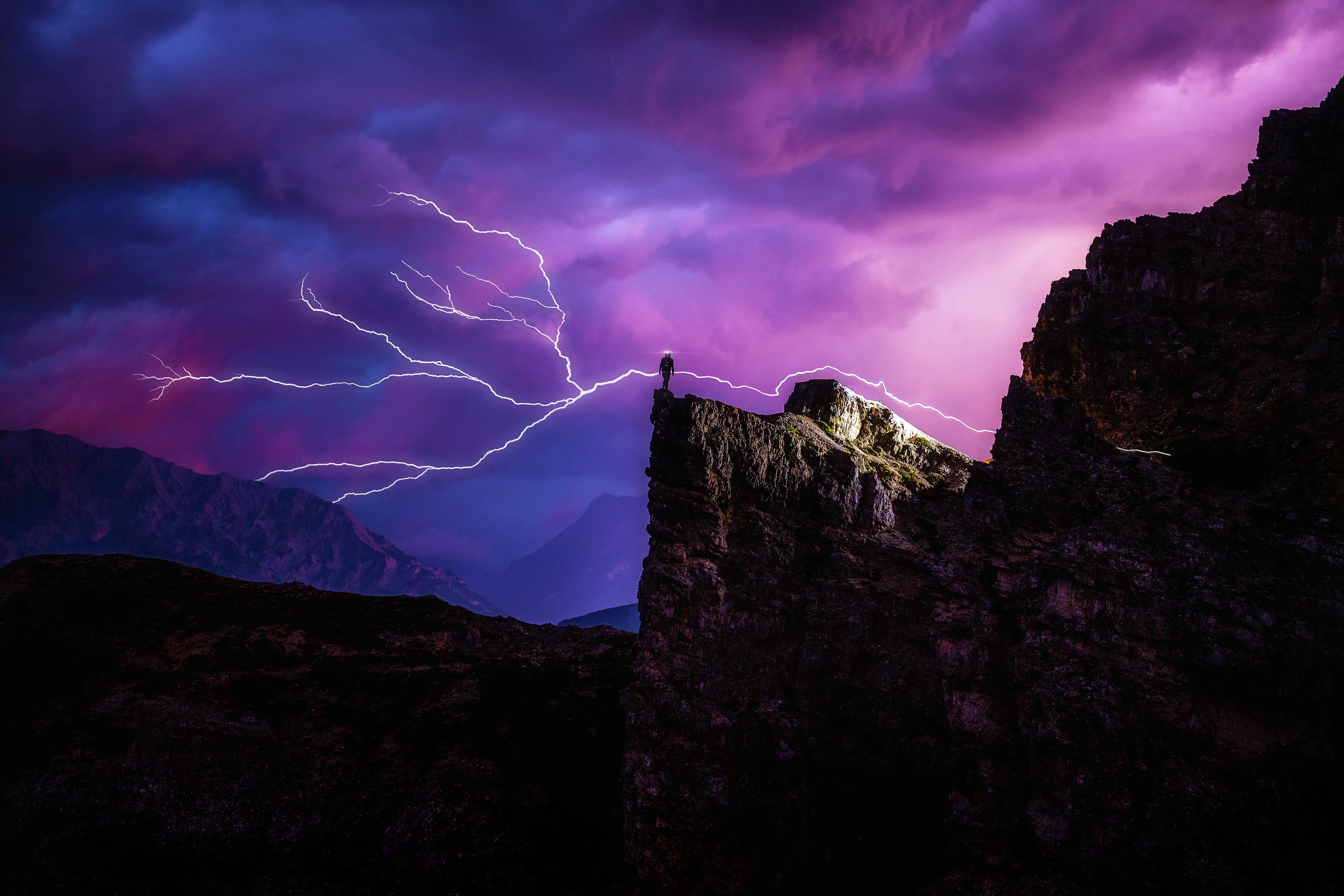 By the light of our headlamps and distant lightning strikes, we trekked out from Tre Cime to the rock outcropping we had scouted earlier that day. 

Darkness fell quickly, and scattered drops of rain began to land.

The landscape was cast a midnight blue, diverting to an electric lavender after every thunder. We took each step carefully, loose rocks and gravel below our feet tumbling down into the valley.

I had a vision for the creation and now it was time to execute.

I stepped up to the ledge, knees trembling. The torch on my head had indicated my path, yet it now only diminished into the void. A bolt of lightning emanating from my figure signifies the divergence from an isolated pursuit into a cosmos of creativity.

The storm drew closer, and my group began their way back to find cover as I continued to shoot the approaching fog. The trails of their lamps can be seen traveling half a mile down the slope.

The illuminated hostel in the distance beckoned us to get back quickly. and to my own demise, I did not listen. 

I stood there behind only my tripod, fully exposed to the elements. The drizzle of rain turned quickly into a torrent, and I realized my mistake. I rushed to pack my camera into my bag, scrambling down the rock face to try and catch up with the others. 

The floodgates opened, dirt turned to mud, every rock turned slick, the light on my headlamp sunk to a flicker. I had only the distant glow of the hostel and the ring of cowbells to guide me home.

As I stumbled along what I could make of the trail, it was very clear that I was in the hands of mother nature. and I would likely only make it to the light if she decided I was deserving.

I had reached the final incline toward shelter when I felt the hair on my head begin to rise. I looked through my fogged glasses to see an electrical pole, 20 feet in front of me, light up like a times square billboard. it was as if someone had unloaded a shotgun next to my ear. I stood waveringly in the electrified air, unsure of how to comprehend how close I had just come to being burnt to a crisp.

There’s nothing like a bolt of lightning nearly being sent through your body to open your mind to the cosmos.

End chapter one.
