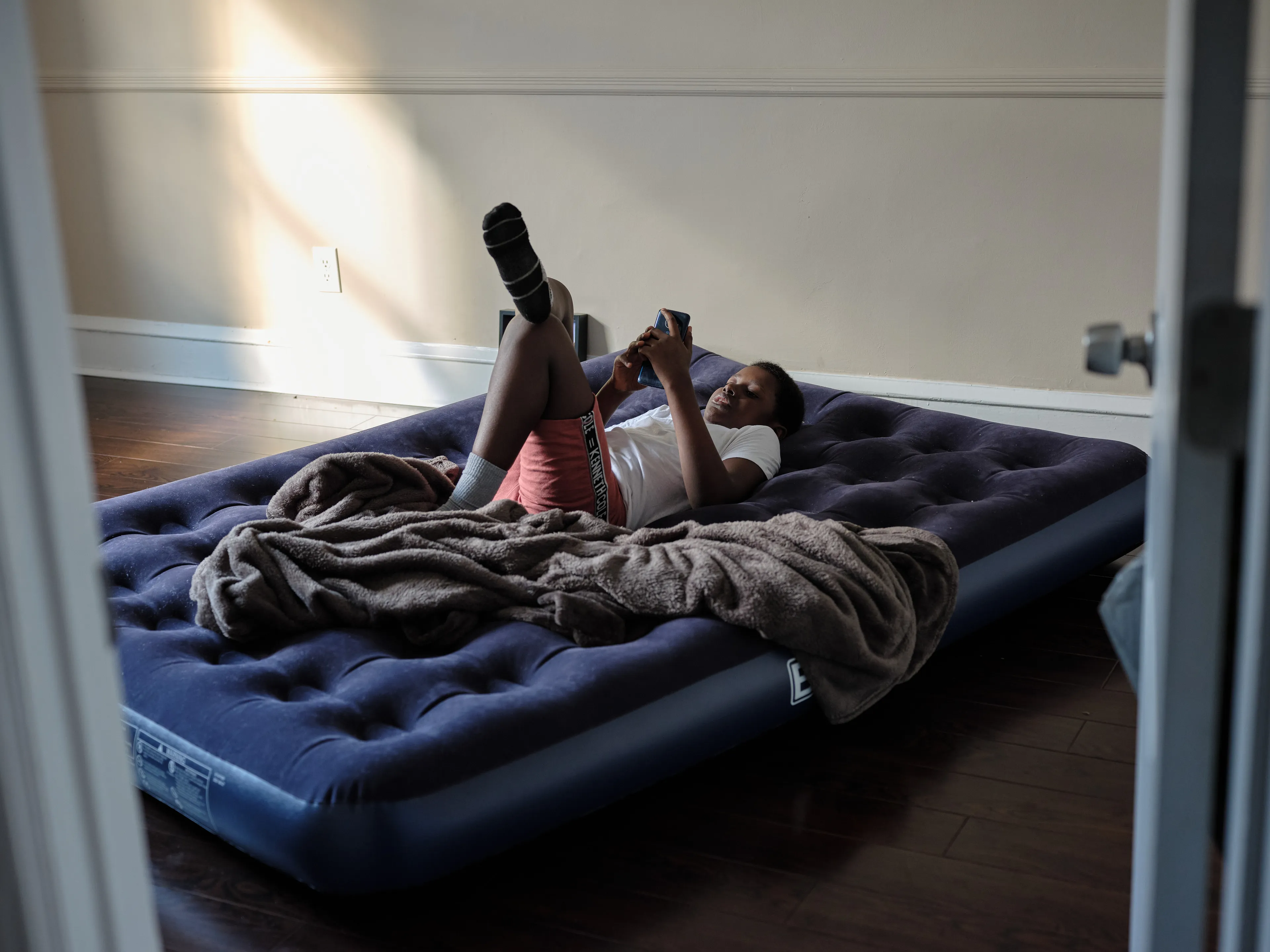 It's Expensive to be Poor #27 Zahir's New Room by Hannah Price

I wanted to create a project on the costs of being poor. About how the U.S. system and bills keep the poor behind and dig a deeper hole in their life. In my research, I found a single mother of 32 years being neglected by affordable housing: Lisa McKine.

I first saw Lisa on a Philly Instagram page called nogunzone; it reposts police news and share reports from people in the community. I find it more informative than the local news, however I know several people who choose not to tune in for mental health reasons; it shows all the bad and we are currently on track to outdo last year’s homicide rate. 

Days after a tragic fire in another Philadelphia affordable housing apartment (PHA) that killed 12 people, a social media trend began with videos of people sharing themselves holding burning cigarettes near a silent smoke alarm. One in particular caught my eye, Lisa’s video of her son, telling him to wake up as a bunch of flies flew off his face.

Lisa did not grow up poor, she was raised by her dad and stepmother. Her dad worked for Philly managing janitorial duties in the courthouse. Her parents separated when she was young and it wasn’t until her 20’s when she learned bad habits from her biological mother of working the system. Lisa found herself a single mother of 2 and living in her first apartment of PHA affordable housing for ten years.

Lisa’s brother, Raul Gore (Bobby, 27) is currently on probation and has dealt with his own circumstances. He told me about the decisions he made in his early twenties that put him in and out of jail. He knows he can’t change how irresponsible he was but is now enjoying life with his family and providing for them. He works during the week and his wife on the weekends, they take turns watching their children. The environment Bobby grew up in at a younger age was surrounded by cops who watched him and his friends go to and from school. He remembers having fun with the cops by making them chase him and his friends. 

My first visit to Lisa’s place was at the beginning of March. There was an exterminator outside her building with hoses hooked up to an apartment on the second floor. Inside her apartment I noticed a particular odor and counted at least two roaches and one dead in the kitchen cabinet. Lisa had been complaining about the roach infestation to PHA since 2020, sharing records of failed exterminations and the summer of 2021 is when the flies started. The infestation has forced her to live out of bins and plastic bags. PHA exterminates the apartment every month and denies Lisa from moving to a new place. 

While photographing Lisa, I learned she has an associate in Applied Science in Construction Management from the college I work at. We crossed paths in 2018 but never met each other. Sharing personal frustrations, we spent a lot of time together as we both needed someone to just hear us and provide emotional support. Her boys Zaahir (11) and Quamir (5) are well behaved, social and sweet. Lisa provides for them all by driving Uber, bartering with her community, making and selling her own hair and skin products, as well as providing different hair services and body contouring.  

Luckily, Lisa found help to make a few months' deposit on rent for a new house outside of affordable housing. Through her 4 businesses, she plans to cover her rent of $2500. Lisa’s new house windows will help with her mood and knowing her dad is 13 minutes away in a nursing home should relieve some stress. Lisa’s dad had a stroke, causing bleeding in the brain which forced him to remove the left side of his brain. Her step mother also had brain surgery due to a horrible fall, and now both her parents are bed ridden while they recover from surgery.

Witnessing Lisa’s life, I imagined myself in her situation. A single mother unhappy in an infested home, barely getting by where the only way out is taking a huge risk renting a house not knowing she can afford it. The point of this NFT is to give back to the community, specifically Lisa so I have shared Lisa’s wallet address with you below.

The more time I spent with Lisa, the closer we became. We talked about dating and tried to provide emotional support for each other’s lives. I don’t become friends with all my subjects, but those who don’t have a problem expressing and sharing their feelings, I tend to share back. One day, I couldn’t help but break down crying and another day Lisa needed to as well. It was when we had planned to take the photograph in the window from the outside perspective that she was telling me how her dad was transferred to a different hospital. Wondering why, she demanded to see him and discovered he had a large infected bed sore that went up his back. From the photo, the scab looked at least 2’ long and 1’ wide with a fist sized faint sore. Why did they wait so long to tell Lisa? More neglect. Lisa would love to take care of him herself if she had known. In the end, Lisa still wanted to make the photograph, she wanted to keep her promise and help me with my project. I said no, but ultimately gave in even though it was completely dark out. My plan was to catch the sun setting. However, life isn’t what we plan it to be. During the photo, I could hear Lisa praying to God and her ancestors, full of sadness, hope and joy. 

To keep up with Lisa, follow her on Instagram @lovelylisa215, @hollywoodglamour.co, @mckine_building_group

Donate ether to Lisa’s address:  0x0cE11858dc7f01E6c2bEB9d1f2F6cb273484076e

Edition: 1 of 1

Commissioned by Obscura