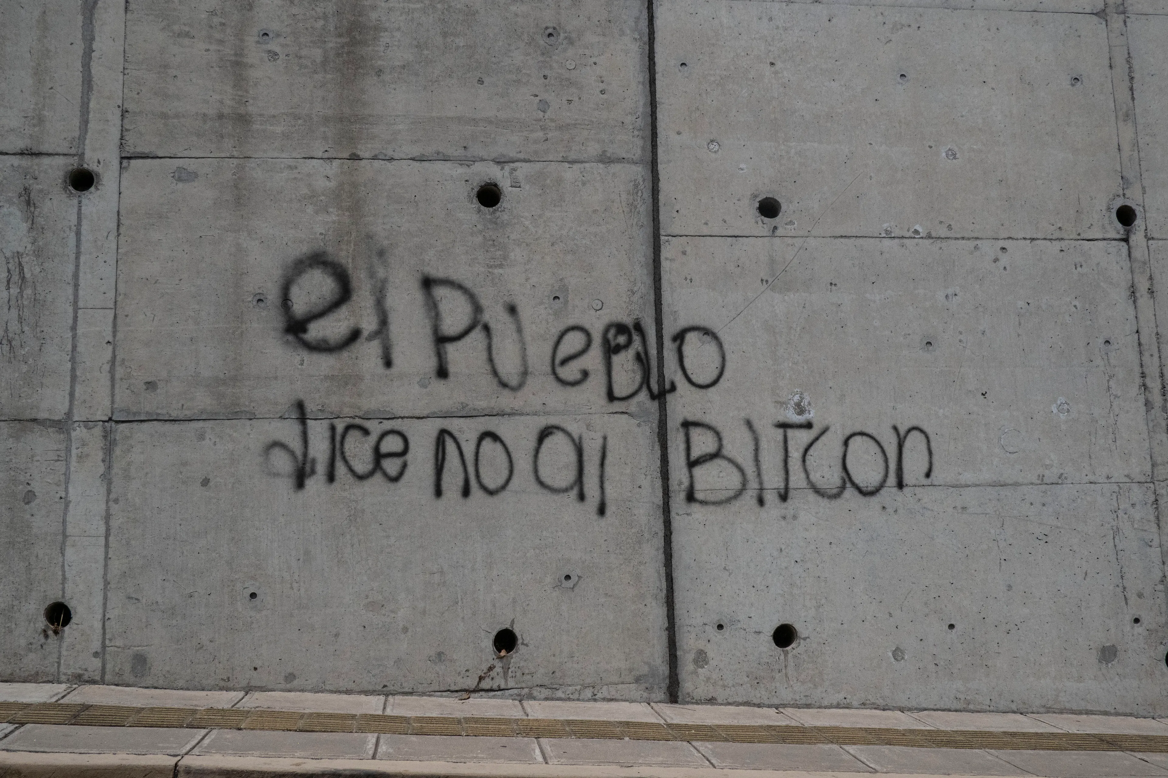 « Bitcoin Nation » #10 by Thomas Dworzak

EL SALVADOR, San Salvador, 2022/3-4. "The people say NO to Bitcoin", graffiti on highway underpass.

« Bitcoin Nation » - El Salvador - Thomas Dworzak / Magnum Photos

Many photographers and journalists of my generation, interested in war and conflict, would at one point read Richard Kapusciznsky's all-time classic "The Soccer War" and watch Oliver Stone's "Salvador. » The latternow feels insanely cheesy. With the country's troubled history in mind and never having been to Central America, I found "Bitcoin Nation - El Salvador" a challenging theme to explore for this NFT project. 

I set out to straightforwardly document this alien and invisible world of bitcoin, and being 'in the realm of crypto,' I hoped it would give me access to President Nayib Bukele's surprise project. Last year he had suddenly declared Bitcoin the official currency of El Salvador - which until now was only the US dollar. The 40-year-old president of Palestinian origin started out as an anti-establishment candidate, describing himself as "the world's coolest dictator," but soon took an authoritarian turn. Yet he continues drumming the bitcoin beat, and bitcoin celebrities from all around the world keep flocking to El Salvador.
The Pacific beach town of El Zonte became "Bitcoin Beach," and "Volcano Bonds" and "Bitcoin City" are meant to be the future.

When official doors remained closed for me, I started digging for clues in the county's troubled past and present or anything, even remotely, related to the bitcoin world. Vignettes of the bloody civil war regularly popped up, and I came across a few "bitcoin events." The sudden spike of almost a hundred homicides in the course of one weekend in late March, due to what seemed a breakdown of a secret deal between the government and the two main gangs, had President Bukele declare a state of emergency, martial law and intensify the war on the gangs. I could see fringes of it. But nothing compared to the brutality of
the spectacularly filmed daily government propaganda videos of mass arrests and more-than-rough prisoner handlings I watched on TV, Twitter, and Instagram.

It was at a small bitcoin event that I found a hint why I may have been shunned and didn't get any access to show the "shiny world of Bitcoin Nation," as I had hoped. My NFT ticket was definitely the "wrong church" in the Bitcoin world. To paraphrase one of the speakers: "If I want to gamble, I go to Vegas and party with beautiful hookers, instead of being a loser, sitting around in my basement, frustrated, minting NFTs. Shitcoins."

El Salvador and the President were meant to be guests of honor at the Bitcoin 2022 conference in Miami. But due to the internal tension, he canceled the visit, and the 30+ thousand delegates had to discuss the future of bitcoin without him.

Edition: 1 of 1

Commissioned by Obscura