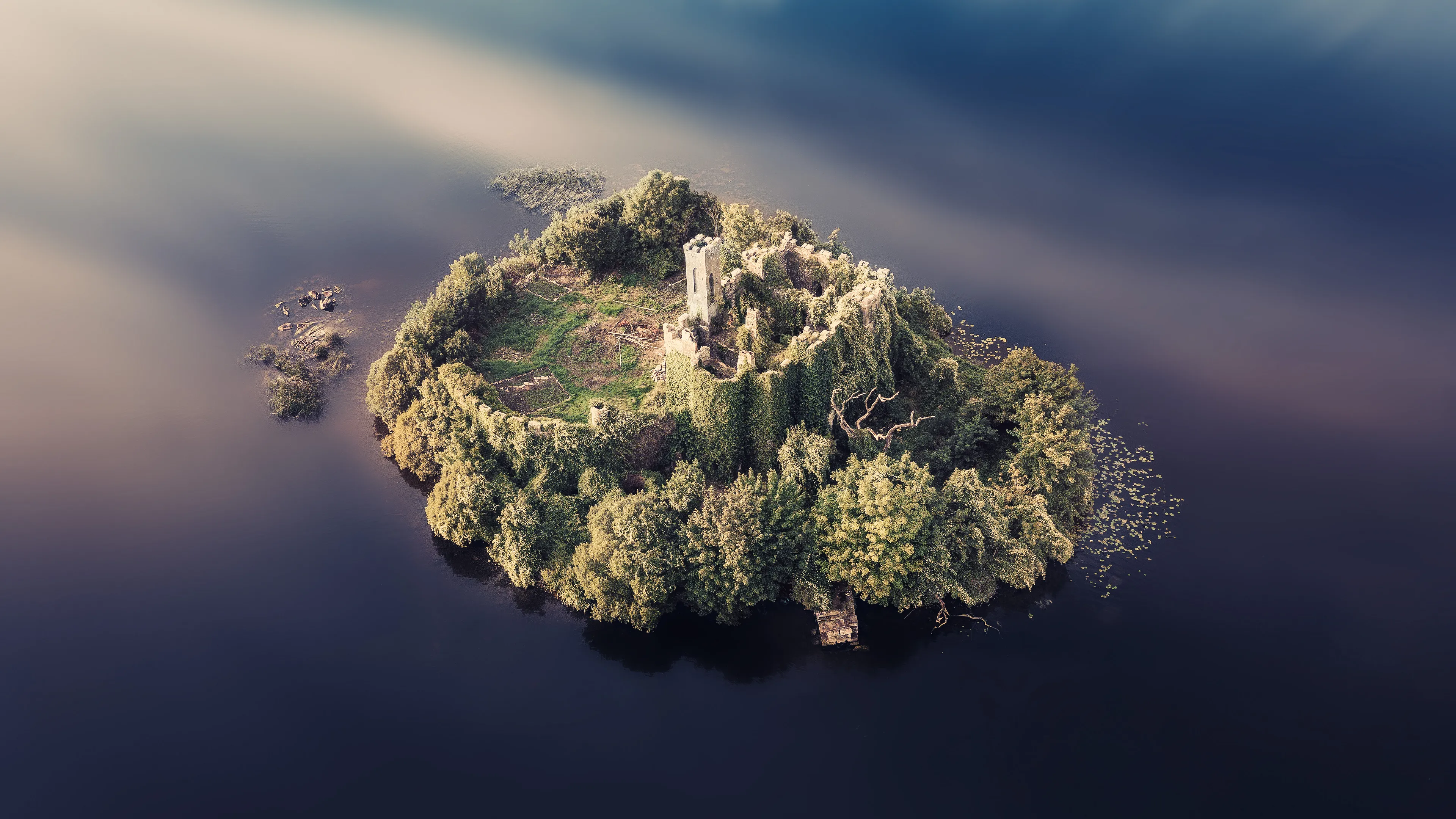 I had imagined for years how I would like to photograph this castle. At dawn, with fog and a mystical atmosphere.

When the time finally came, the weather was not at all to my liking. 
But when I flew the drone over the castle and saw the reflection of the sky, I came up with the idea of a composition with the castle floating on the clouds. 
In retrospect, I'm glad I did, because I was able to capture it in a unique way.

Info:
McDermott's Castle is located on a small island in Lough Key in County Roscommon, Ireland. The history of this castle goes way back to the Middle Ages, when it served as the seat of the McDermott clan. However, the current building was built in the 19th century in the neo-Gothic style and reflects the romantic ideas of the time.

The castle was abandoned towards the end of the 19th century and has been largely uninhabited ever since. Due to its age and lack of maintenance, it is in a dilapidated state, which gives it a special, enchanted atmosphere. Despite its dilapidated state, the castle continues to attract visitors who are drawn to its picturesque location and mystical aura.
