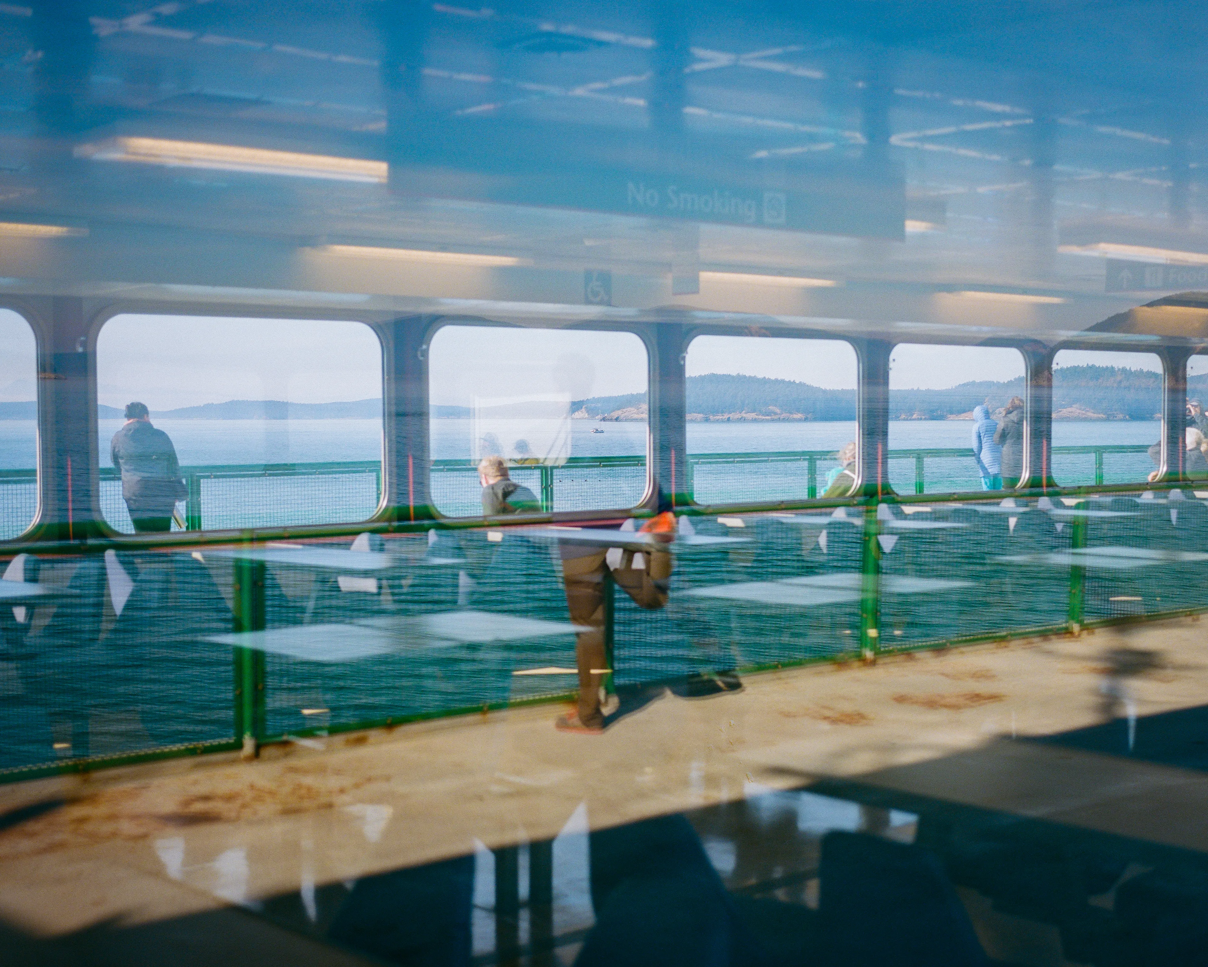 Leaving Orcas Island on a cold, but sunny September day, I came across the opportunity to capture three scenes in one single frame. 

Behind me, reflected in the window's glass, a passenger was getting their morning stretch in. 

Just beyond the glass in front of me, there were empty seats in a seasonally-closed section of the ferry. 

Looking through that closed section were passengers on the other side of the ferry deck, framed in the windows.

Please enjoy, "Transparent Reflections".